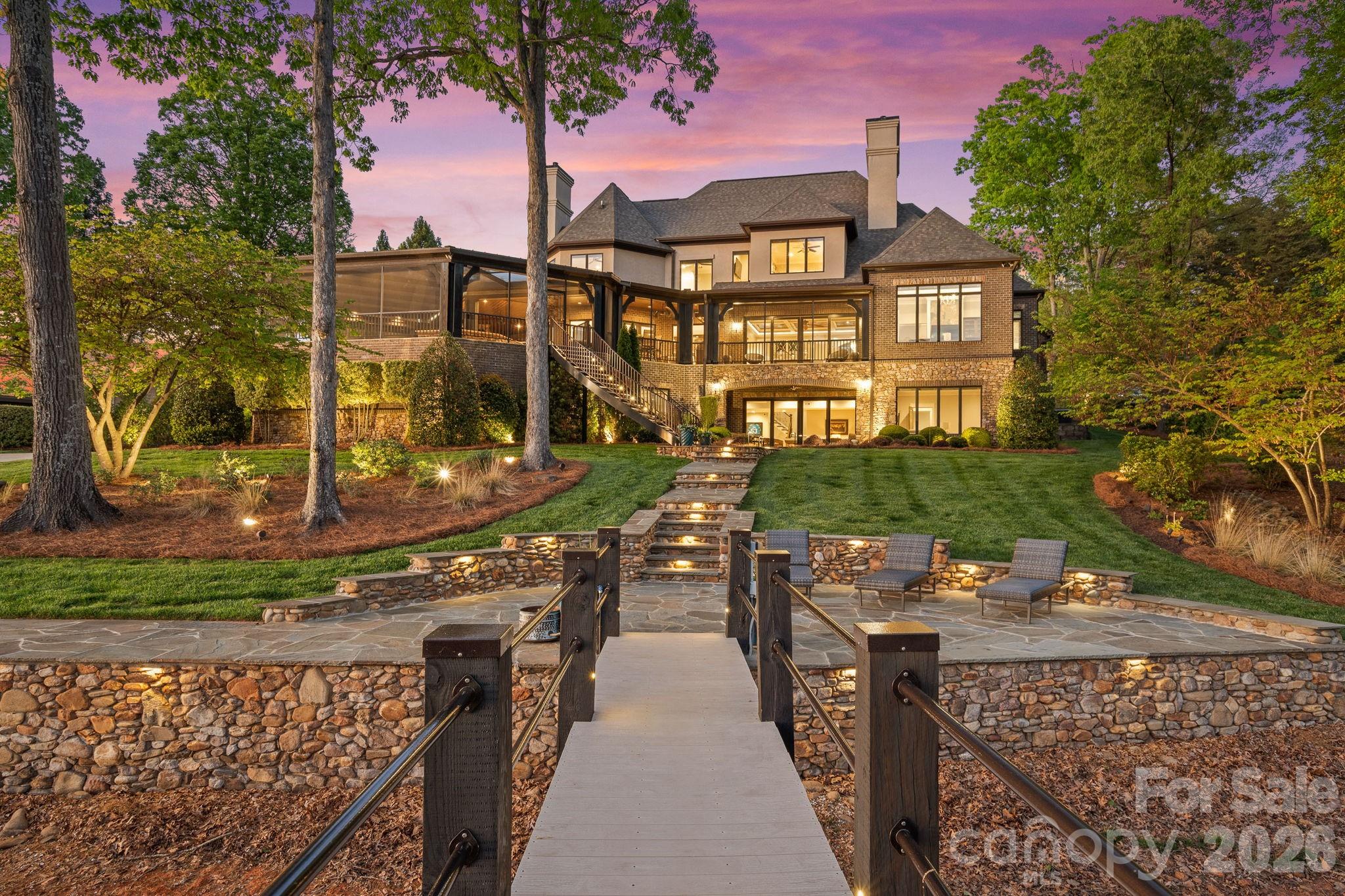 Located just beyond The Point, in one of the most sought-after and exclusive stretches of Lake Norman, this property offers the perfect balance of prestige, privacy, and open water access. Here, life slows down in the best way—mornings on the porch with coffee, afternoons on the water, and evenings spent soaking in golden skies from your own backyard.
The home itself is built for both comfort and connection. The expansive main level invites effortless living, with a spacious primary suite and open-concept design that flows seamlessly to a stunning screened veranda and resort-style pool—perfect for hosting or simply enjoying the peaceful waterfront setting. An elevator ensures ease and accessibility throughout.
Upstairs, guests are treated to their own private retreat with three bedrooms, each featuring en suite baths, and incredible water views, along with a large bonus living space ideal for entertaining or relaxing after a day on the lake.
The lake level transforms into the ultimate gathering space—an entertainer’s dream with a dedicated office, workout room, game room, and an additional two-car garage car enthusiast showroom (four-car total), designed as a true retreat. Whether it’s game day, a weekend getaway with friends, or quiet evenings by the water, this level offers unmatched versatility and lifestyle appeal.
Step outside to your beautifully lit outdoor spaces and follow the path to a covered private dock with deep water access and a private boat ramp and custom stone sea wall and boardwalk.