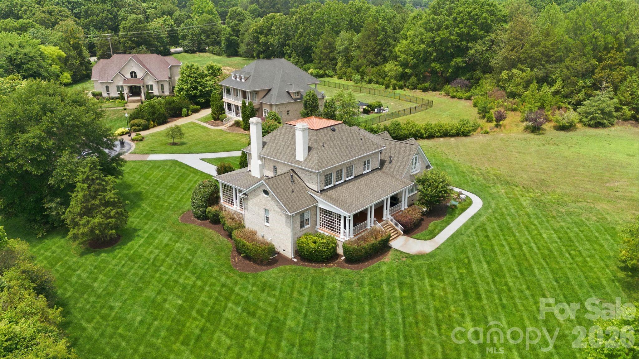 Designed for both elegant entertaining and comfortable everyday living, this beautifully crafted home is tucked within an exclusive gated community in Marvin, offering a lifestyle defined by privacy, beauty, and convenience. Surrounded by mature landscaping and peaceful natural views, the property provides a rare sense of retreat while remaining just minutes from the dining, boutiques, fitness studios, and everyday conveniences of Waverly, Blakeney, Ballantyne, and South Charlotte. The home is also conveniently located near some of the area’s top-rated schools, further enhancing the appeal of this exceptional location.
From the moment you enter, the home’s sense of scale and warmth is immediately apparent. Soaring ceilings, extensive millwork, oversized windows, and plantation shutters create a timeless interior filled with natural light and refined architectural detail. Every space has been thoughtfully designed to feel both elevated and welcoming, blending sophistication with true livability.
The dining spaces and gathering areas flow effortlessly, creating an ideal backdrop for everything from intimate dinners to holiday celebrations and relaxed evenings at home. Expansive windows frame tranquil views of the surrounding greenery, bringing a sense of calm and connection to nature throughout the home. Rich hardwoods, gracious room proportions, and detailed trim work add to the home’s classic architectural character while still feeling fresh, understated, and comfortable.
The primary suite serves as a true private retreat, offering generous proportions, serene natural light, and a spa-inspired bath complete with dual vanities, a soaking tub, walk-in shower, and oversized custom closet. Secondary bedrooms and flexible living spaces provide versatility for guests, home offices, fitness, media, or creative spaces, adapting effortlessly to both everyday routines and special occasions.
Designed with functionality in mind as much as beauty, the home offers exceptional storage, expansive living areas, and an oversized garage rarely found in today’s market. Whether enjoying slow mornings overlooking the private grounds, entertaining friends and family, or simply returning home to the quiet comfort of the neighborhood, this property offers a lifestyle centered around elegance, privacy, and ease within one of Marvin’s most desirable gated communities.