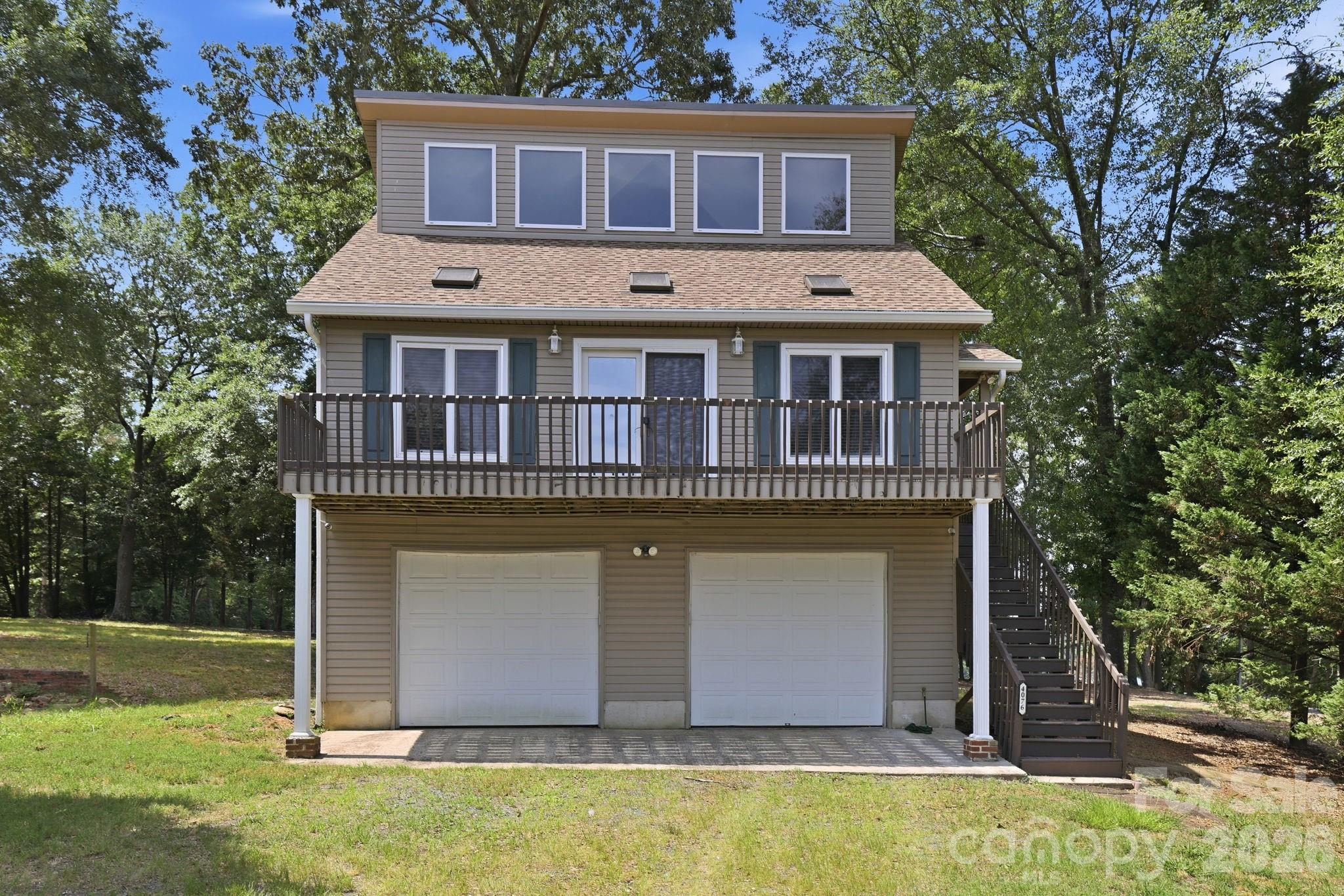 Enjoy beautiful, year-round views of Lake Wylie without the restrictions of an HOA! Nestled on a spacious 1-acre lot, this property offers privacy, potential, and an impressive list of recent updates. Major improvements include a new roof, gutters with gutter guards, whole-house plumbing, and a new septic system—all completed in 2025—as well as a new HVAC system in 2024 and new garage doors in 2023.
A gravel driveway leads to the oversized two-car garage, providing plenty of space for parking, storage, or a workshop. Inside, you’ll find a bright, open living area featuring rare wide-plank red cherry hardwood flooring and French doors that open to an elevated deck overlooking Lake Wylie, an ideal spot to relax and enjoy the view in every season. The kitchen offers solid wood cabinetry, tile counter tops, an oversized sink, and ample storage. The main-level bedroom features generous closet space and beautiful tongue-and-groove oak flooring. Upstairs, the spacious loft-style bedroom includes a half bath and a nook that could easily be converted into a closet. (Per MLS guidelines, this room meets the criteria for a bedroom except for the absence of a closet.)
The refrigerator, washer, and dryer will convey with the home.  Conveniently located near Lake Wylie access, parks, dining, shopping, schools, and I-77, this home combines peaceful lakeside living with everyday convenience.