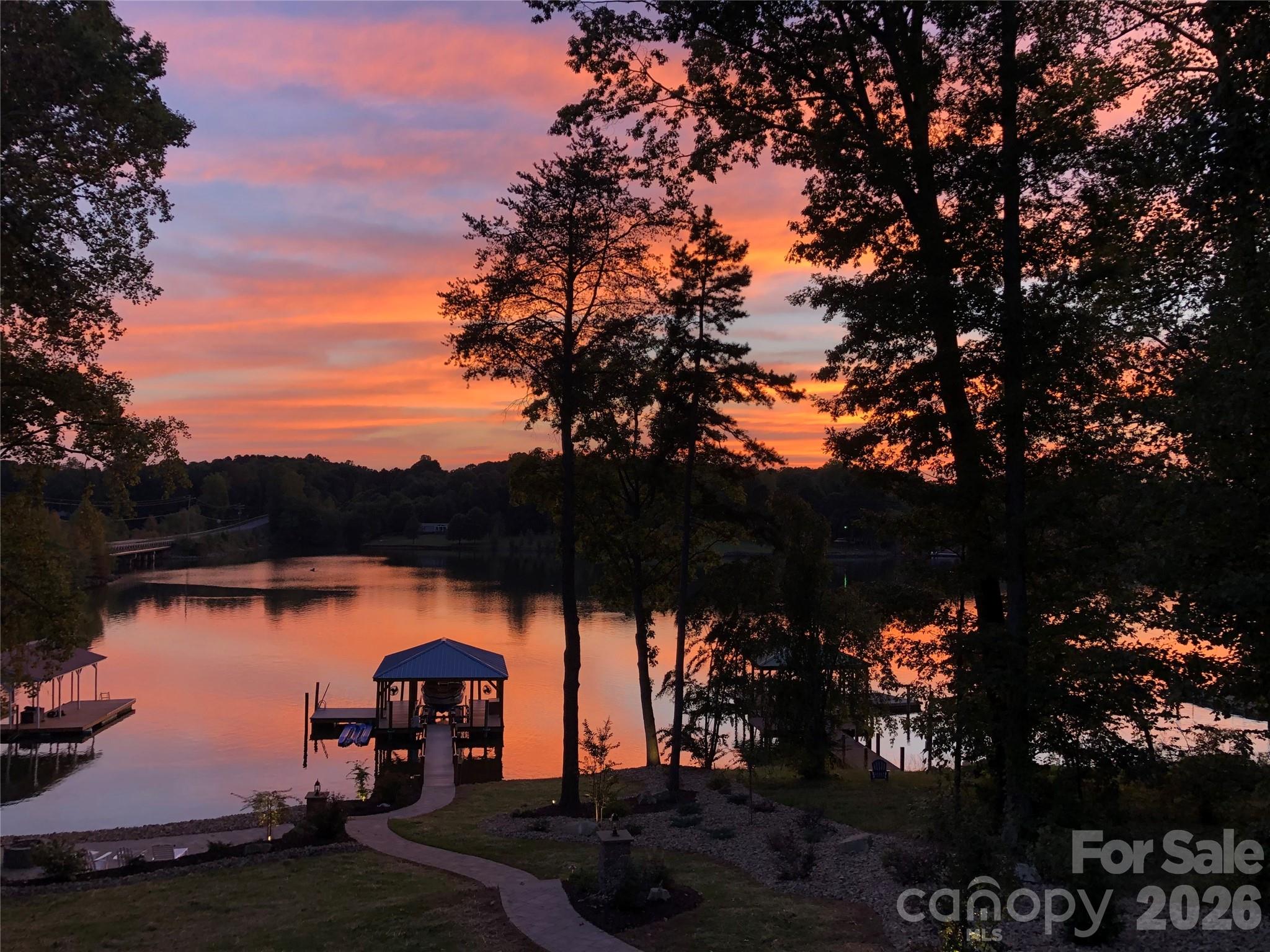 PRICED BELOW APPRAISAL – FULLY FURNISHED– TURNKEY WATERFRONT WITH DOCK + SUNSET VIEWS ON LAKE NORMAN

Welcome to a luxury waterfront residence on Lake Norman, offering a rare combination of refined interior upgrades, highly functional outdoor living, An exceptional opportunity to secure a fully furnished, move-in ready waterfront home positioned on open water with a private dock and sunset-facing views—now offered below appraised value. Walk-out lower level offers significant expansion potential—ideal for adding living space, guest suite, or increasing overall value. Property offers potential for future detached garage/guest suite addition (subject to buyer verification and permitting), creating an opportunity to further expand functionality and value.

Built in 2018 and significantly upgraded beyond builder standards, this property delivers the rare combination of condition, location, and immediate usability that today’s buyers are searching for.
Vaulted ceilings and expansive windows frame wide lake views and fill the open-concept living space with natural light. The kitchen is designed for both everyday living and entertaining, featuring River Marble flooring, upgraded granite, and premium appliances including a Bosch dual-fuel range, warming drawer, Bosch dishwasher, and LG refrigerator. The oversized peninsula creates a seamless flow into the dining and living areas, anchored by a gas fireplace and direct access to a sunroom overlooking the water.
Hickory hardwoods extend throughout the main living areas and bedrooms. The primary suite captures lake views and offers functional convenience with direct access to the laundry room. Interior finishes include crown molding, custom window treatments, and well-appointed baths with a soaking tub.
Outdoor living is where this property separates itself. A maintenance-free deck with a fully equipped outdoor kitchen and electric awning overlooks the lake, while professionally designed landscaping—with over 100 tons of river rock—creates a polished, low-maintenance setting. A lighted pathway leads to a lakeside patio with fire pit and down to the private dock.
The covered dock includes an 8,000 lb boat lift, sun pad, and dual jet ski ports—ideal for immediate lake use or short-term rental income potential.
Additional features include a whole-home generator, 10x12 storage building, and walk-in basement with partially finished bath offering expansion potential. No HOA.
Offered fully furnished for a true turnkey experience.
Ideal as a full-time residence, second home, or investment property with strong rental appeal.
Opportunities like this—priced below appraisal, fully furnished, and ready for immediate enjoyment—are limited on Lake Norman. Schedule your showing today.