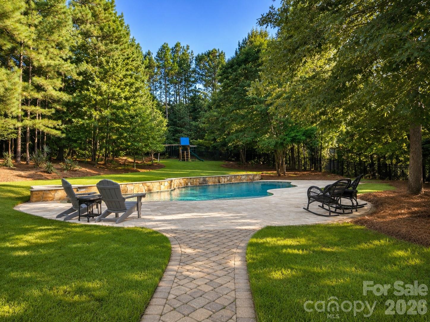 Welcome home to your own private retreat in sought after Trinity Ridge neighborhood. Set on 1.45 fenced acres surrounded by mature trees, this custom home was designed to capture the beauty of its setting. Walls of oversized windows overlook the backyard from the great room, kitchen, breakfast area, and primary suite, creating views that bring the outdoors in. Whether you're enjoying your morning coffee, gathering with family, or watching the seasons change, the connection between the home and its surroundings is something truly special.
The backyard is designed for year-round enjoyment with a custom pool and spa, expansive paver patios and walkways, fireplace, outdoor kitchen, large fenced yard, and wooded privacy. 
Inside, a grand two-story foyer opens to an executive office with floor-to-ceiling wood paneling and stone fireplace, a formal dining room with a stepped tray ceiling, and a two-story great room featuring a wall of arched windows and a see-through fireplace shared with the keeping room.
The gourmet kitchen serves as the heart of the home with custom cabinetry, granite counters, stainless steel appliances, 6 burner gas stove, decorative vent hood, walk-in pantry, and a large island with seating. Open to the breakfast area and keeping room, the layout flows naturally to the screened porch and outdoor living spaces.
The main-level primary suite offers a private retreat with a stepped tray ceiling, fireplace, sitting area, and same gorgeous views of the backyard. The en-suite bath features separate vanities, a jetted soaking tub, tiled walk-in shower, and walk in closet with custom built-ins including drawers, shelving, and shoe storage.
Additional features include Brazilian hardwood floors throughout the main living areas and upstairs hallway, extensive crown molding and millwork, coffered and tray ceilings, multiple fireplaces, a screened porch, three-car garage, and generous secondary bedrooms plus bonus room. Located just minutes from new Harris Teeter, shopping, dining, and top-rated Fort Mill Schools including Catawba Ridge HS, this home offers an estate setting with the convenience of Fort Mill living.
Homes with this level of privacy, lot size and outdoor living are rarely available.