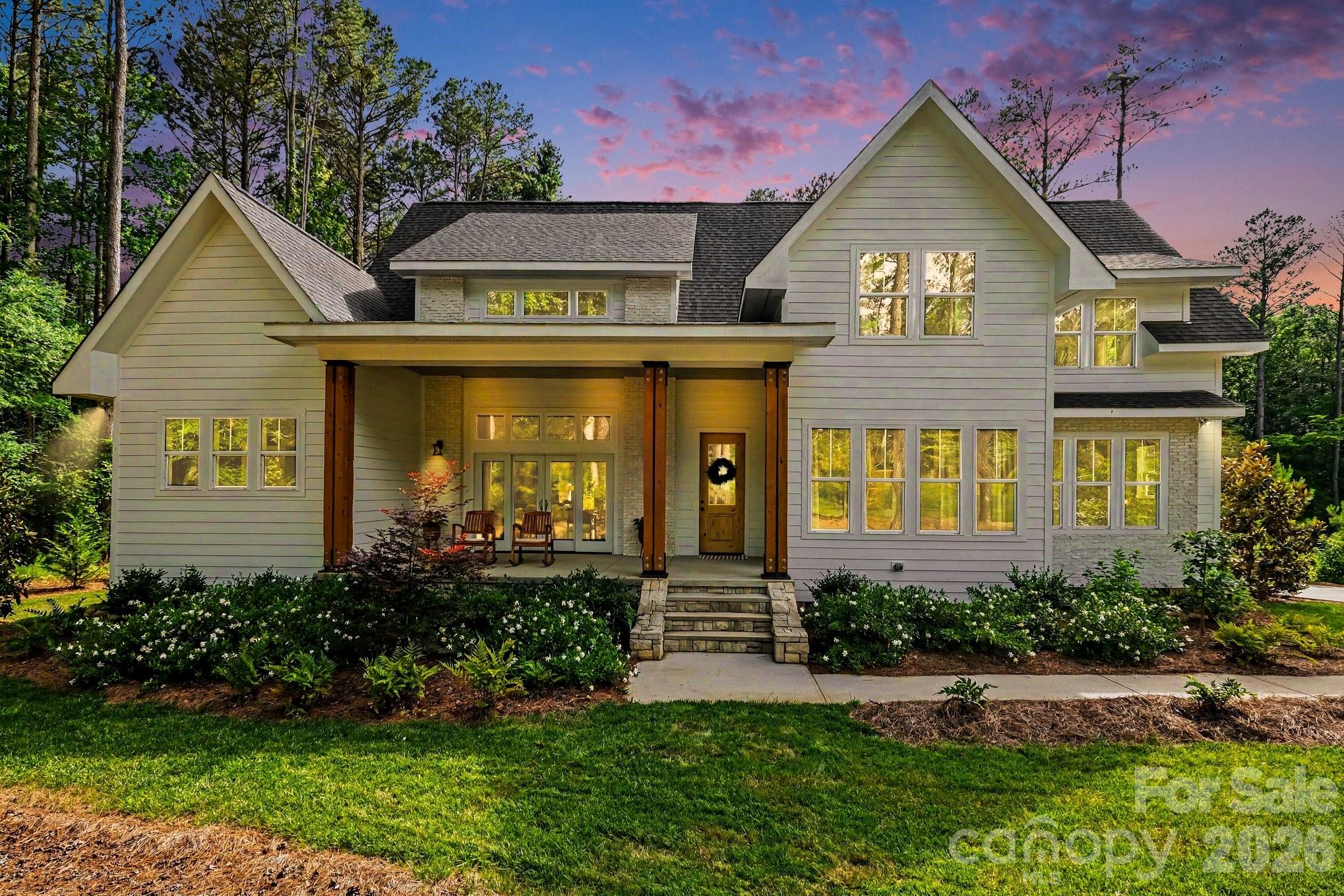 Beautifully crafted custom home offering upgraded finishes, exceptional flexibility, and serene wooded backyard privacy. The striking exterior showcases crisp white siding accented by warm wood columns, stone details, double front doors, and modern black lighting. Inside, an open and airy floor plan is filled with natural light and highlighted by soaring ceilings, designer lighting, and wide-plank rustic wood flooring sourced from trees harvested on the property.
The spacious great room living space offers seamless access to front and rear covered porches, creating ideal indoor-outdoor living expandable for entertaining. The chef’s kitchen features a bold center island with butcher block countertop and bar seating, quartz countertops, subway tile backsplash, five-burner gas range with hood, convenient butler’s pantry with wine fridge, and a walk-in pantry. An adjacent dining area completes the open-concept design.
The main-level primary suite is a slice of heaven with cathedral ceilings accented by wood beams, direct access to the rear patio, and peaceful wooded views. The windows allow lots of natural light without compromising privacy. The premier ensuite bath includes dual vanities, a soaking tub, and a tiled walk-in shower. A private office, spacious mudroom with built-ins, laundry area, and oversized side-entry garage complete the main level. Upstairs, a versatile loft provides additional living space alongside three generously sized bedrooms. Two bedrooms share a Jack-and-Jill bath, and a dedicated craft/storage closet adds convenience.
A standout feature of the home is the separate bonus living area with private rear entrance, offering exceptional flexibility for guests, multigenerational living, a studio, office, or recreation space. The lower level features impressive 14-foot ceilings and lounge space, while the upper level includes a kitchenette, dining area, and full bath.
Outdoor living is equally impressive with a covered rear porch featuring a stone fireplace, multiple seating areas, and expansive backyard space with mature landscaping, garden area, and lush tree canopy for added privacy. A full cabana bath off the porch and ample room for a future in ground pool to further enhance the property.
Residents of Riverchase Estates enjoy the peace and quiet of this location along with the resort-style amenities including a The clubhouse at Riverchase Estates which is part of a $4.5 million world-class amenity center, which includes a state-of-the-art fitness center, a resort-style pool, and a ballroom. It is designed for socializing and community meetings, making it a central feature of the community. The amenities include basketball, tennis, pickle ball courts, picnic area, playground, pond, street lights, walking trails and 500 acre nature preserve and access to the Catawba River, all conveniently located less than 15 minutes from shopping, dining, and everyday conveniences in Indian Land. If you are looking for a new lifestyle - come explore this opportunity today!