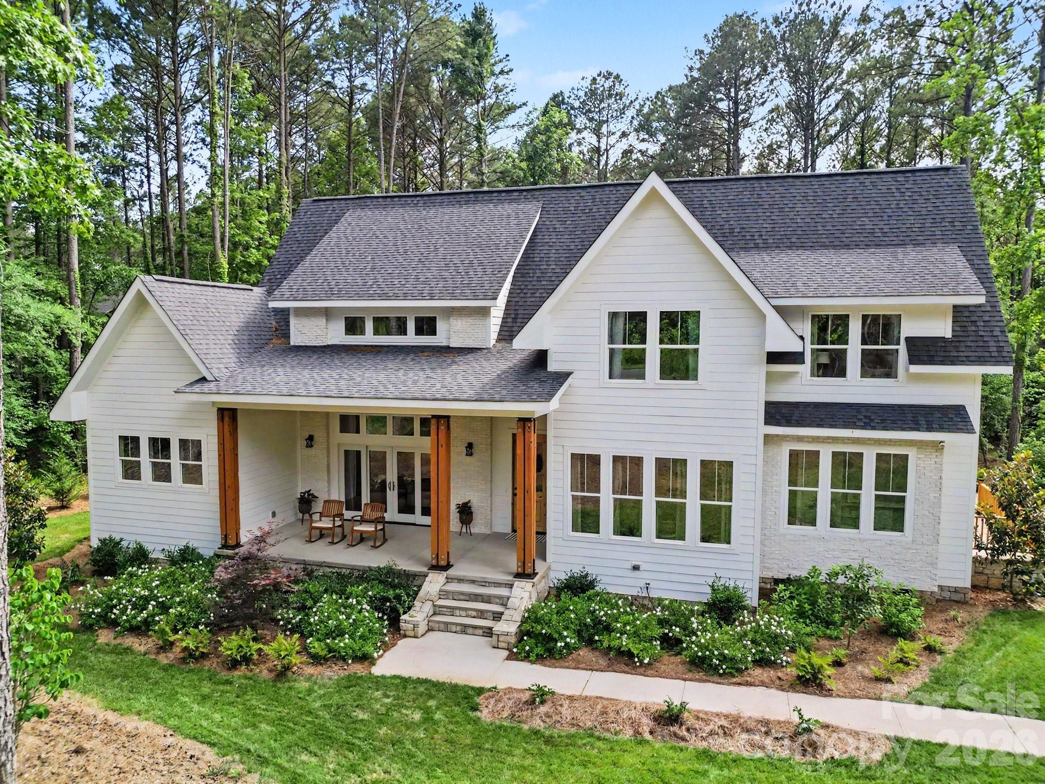 Beautifully crafted custom home in sought-after Riverchase Estates offering luxury finishes, exceptional flexibility, and serene wooded privacy. The striking exterior showcases crisp white siding accented by warm wood columns, stone details, double front doors, and modern black lighting. Inside, an open and airy floor plan is filled with natural light and highlighted by soaring ceilings, designer lighting, and wide-plank rustic wood flooring sourced from trees harvested on the property.
The spacious great room living space offers seamless access to front and rear covered porches, creating ideal indoor-outdoor living expandable for entertaining. The chef’s kitchen features a bold center island with butcher block countertop and bar seating, quartz countertops, subway tile backsplash, five-burner gas range with hood, convenient butler’s pantry with wine fridge, and a walk-in pantry. An adjacent dining area completes the open-concept design.
The main-level primary suite is a slice of heaven with cathedral ceilings accented by wood beams, direct access to the rear patio, and peaceful wooded views. The windows allow lots of natural light without compromising privacy. The premier ensuite bath includes dual vanities, a soaking tub, and a tiled walk-in shower. A private office, spacious mudroom with built-ins, laundry area, and oversized side-entry garage complete the main level. Upstairs, a versatile loft provides additional living space alongside three generously sized bedrooms. Two bedrooms share a Jack-and-Jill bath, and a dedicated craft/storage closet adds convenience.
A standout feature of the home is the separate bonus living area with private rear entrance, offering exceptional flexibility for guests, multigenerational living, a studio, office, or recreation space. The lower level features impressive 14-foot ceilings and lounge space, while the upper level includes a kitchenette, dining area, and full bath.
Outdoor living is equally impressive with a covered rear porch featuring a stone fireplace, multiple seating areas, and expansive backyard space with mature landscaping, garden area, and lush tree canopy for added privacy. A full cabana bath off the porch and ample room for a future in ground pool to further enhance the property.
Residents of Riverchase Estates enjoy the peace and quiet of this location along with the resort-style amenities including a The clubhouse at Riverchase Estates which is part of a $4.5 million world-class amenity center, which includes a state-of-the-art fitness center, a resort-style pool, and a ballroom. It is designed for socializing and community meetings, making it a central feature of the community. The amenities include basketball, tennis, pickle ball courts, picnic area, playground, pond, street lights, walking trails and 500 acre nature preserve and access to the Catawba River, all conveniently located less than 15 minutes from shopping, dining, and everyday conveniences in Indian Land. If you are looking for a new lifestyle - come explore this opportunity today!