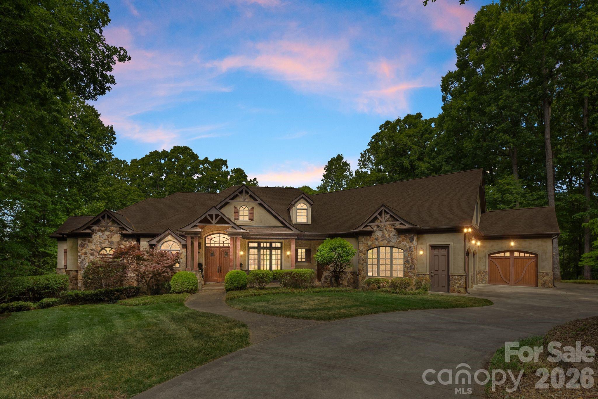 This is not a home you walk into and forget. Reportedly designed by a well-known local architect, this one-of-a-kind custom estate sits on over 2 private, wooded acres with no HOA — where European luxury, rustic grandeur, artisan stonework, and custom convenience lighting converge into something truly extraordinary.
From the moment you enter the exquisite foyer, the architecture commands your attention. Hickory plank flooring, rich custom woodwork, arched doorways, crown molding, and 8' doors set an immediate tone of quality and intention. But it's the ceilings that may be this home's most distinctive architectural signature — no two rooms feel the same. Soaring cathedral peaks with massive rustic king cross beams anchor the great room, while coffered ceilings, tray ceilings, beamed expanses, and wood beam details flow room to room, creating a dynamic, layered experience rarely found at any price point.
The great room is the heart of it all — a floor-to-ceiling stone fireplace, hand-laid and breathtaking in scale, rises as the room's undeniable focal point, framed by a built-in entertainment center that balances grandeur with function. And framed just beyond the windows, long wooded views stretch across the private acreage, bringing the outside in and adding a sense of serenity and seclusion that few homes can offer.
The chef's kitchen is both functional and stunning, and it tells a story in stone. Two distinct stone features define the space: a striking stone arch surround framing the commercial-grade range, and a second stone accent wall that adds depth and unmistakable character. Rustic ceiling beams carry through from the great room, tying the spaces together in warmth. Granite countertops, carved wood accents, a wine refrigerator, double oven, dishwasher, and premium Fisher & Paykel appliances complete a kitchen built for both everyday living and effortless entertaining — all while looking out over a lush, private tree line that makes even a quiet morning feel like a retreat.
Upscale European lighting illuminates Travertine, designer tile, and 5" wide hickory hardwood floors throughout, while 8" baseboards and custom finishes underscore the craftsmanship at every turn. The formal dining room and private office flank the foyer with elegance. The primary en-suite retreat offers a soaking tub, oversized walk-in shower, dual vanities with granite countertops, dual walk-in closets, and a dedicated exercise room — a true spa-like sanctuary within the home. Additional bathrooms continue the theme with custom vanities, granite, and a few will surprise you with hammered copper sinks!  DETAILS!!!
The fully finished lower level expands the home's versatility in spectacular fashion. A purpose-built media room delivers a true theater experience — projector, 6x9 screen, built-in surround sound with in-seat bass, acoustic wall treatments, and custom lighting make every viewing unforgettable. A second full kitchen, living room, large bedroom with full bath, and half bath add incredible flexibility for multi-generational living, long-term guests, or extended stays.
An Elan home system integrates security, audio, and media control throughout and also features Centralite whole-home lighting controls, three-zone HVAC, dual-pane windows, central vacuum, and full cable and ethernet wiring ensure every modern need is met. Built-in speakers extend seamlessly from interior living spaces to the outdoors.
Step outside to a tiled terrace and covered patio both featuring their own fireplacesand let the setting do the rest. Long, sweeping views of mature trees unfold before you, creating an atmosphere of privacy and natural beauty complimented by a fenced in backyard. A built-in gas grill, professional lighting, and in-ground irrigation fed by a private well round out the outdoor living space. Even the garage has been thoughtfully elevated with a tiled dog wash station, because no detail was overlooked.  Your sanctuary awaits!