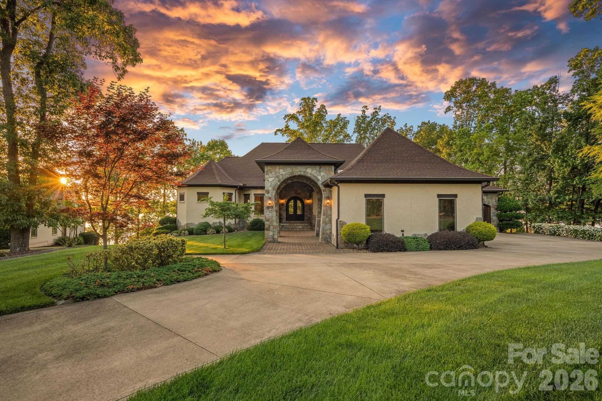 Where luxury meets the water’s edge! This exquisite waterfront retreat on the highly sought-after Brawley School Road peninsula offers the ultimate blend of luxury, craftsmanship, and outdoor living on nearly one acre with almost 200 feet of shoreline and year-round deep water. Perfectly positioned just beyond The Point with easy main channel access, this stunning home captures breathtaking long-range sunset views and lake vistas from almost every room. Designed for both grand entertaining and everyday comfort, the open-concept main living areas showcase exceptional architectural detail including high custom ceilings, beautiful arches, rich wood moldings, custom stair railings, many arched iron-and-glass exterior doors, solid knotty alder interior doors throughout, and walls of custom Andersen windows, many arched, that frame the sparkling waters of Lake Norman. The impressive great room features a striking stone fireplace flanked by wood built-ins with stone arches and a live-edge wood mantel. The chef’s kitchen is beautifully appointed with granite countertops, wood cabinetry, a large island with breakfast bar, decorative range hood, hammered copper sink, premium stainless appliances including a gas cooktop, wall oven and built-in microwave, cabinet-faced refrigerator and dishwasher, plus thoughtful custom storage features throughout. Formal living and dining rooms add elegance, while the spacious lakefront office with fireplace creates an inspiring work-from-home setting. Every bedroom enjoys its own ensuite bath, complemented by powder rooms on both the main and lake levels. The luxurious primary suite features a fireplace, private balcony access, 2 spacious custom walk-in closets, and a stunning bath with a large soaking airtub, walk-in shower room, and 2 beautiful vanities. Multiple indoor fireplaces create warm gathering spaces throughout the home, including the primary suite, office, family room, and great room. Outdoor living is truly exceptional with tiered entertaining spaces designed to embrace the lake lifestyle. Enjoy a massive patio with outdoor kitchen, lakeside terrace with built-in seating and outdoor fireplace, rear balcony and covered terrace, irrigated lawn areas, and a scenic deck/boardwalk overlooking the water. The private pier leads to a covered dock with boat lift, deep-water access, steps into the lake, plus a private beach and paddle sport launch area. Additional luxury features include a home elevator, emergency generator, multizone HVAC systems, cedar garage doors, abundant storage, & a 4-car garage. With no HOA dues and an unmatched combination of privacy, quality, and breathtaking waterfront living, this remarkable Lake Norman property delivers an extraordinary lifestyle both inside and out.