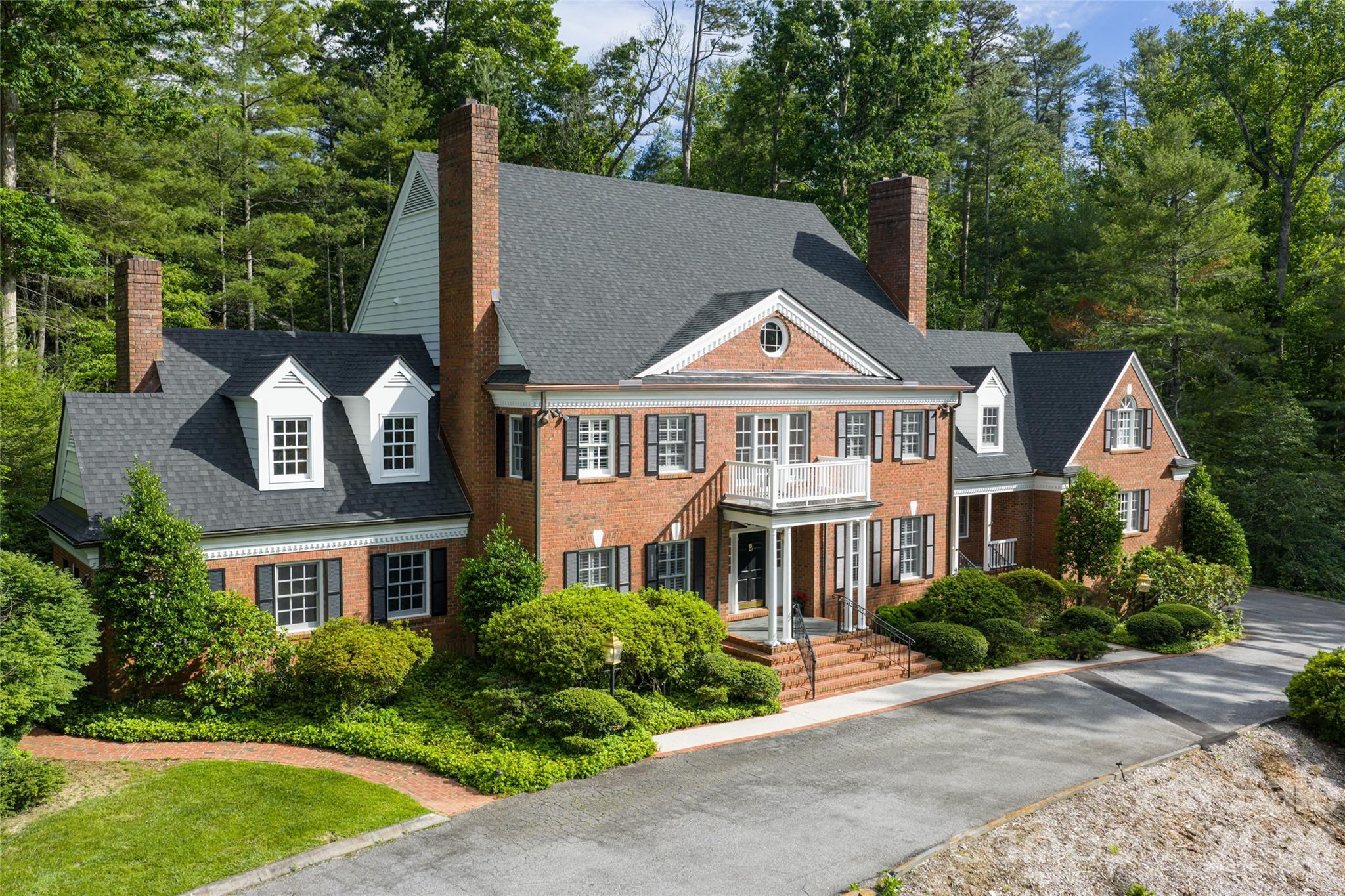 Enter inside and be captivated by this timeless traditional estate in the heart of Biltmore Forest. From the moment you enter, exquisite craftsmanship and high-end finishes set the tone, including detailed wainscoting, crown molding, oak paneling and beams, plantation shutters and solid wood doors throughout. The inviting foyer opens to a beautifully designed three-story home featuring a luxurious primary suite wing and elevator access to all levels. Entertain effortlessly in the formal living and dining rooms or gather in the warm and inviting oak-paneled den, complete with a fireplace, wet bar and mini refrigerator. A refined library/study provides the perfect space for working from home or relaxing with a favorite book. The spacious chef’s kitchen is thoughtfully appointed with granite countertops, premium stainless steel appliances and a Dacor six-burner gas range with double ovens and a warming drawer. A massive walk-in pantry off the breakfast room offers exceptional storage and organization. Designed for both comfort and functionality, the home offers abundant storage throughout, as well as a large basement ideal for recreation, hobbies or additional living space. The expansive primary wing serves as a private retreat, featuring a generous bedroom and sitting room with a fireplace, dual baths, a dressing area and multiple walk-in closets. Set on 3.6 acres, this remarkable property is one of the largest estates in Biltmore Forest, offering a creek, wooded surroundings, a private patio and a level backyard. All of this is conveniently located just minutes from Biltmore Village, downtown Asheville and the River Arts District.