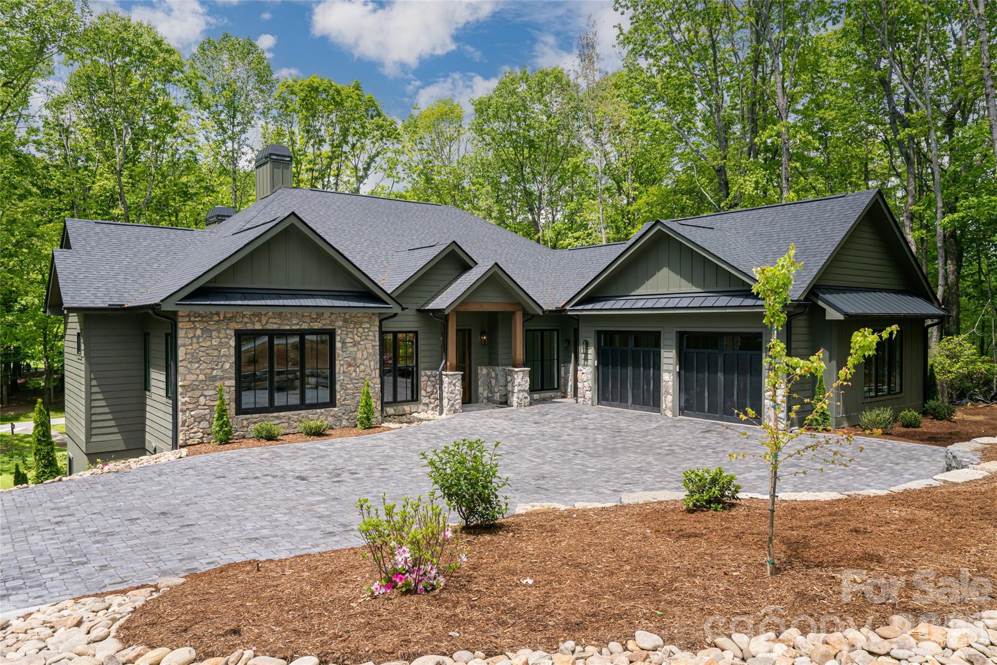 Perfectly positioned overlooking the 7th tee at Champion Hills — one of Western North Carolina's most coveted private golf communities — this newly constructed luxury residence offers a rare opportunity to live within a world-class Tom Fazio-designed course community while enjoying all the charm and convenience of downtown Hendersonville just minutes away.

Spanning more than 4,800 square feet, the home was thoughtfully designed for both daily comfort and elevated entertaining, with four bedrooms, a dedicated office, flexible bonus space, and a fully appointed lower-level recreation room. From the moment of arrival, intention and quality are unmistakable — a stately paver driveway, curated landscaping, and an architectural presence that announces something exceptional within.
Inside, wide-plank white oak flooring flows throughout the main living spaces, anchored by 10-foot ceilings, bespoke designer lighting, and an oversized wood-burning fireplace that brings warmth and permanence to the heart of the home. The open-concept layout connects living, dining, and kitchen seamlessly, with walls of windows framing unobstructed golf course views.

The kitchen is both a culinary showpiece and an entertainer's command center — anchored by a dramatic island wrapped in Taj Mahal quartzite and equipped with a full Thermador appliance package, including a 48-inch professional gas range. A dedicated scullery and oversized walk-in pantry keep the kitchen surface pristine while providing serious prep infrastructure behind the scenes.

The main-level primary suite is a study in considered luxury: marble tile floors and shower surrounds, a freestanding soaking tub, dual vanity, oversized walk-in shower, and a custom walk-in closet designed for wardrobe and ease. A beautifully finished mudroom with built-in cabinetry and marble flooring, a main-level guest suite, and a covered outdoor living area with Trex decking and a second wood-burning fireplace complete the main level — all oriented toward the course and the mountain air.

Below, the lower level was purpose-built for hosting: a generous entertainment room with a custom wet bar, designer lighting, prep sink, ice machine, and beverage cooler creates a space that rivals any private club lounge. An oversized two-car garage and dedicated golf cart garage round out the functionality.

Life at Champion Hills extends well beyond the home itself. Residents enjoy exclusive access to the Tom Fazio championship golf course, a full-service clubhouse with dining, fitness center, tennis, pickleball, hiking trails, and a vibrant year-round social calendar — all within a gated mountain setting that defines the Western North Carolina luxury lifestyle. When adventure calls beyond the gates, Hendersonville's celebrated Main Street is minutes away, offering acclaimed dining, craft breweries, boutique shopping, a thriving arts scene, and premier healthcare — all set against the backdrop of the Blue Ridge Mountains.

This is new construction luxury mountain living at its finest — where championship golf, refined finishes, and community culture converge in one of Hendersonville, NC's most distinguished addresses. Agent is part owner.