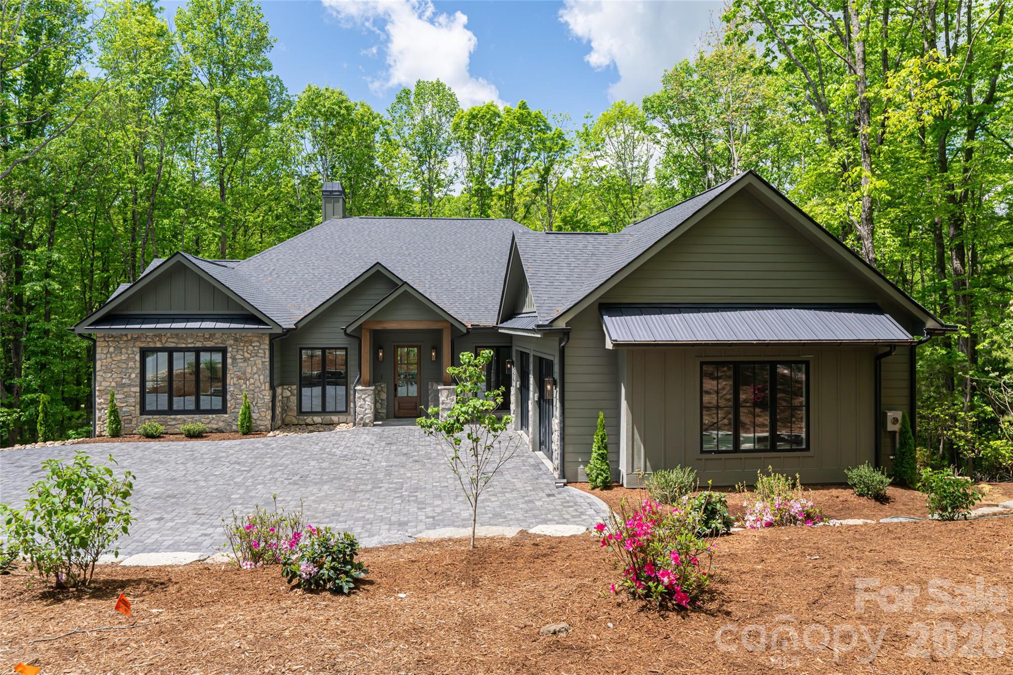 Perfectly positioned overlooking the 7th tee at Champion Hills — one of Western North Carolina's most coveted private golf communities — this newly constructed luxury residence offers a rare opportunity to live within a world-class Tom Fazio-designed course community while enjoying all the charm and convenience of downtown Hendersonville just minutes away.

Spanning more than 4,800 square feet, the home was thoughtfully designed for both daily comfort and elevated entertaining, with four bedrooms, a dedicated office, flexible bonus space, and a fully appointed lower-level recreation room. From the moment of arrival, intention and quality are unmistakable — a stately paver driveway, curated landscaping, and an architectural presence that announces something exceptional within.
Inside, wide-plank white oak flooring flows throughout the main living spaces, anchored by 10-foot ceilings, bespoke designer lighting, and an oversized wood-burning fireplace that brings warmth and permanence to the heart of the home. The open-concept layout connects living, dining, and kitchen seamlessly, with walls of windows framing unobstructed golf course views.

The kitchen is both a culinary showpiece and an entertainer's command center — anchored by a dramatic island wrapped in Taj Mahal quartzite and equipped with a full Thermador appliance package, including a 48-inch professional gas range. A dedicated scullery and oversized walk-in pantry keep the kitchen surface pristine while providing serious prep infrastructure behind the scenes.

The main-level primary suite is a study in considered luxury: marble tile floors and shower surrounds, a freestanding soaking tub, dual vanity, oversized walk-in shower, and a custom walk-in closet designed for wardrobe and ease. A beautifully finished mudroom with built-in cabinetry and marble flooring, a main-level guest suite, and a covered outdoor living area with Trex decking and a second wood-burning fireplace complete the main level — all oriented toward the course and the mountain air.

Below, the lower level was purpose-built for hosting: a generous entertainment room with a custom wet bar, designer lighting, prep sink, ice machine, and beverage cooler creates a space that rivals any private club lounge. An oversized two-car garage and dedicated golf cart garage round out the functionality.

Life at Champion Hills extends well beyond the home itself. Residents enjoy exclusive access to the Tom Fazio championship golf course, a full-service clubhouse with dining, fitness center, tennis, pickleball, hiking trails, and a vibrant year-round social calendar — all within a gated mountain setting that defines the Western North Carolina luxury lifestyle. When adventure calls beyond the gates, Hendersonville's celebrated Main Street is minutes away, offering acclaimed dining, craft breweries, boutique shopping, a thriving arts scene, and premier healthcare — all set against the backdrop of the Blue Ridge Mountains.

This is new construction luxury mountain living at its finest — where championship golf, refined finishes, and community culture converge in one of Hendersonville, NC's most distinguished addresses. Agent is part owner.