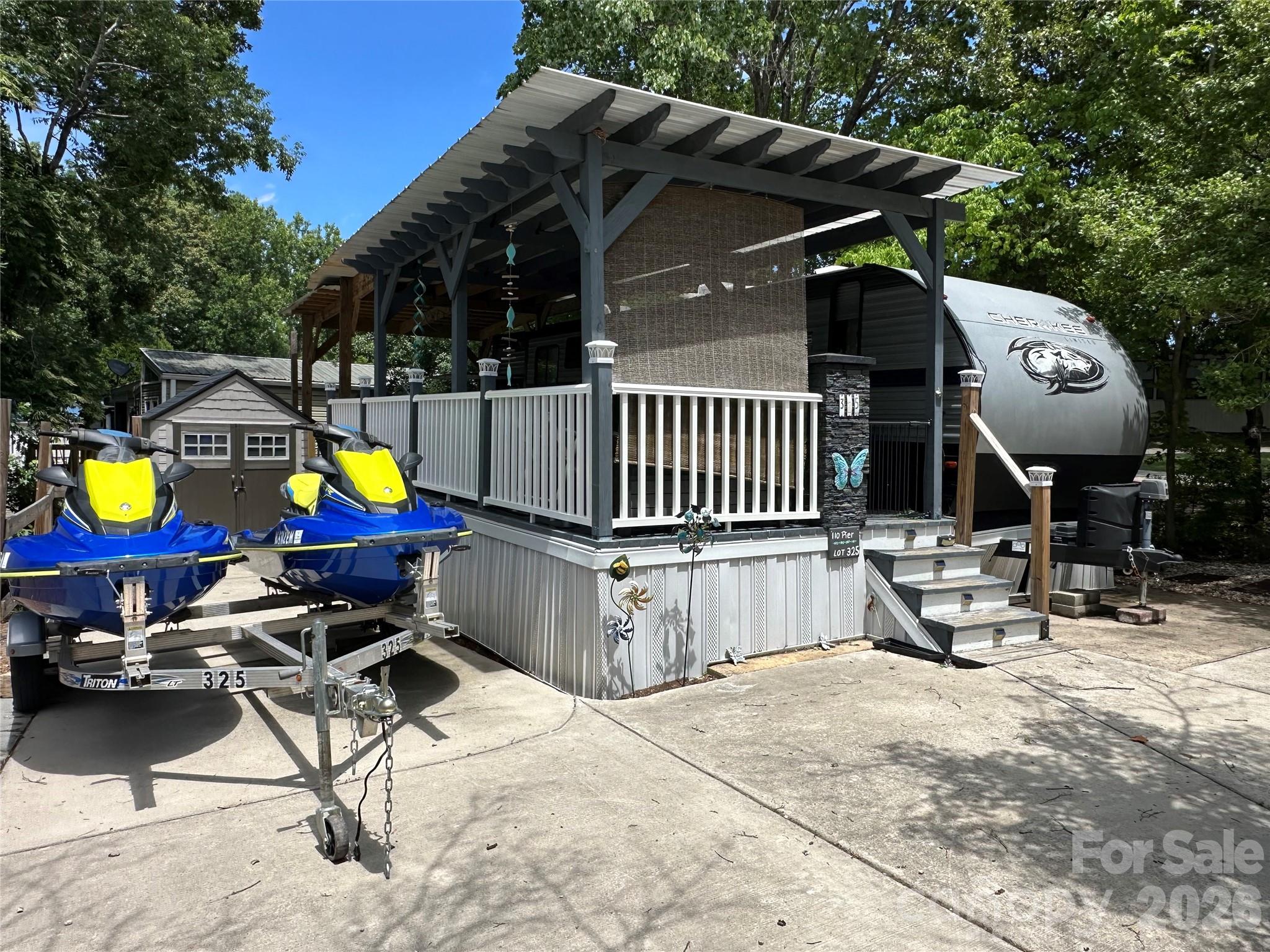 This 2020 Cherokee 2-bedroom bunkhouse camper is permanently set up on a deeded lot in the gated waterfront community of Badin Shores Resort at Badin Lake. The concrete parking area provides easy maintenance and abundant space for your boat, jet skis, golf cart, and multiple vehicles. Inside, you'll find a bright, modern interior featuring a center kitchen island, a recently updated household-style refrigerator, microwave, propane stove, and a spacious pantry for added storage. The primary bedroom offers an ensuite-style bath with a spacious corner shower and convenient access from both the bedroom and hallway. The private bunkroom comfortably sleeps up to four, and all mattresses have been upgraded to household memory foam mattresses for exceptional comfort. Step outside to enjoy the covered deck designed for entertaining, complete with an outdoor kitchen featuring a pull-out gas grill, sink, and small refrigerator—perfect for relaxing after a day on the lake.