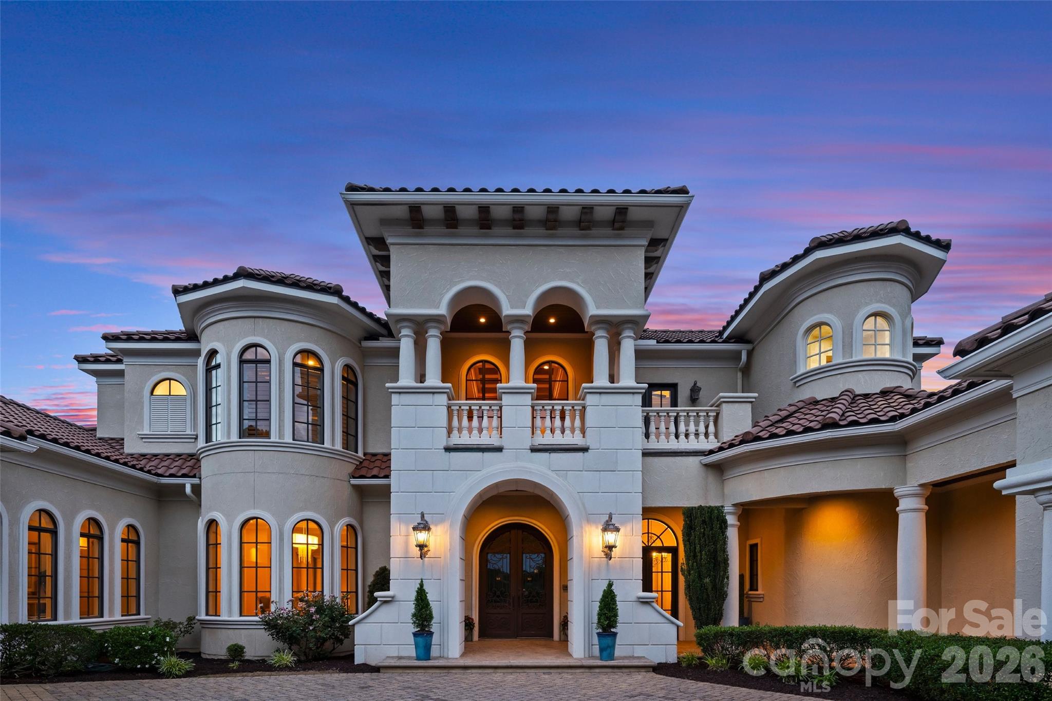 Nestled along the shores of Lake Norman, this extraordinary Mediterranean-inspired waterfront estate blends timeless architecture with resort-style living across 10,320 square feet of luxurious interior space. Situated on approximately 1.35 private waterfront acres, the residence offers six bedrooms, six full bathrooms, three half bathrooms, and elevator access to all three levels of the home. Designed for both grand-scale entertaining and everyday luxury, the estate showcases exceptional craftsmanship, dramatic architectural detailing, and breathtaking indoor-outdoor living throughout. Soaring ceilings, extensive custom millwork, sweeping archways, intricate ceiling treatments, rich hardwood flooring, tile and walls of windows create an atmosphere of elegance and sophistication while capturing stunning water views from nearly every vantage point. Additional luxury amenities include a wine room a five-car garage, three wet bars, two laundry rooms, a state-of-the-art media room, main floor generator and an expansive club-style recreation room designed for entertaining on every level. The outdoor living experience is equally impressive, highlighted by a hotel-sized covered veranda complete with its own wet bar and outdoor fireplace, creating the ultimate setting for year-round waterfront enjoyment. The luxurious primary suite serves as a private retreat featuring a spacious sitting area, spa-inspired bath with elevated soaking tub, boutique-style dressing room, oversized custom closets, and serene waterfront views. Secondary bedroom suites continue the home’s architectural elegance with custom details, arched windows, and beautiful natural light.
Designed to rival a private resort, the outdoor living experience is truly unforgettable. Expansive covered verandas feature dramatic wood-paneled ceilings, a stone fireplace, outdoor dining and lounge spaces, and lake views. Resort-inspired grounds include a basketball court multiple terraces, manicured lawns, a custom freeform pool and spa, and a spectacular cascading waterfall feature flowing from the upper pool into a lower plunge pool. A rare offering combining architectural significance, resort-caliber amenities, and exceptional waterfront living.