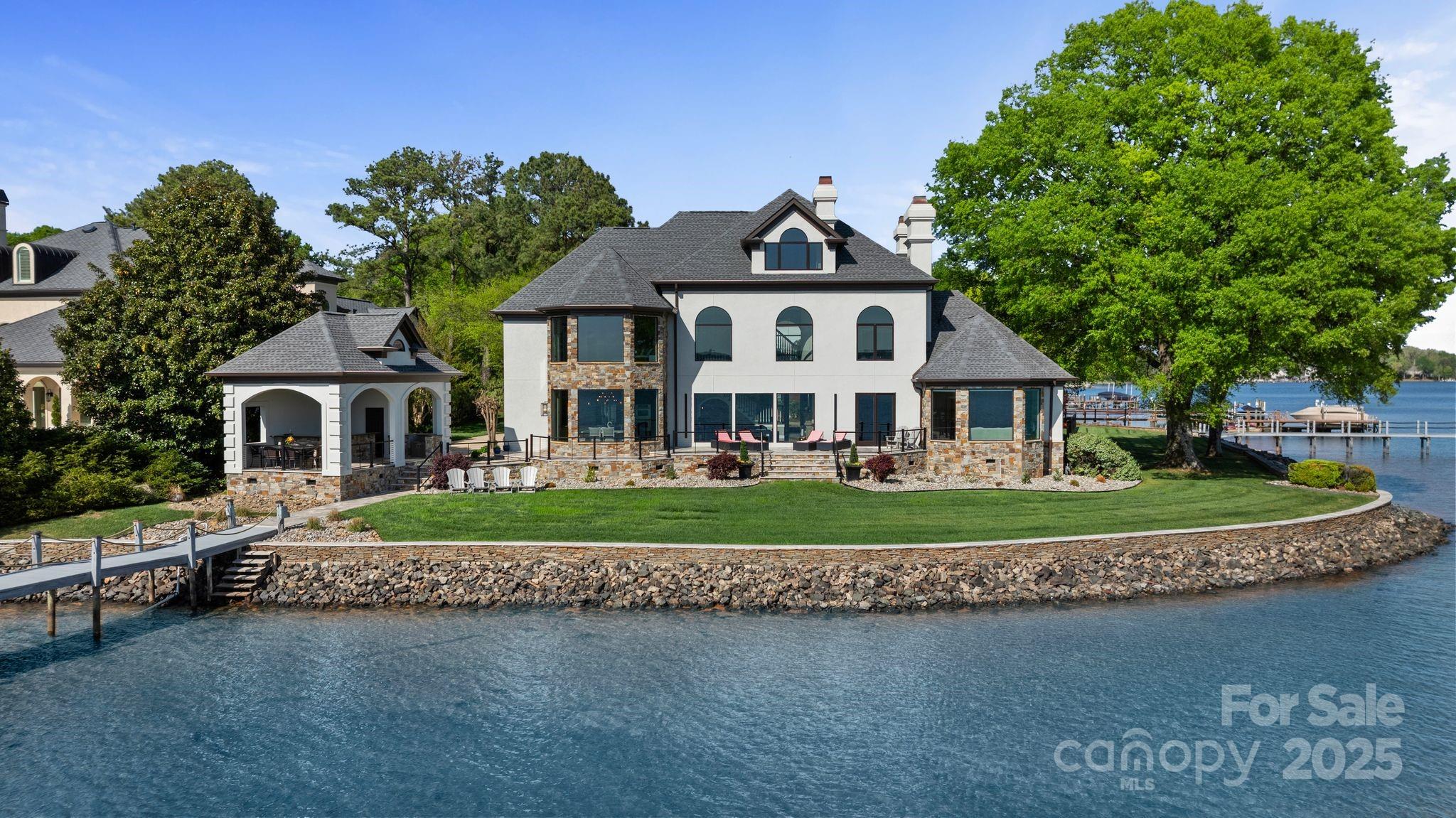 Nestled within the prestigious gated community of Alexander Island, this waterfront estate offers unparalleled luxury & breathtaking sunset views of Lake Norman. AMAZING value, priced far below appraisal. Grand foyer that opens into a 2-story great room, showcasing expansive views of the lake. Bright and open main level with primary suite. The upper level boasts a second primary suite, 3 additional bedrooms, 4.5 baths & a versatile media/bonus room. Top floor offers a loft, full bath, & an additional bed/bonus room. Outdoor amenities include an expansive terrace, newly updated outdoor kitchen, dining area, & half bath, perfect for entertaining. Enjoy over 4 miles of stunning sunset views and proximity to Langtree's dining & lifestyle offerings. This property also features a stationary dock with boat lift. Alexander Island is a private gated community with tree-lined streets, minutes to Langtree w/easy access to Hwy 77. Priced below appraisal! Make this your lakefront paradise!