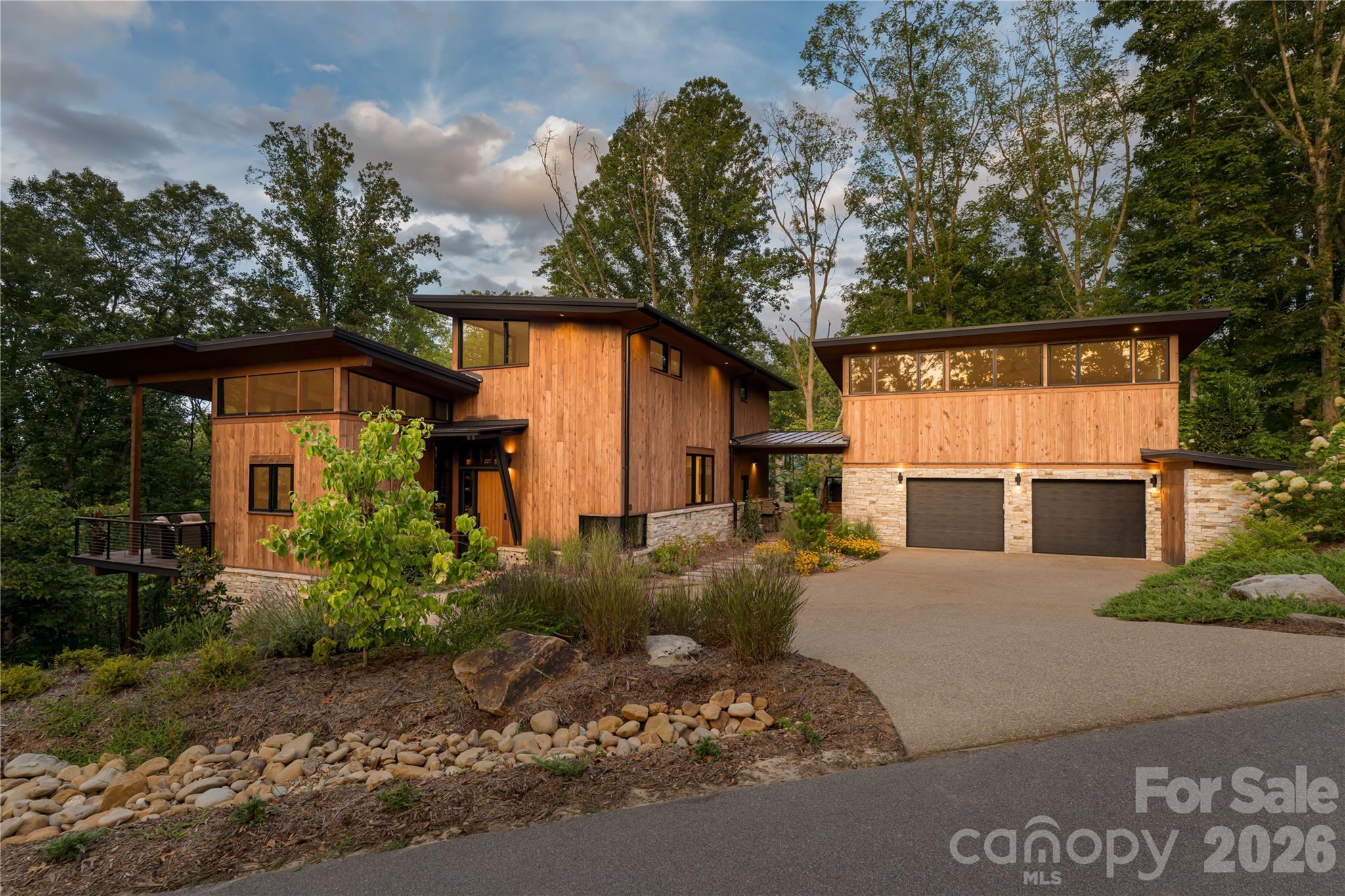 Tucked into the trees in the sought-after community of Olivette, this custom mountain modern home by Jade Mountain Builders is a seamless blend of architectural design, craftsmanship, smart technology and natural beauty.

Striking rooflines, warm wood siding, stacked stone accents, and dramatic walls of glass create a bold architectural statement. Inside, refined finishes and intentional details define every space.

The main living area is framed by expansive windows that capture the surrounding forest, filling the home with light and an ever-present connection to nature. In the winter months, enjoy views and sounds of the French Broad River shimmering through the trees—a rare and peaceful seasonal bonus. A stunning custom built-in shelving wall anchors the space, offering both artistry and function.

The chef’s kitchen is a modern showpiece—sleek black cabinetry, rich wood accents, exposed beams, and polished concrete floors with radiant heat for added comfort. A generous island invites gathering and conversation, blending sophistication with warmth in true mountain modern style.

Above the garage, a full luxury studio apartment offers exceptional flexibility—perfect for guests, extended family/in-law suite, rental income, or a private home office. Thoughtfully designed and beautifully finished, it mirrors the quality and aesthetic of the main residence.

Outdoor living is equally compelling, with covered terraces and elevated balconies designed to immerse you in the peaceful wooded setting. Or enjoy hanging out in the backyard down by the firepit. There is also a fenced in side yard for your 4-legged companion animal.

And then there’s Olivette.

Set along the French Broad River, this one-of-a-kind community offers river frontage, vineyards, a working community farm, miles of walking and biking trails, a dog park, and acres of preserved green space. Just minutes from Asheville, yet worlds away, Olivette is known for its architectural integrity, sustainability, and vibrant sense of community.

This is more than a home.
It’s refined mountain living.

Furnishings are negotiable.