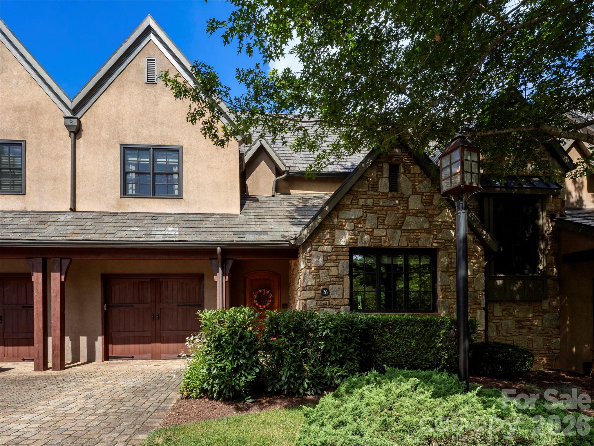 Situated within the gates of The Cliffs at Walnut Cove, this refined townhouse at 26 Village Oak Drive features an expansive 3,863 square feet of impeccably designed interior living space distributed across three beautifully finished levels. A private residential elevator connects all three floors, opening onto a main level designed for smooth transitions between daily living and upscale entertaining. The central living room features a coffered ceiling with custom inset panels and a folding glass wall system that slides open to an elevated, screened balcony. This space flows directly into a kitchen equipped with a functional centerpiece island and breakfast bar, which sits adjacent to a dramatic formal dining room defined by a double-height vaulted ceiling, heavy accent molding, and a prominent floor-to-ceiling fireplace. A main-level guest bedroom suite, an attached garage, and a full bathroom complete this floor's highly accessible layout.

The upper level serves as a private primary sanctuary, hosting an expansive bedroom with its own viewing balcony and bathroom featuring a deep soaking tub and separate walk-in shower. This upper floor also includes a large walk-in wardrobe and laundry area, alongside a flexible bonus room perfect for an executive office or media den. Below, the walk-out lower level is configured for leisure or guest privacy, centered around a spacious family room with a fully equipped wet bar and premium cabinetry. French doors open from the family room to a beautifully paved courtyard patio that captures sweeping views of the surrounding lush greenery and rolling mountain ridges, creating an idyllic backdrop for outdoor relaxation. This level also accommodates an additional private bedroom, a versatile den, a full bathroom, a separate laundry/utility room, and two storage closets. Combining upscale architectural design, multi-generational flexibility, and lock-and-leave convenience, this townhouse represents the pinnacle of premium mountain living.

With a Membership at The Cliffs, residents of Walnut Cove enjoy access to a world-class lifestyle centered around an 18,000-square-foot wellness center featuring indoor and outdoor pools, tennis courts, and a luxury spa. The community's crown jewel is the Jack Nicklaus signature golf course, which is complemented by an award-winning clubhouse and "The Tavern," a social hub for fine dining and member events. Bordering the Pisgah National Forest and located just minutes from the Blue Ridge Parkway and Asheville, The Cliffs at Walnut Cove offers a rare combination of high-altitude privacy and convenient access to premier cultural and recreational amenities. This magnificent property represents the absolute pinnacle of luxury mountain living.