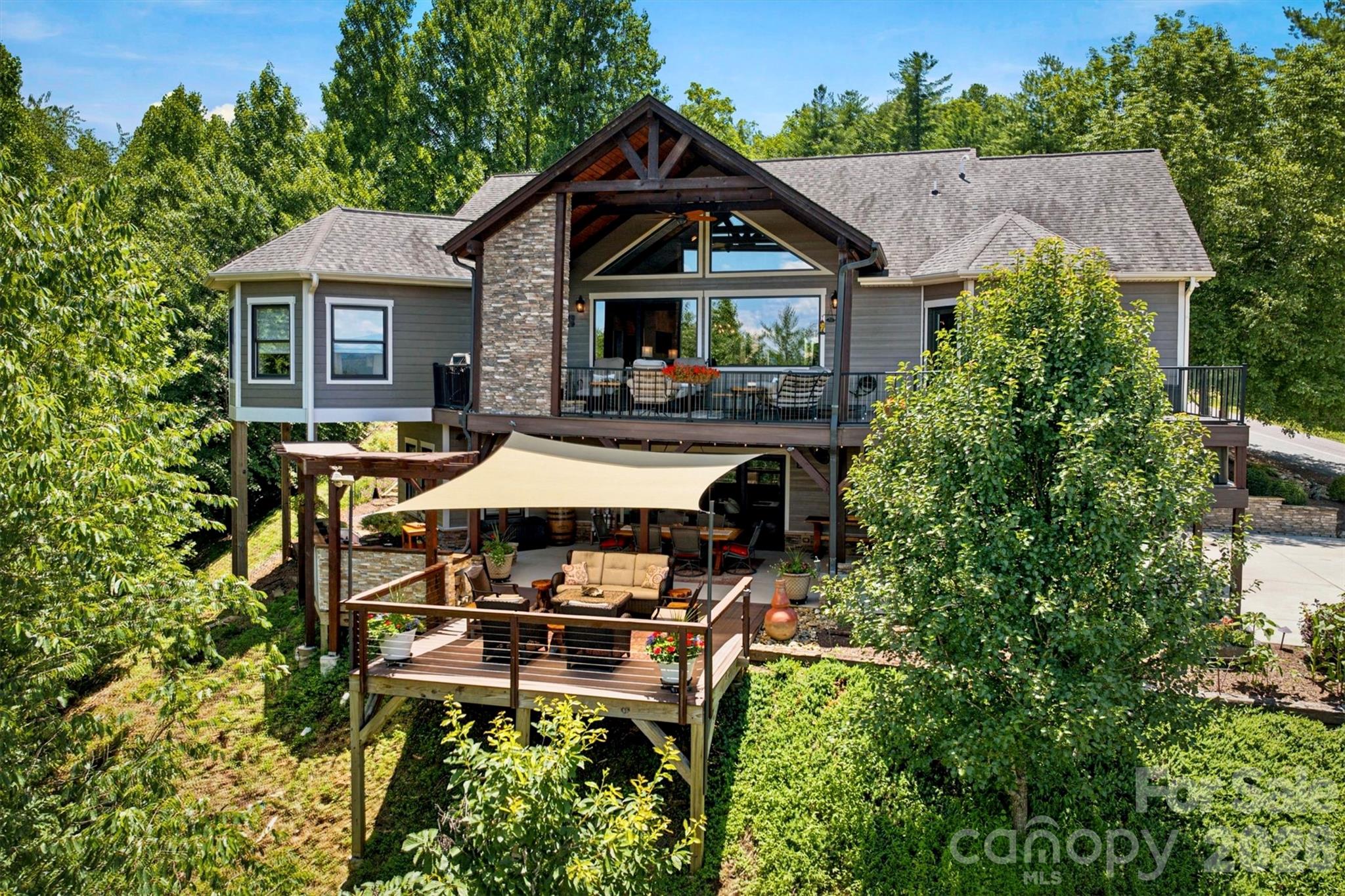 Perched above the landscape, this custom mountain retreat at The Coves Mountain River sits on 1.6 acres, perfectly balanced with natural beauty and elevated living. 
An inviting flagstone front porch and double mahogany doors welcome you to a spacious foyer with cedar vaulted ceiling.  Past the formal dining area is the great room, where floor-to-ceiling windows showcase dramatic multi-layered mountain views. Natural light balances warm rich tones of red oak floors, distinctive wood framing, and a stone fireplace with 100-year-old hand-hewn wood mantel.  In the Chef’s kitchen, luxury, organization, and functionality are maximized.  Timeless, hard maple cabinets offer abundant storage.  Warm under-cabinet lighting illuminates the workspace and highlights elegant granite surfaces below.   An 8 ft island is the central hub, with granite countertop and dedicated bar seating.  The kitchen is equipped with premium Thermodor appliances: 5 burner gas stove, wall oven microwave combo, and dishwasher.  A beverage fridge keeps your favorite drinks perfectly chilled and easily accessible.  A custom-designed walk-in pantry provides immense organizational storage space.  Flowing from the main kitchen is a striking, half-octagon keeping room. Dramatic wrap-around windows create a bright inviting gathering spot or quiet place to start your day.  Step out to the stunning back porch, with low-maintenance composite decking underfoot, and above, a vaulted wood ceiling peaks with dramatic cross-beams. This outdoor living room is warmed by a magnificent stone fireplace with hand-hewn reclaimed wood mantel; the perfect spot to savor a cup of coffee as the morning mist lifts from the river valley below or warm your cheeks and toes after an autumn hike.  The ensuite primary bedroom combines architectural elegance and ultimate relaxation.  Tray ceilings add height and a touch of modern luxury. Oversized windows and a full glass door bring stunning mountain scenery into your room.  An open-air hot tub is just outside, ideally positioned for mountain tranquility and unobstructed star-gazing.  
The luxurious bathroom and dressing room are a spa-sanctuary: dual vanities with rich wood cabinetry, walk-in rainfall shower with built-in bench, large soaking tub, and a fully tailored dressing room-closet, complete with floor-to-ceiling shelving, drawers, integrated shoe racks, and dedicated long-hanging sections to maximize every inch of space.
Seamless indoor-outdoor spaces, and more are on the lower level. The cozy den has a stone fireplace and a custom bar crafted of natural woods and stacked stone, evoking the feel of a private mountain tavern.  Behind a handcrafted barn door is the office/craft room with floating shelves. An expansive outdoor kitchen made of stacked stone, stained concrete countertops, and a handsome pergola is fully integrated with the deck, making it perfect for grilling, and serving.  A warm natural wood light fixture creates a striking focal point over the outdoor dining table.  The lower outdoor living area is completed with a large deck sitting area, topped with a shade sail.  2 spacious guest bedrooms and a luxury guest bathroom are also on the lower level, as well as a large work-shop/room and fitness room.  The main-level 2 car garage features a professional epoxy floor and built in storage shelves.  Just inside is a convenient drop-zone with live-edge wood bench, coat hooks, and shelves with storage baskets.   Impeccable mature landscaping surrounds this dream mountain home. The Coves Mountain River Club is a 3,200 acre gated community on Johns River. Amenities: trail system, river access areas, picnic pavilions. 2 Equestrian Centers. Community Garden. Vineyard. Dog Park. Mountain-top clubhouse, pool, fitness center and more! 500K acre Pisgah National Forest and Wilson Creek River Area are across the road! 1.25 hour drive to Charlotte/Asheville, minutes to Lenoir, Blowing Rock, Morganton, and Blue Ridge Parkway.