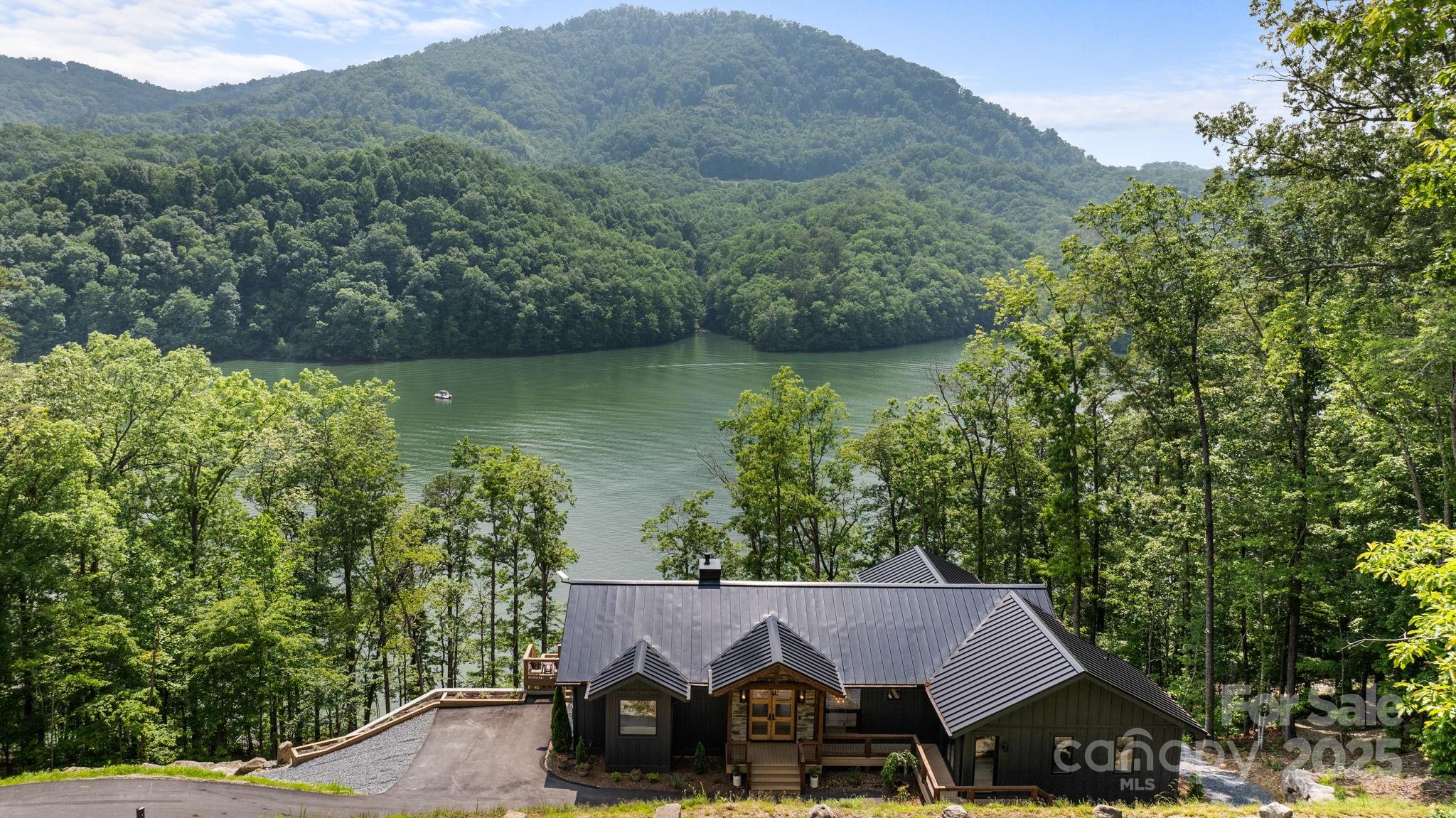 Nestled in the Great Smoky Mountains, Fontana Lake Estates is a premier gated lakefront community where nature & adventure thrive. This stunning approx. 3,791 sq ft, 5-bed, 3.5-bath mountain modern home blends rustic charm w/ modern design. Built for longevity, it features a poured concrete foundation, standing seam metal roof, & Hardie plank siding. Inside, find hardwood floors, cathedral ceilings, quartzite & leathered granite countertops, custom cabinetry, & a spacious butler’s pantry. The primary suite boasts a coffee bar, custom closet, & spa-like bath. A bonus flex space is perfect for a studio. An approx. 374 sq ft workshop is accessible from the lower level exterior. A TimberTech deck offers breathtaking lake & mountain views, w/ a gently sloped path to a private dock w/ water & power. Community amenities include paved roads, a boat launch, scenic trails, & more. Nearby, Cherokee, Bryson City & the Nantahala Outdoor Center offer rafting, hiking, & dining. Adventure awaits!