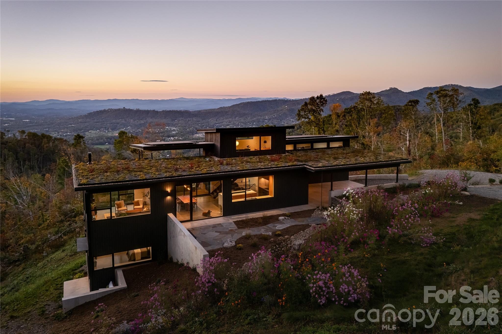 Stunning winner of 2025 Parade of Homes Gold Awards for Craftsmanship and Green Certification perched above the Reems Creek Valley and adjacent to its headwaters - 310 acres protected through a conservation easement with Southern Appalachian Highlands Conservancy. Expansive glass and natural materials seamlessly connect this home to the surrounding forest and distant mountain views. A restrained palette of concrete & steel, charred cypress, white oak & black walnut, and consistent, minimalist details allow nature to be the focal point. Enter through the sunken patio garden into the heart of the home under a 2,000sf living roof. An open floor plan spans the inviting glass-lined living room, a gracious central dining area, and flows through a 16ft wide opening to the covered porch with panoramic mountain sunsets. The stunning sunrise-kissed kitchen inspires culinary creativity with warm wood tones & clean quartzite countertops paired with the finest Fisher & Paykel integrated appliances, the perfect pantry, and a baker's nook. The primary bedroom boasts some of the best views in the house. Enjoy an elevated en-suite bath with quarter sawn oak cabinetry, a handmade tile & frameless glass shower, and a well appointed walk-in closet. An upper level office provides a close, yet secluded workspace with astounding long range & forest views. Downstairs is centered on a sumptuous media lounge that's open to a covered patio and big beautiful views. Two bedrooms flex into one shared space with a retractable wall. The game & fitness room works for anything, including a large fourth bedroom. And there's a secure & conditioned 6x12 wine cellar. Back on main, an oversized carport lends access to a conditioned workshop/studio space that can easily connect for an expanded primary suite. Minimalism has been maximized with a conscious curation of exactly what one needs. Sustainability & efficiency abound as this home earns the record highest GreenBuilt Platinum Level Net Zero and Regenerative certifications in NC. A 15.79 kW solar system with 15 kW of battery storage keeps the power on even if grid is down. Comfort & healthy indoor air quality are certain with 2 geothermal heat pumps providing radiant floor heat, ducted cooling, and whole house ventilation & dehumidification. Ask for attached specifications, floor plans, awards & certifications. This place embodies intentional design, award winning craftsmanship and green building techniques, and an eco-conscious, luxury lifestyle. Three other adjacent lots that all support symbiotic privacy and significant additional acreage available. Inquire for details.