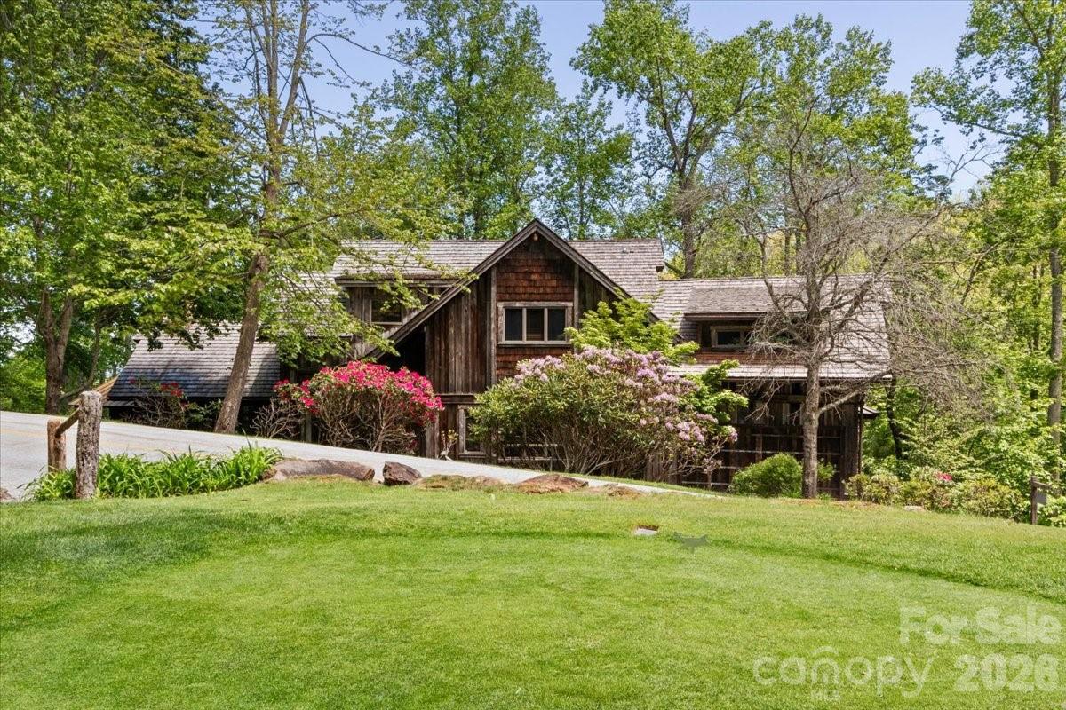 Nestled in the bucolic Mountain Air Country Club community on Spring House Drive, this custom-designed mountain estate provides a spacious, luxury home on a large, forested property. The exterior features reclaimed barnwood and a cedar shake roof. The interior provides more than 5,500 square feet of classic, mountain elegance for family gathering and entertaining. Rich woodwork is everywhere, including the cathedral ceilings in the great room and the upstairs bedrooms. There are custom, wood mantles over stone fireplaces, handcrafted accents, and mixed hardwood floors throughout. The open floor plan main living area flows seamlessly from a great stone fireplace to the spacious dining area, featuring a unique table that seats 14, and on into a chef's kitchen with abundant custom cabinetry and thoughtfully designed conveniences at every turn. Outdoor decks are accessible on all three levels and provide over 2400 square feet of space to relax, entertain, and enjoy the mountain beauty and the sound of the stream running along the property. The expansive main-level deck includes a seating area around a cozy gas-log fireplace for year-round enjoyment. The private primary suite on the upper level includes a bonus room that is currently used as an office/den. Additional guest suites include one on the main floor, and 2/3 on the lower floor, each with direct outside deck access plus a common gathering room with a stone fireplace. There is a spacious, two-car garage and abundant guest parking. This home offers a generator and a central alarm system. The entire property is approximately 3.24 acres, including the original lots 106 & 107 and the adjoining lot 108, to provide enhanced privacy and the potential to enhance long-range mountain views. Furniture and furnishings are included, except for the seller's personal items. A list of exceptions to be provided.