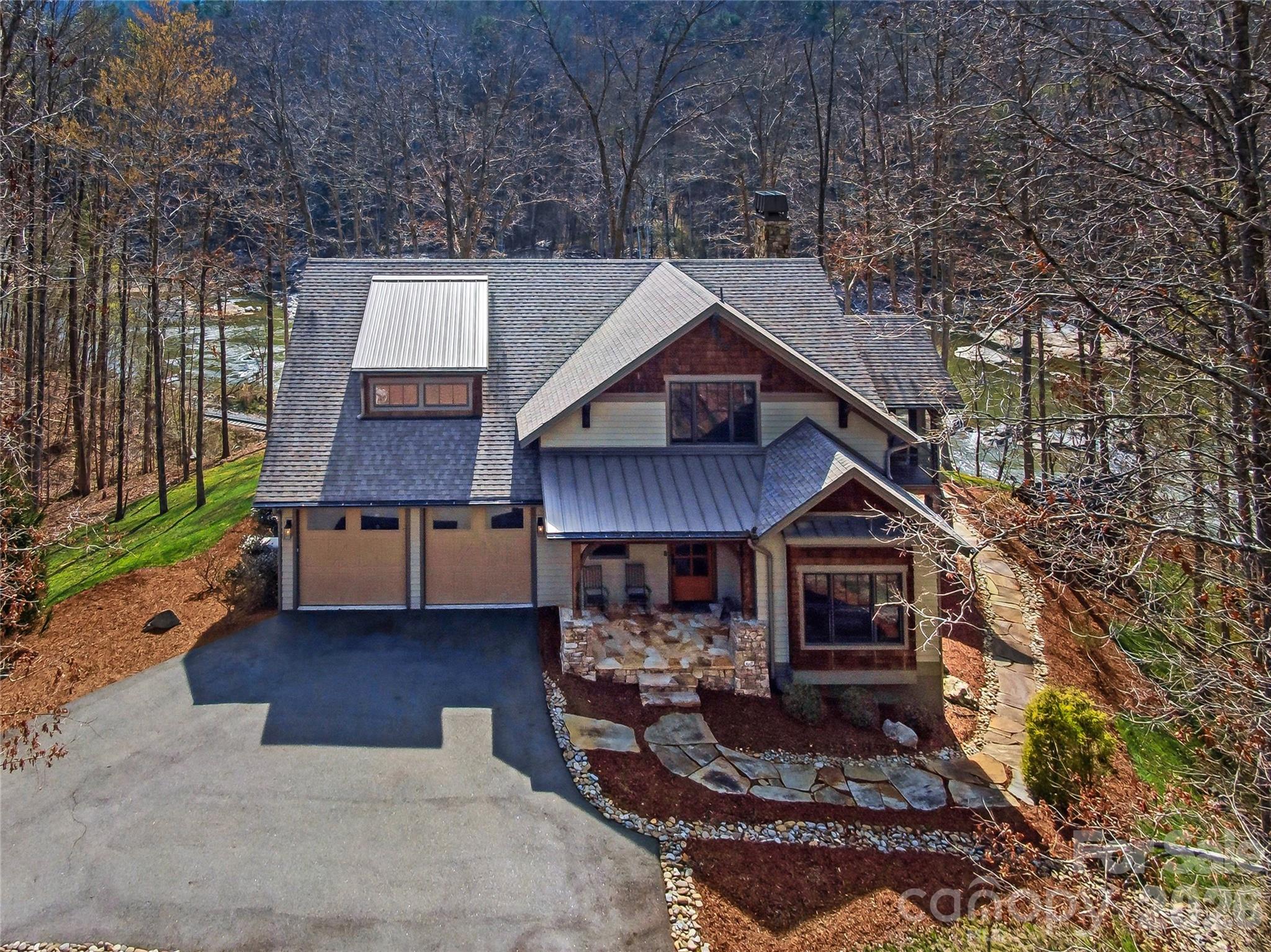 Do you ever dream about waking up to the sound of water flowing over rocks below and sinking into your pillow at night with the windows open? There isn't a better sound of music than nature's. Rise and shine with pure relaxation while savoring that morning cup of coffee riverside. Tucked away in the gated conservation community of French Broad Crossing, 3735 French Broad Parkway is a stunning riverside sanctuary offering a living experience that is second to none. This retreat is perfect for daily living or a second-home all while enjoying an elevated mountain experience. Situated on a large flat lot and being the closest home to the French Broad River in the community, this stunner offers thoughtful design and features that await your arrival. This home was built by Livingstone Design + Build with aging in place standards such as zero-grade entry into the home and showers, the practical placement of outlets, and wide door openings. The primary ensuite is on the main level offering a relaxing ambience with dual vanities, large walk-in shower, water closet, and heated floors. There are also two additional bedrooms and a bathroom on this level. The open concept living area with a chef's kitchen is well-appointed with views of the mountains and river below flowing seamlessly with elevated outdoor living. A screened porch with a wood burning fireplace  and heaters along with an open deck for taking in the stunning views or relaxing in the shade await your arrival. There isn't a better place to unwind or entertain after a day of hiking or rafting! As the heart of the home, the kitchen features granite countertops, stunning cabinetry, open wood and granite island, breakfast bar, and large walk-in pantry. The great room has soaring ceilings, built-ins and a beautiful wood burning fireplace which also allows for a gas log system. This serene space flows with a beat of luxury, yet it's cozy and comfortable. The mudroom off of the garage has ample space to unload after a day in nature. If your adventure has been on the river, step into the private outdoor shower to wash away all that should stay outside! The upper level features a bedroom/bonus room with an en-suite bathroom that serves well as a bunk and game room! Storage is not an issue as there's a huge climate controlled walk-in storage area as well as open ceiling storage the whole length of the garage. This home delivers on functionality without compromise and also includes a Kohler 20kw generator with remote access, security system, and hard-wired cameras for peace of mind. Elaborate neighborhood amenities are all added luxuries that add to the appeal of life in French Broad Crossing. Asheville, Marshall, Hot Springs, and Weaverville are all in close proximity for dining and entertaining adventures as well as providing easy access to life's necessities. After a long day of exploring the hiking/ATV trails right out your door, relax at your personal safe haven in French Broad Crossing. Enjoy evenings at the lodge, by the pool, or riverside. The choice is yours! French Broad Crossing is the ideal outdoor playground to take you away from the daily hustle and bustle. Breathe easy.