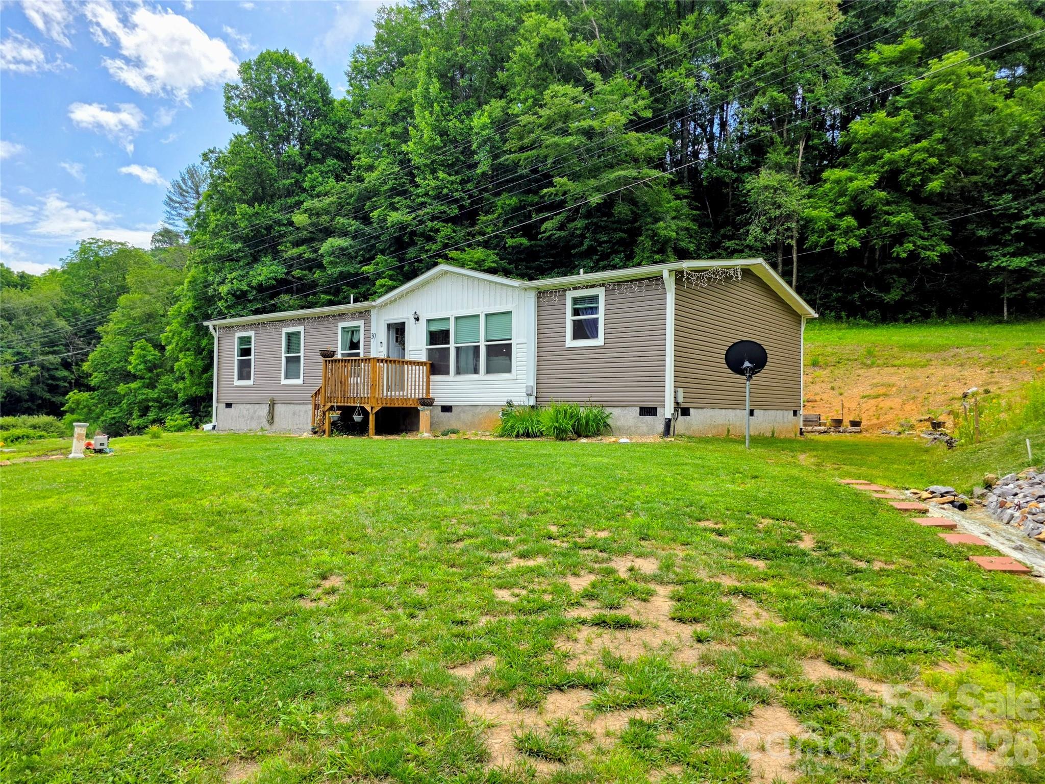 This beautiful 3-bedroom Oakwood modular is only 2 years old and looks and feels like a new home. All of the work has already been done, saving the costs of grading, septic, well and driveway. This house has 2.94 acres of mostly wooded land and has a small spring-fed stream originating on the property. The split bedroom floor plan is built around a large open central space encompassing the kitchen, living room and dining area. The kitchen has a large island that provides lots of food prep space and can be used for casual dining. This energy efficient house is already solar ready. The tankless water heater comes with a programmable heat pump assist saving money on utility bills. The kitchen has a walk-in pantry with a sliding barn door and a handy coffee nook. The floor covering throughout the house is durable luxury vinyl planking. The primary bedroom is roomy and has a walk-in closet. The ensuite bathroom has a large soaker tub and a walk-in shower with subway tiled walls. Both the ensuite bathroom and the guest bathroom feature double sinks. The sellers have completed quite a bit of the lawn work with flowers and shrubs already established. There is a large 12 ft x 20 ft utility building with a garage door located on the western end of the property. This utility building provides plenty of room for storage and shop space. The location of this home is perfect for the buyer who travels frequently to Asheville for work or entertainment. Asheville is a short 30-minute drive away. The charming town of Burnsville is a 10-minute drive away. Burnsville's historic town square hosts many events during the year including one of the largest arts and crafts fairs in the southeast the first weekend in August. The town square also is home to the NuWray Hotel first opened in 1833. There are more artisans in Yancey County per capita than any other county in the southeast. There is plenty of room on this property to build a studio if you want to indulge your artistic side. This property is perfect for first time buyers and empty nesters looking to downsize. Come check out this well located home and see why so many have embraced the beauty and serenity of the mountains.