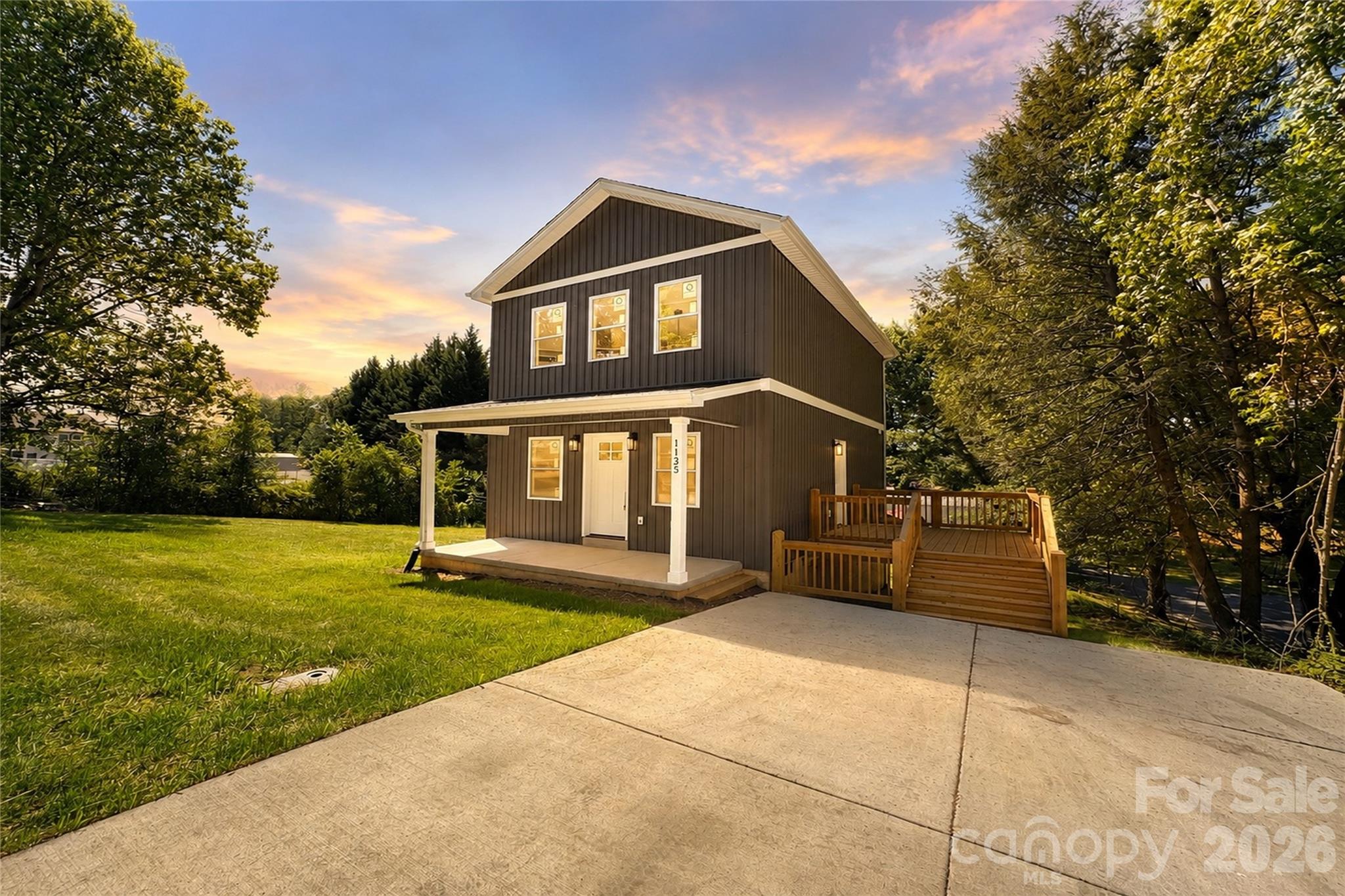 1135 Apple Lane offers a rare blend of modern design, architectural character, and functional flexibility — all tucked within a quiet and private setting just minutes from Granite Falls, Hickory, and Lenoir.

This newly constructed home immediately stands apart with its bold exterior presence, covered front porch, expansive side entertaining deck, and dramatic two-story interior design that creates a sense of openness far beyond what most homes in this category offer.

Step through the front door into an impressive open-concept living space highlighted by soaring approximately 20-foot ceilings, oversized windows, abundant natural light, and a striking vertical layout that gives the home a custom-built feel. The main living area flows seamlessly into the dining space and beautifully designed kitchen, creating an ideal environment for both everyday living and entertaining.

The kitchen was thoughtfully designed with upscale finishes including stainless steel appliances, shaker-style cabinetry, modern countertops, subway tile backsplash, matte black fixtures, and generous cabinet storage. The combination of clean lines, warm textures, and designer selections creates a polished modern aesthetic throughout the home.

One of the most visually impressive features of the property is the custom staircase with oak treads and contemporary railing system that overlooks the two-story great room below, adding both architectural interest and warmth to the interior.

The upper-level primary suite offers a private retreat complete with a walk-in closet and designer-inspired ensuite featuring a navy vanity accented by elegant gold hardware, modern lighting, and elevated finish selections rarely found at this price point.

On the main level, the home also features an additional flex/bonus room with closet that functions perfectly as a guest room, office, secondary sleeping area, workout space, or multipurpose room depending on your needs. A second full bathroom on the main level includes a striking black vanity with coordinating hardware and modern fixtures that continue the home’s cohesive upscale design.

Beyond the interior living space, the property also offers an unfinished walk-up basement area with exterior access, providing excellent storage potential for tools, outdoor equipment, seasonal items, or hobby space.

Outdoor living is equally inviting with both the covered front porch and oversized side deck creating multiple opportunities to enjoy morning coffee, evening gatherings, outdoor dining, or peaceful time surrounded by the property’s quiet natural setting.

Whether you are searching for your first home, a stylish low-maintenance primary residence, a flexible live/work setup, or an investment opportunity with strong modern appeal, 1135 Apple Lane delivers a unique combination of design, functionality, and value that is difficult to find in today’s market.