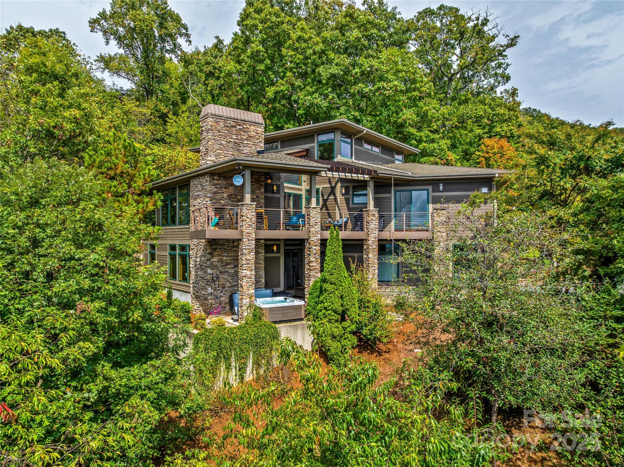 Exceptional home on Reynolds Mountain with long-range southwest views from nearly every room. Offering “top of the mountain views without being on top of a mountain,” this 4BR/3BA/2HB residence features 4,664 SF of thoughtfully designed living space with floor-to-ceiling windows that capture the mountains. The main level showcases an open living, dining, and kitchen area with custom cabinetry, multiple pantries, and seamless flow to outdoor spaces. A covered deck off the dining room connects to a fenced area, while the expansive back deck with durable Ipe decking includes a wood-burning fireplace and space for dining and entertaining. A separate patio with hot tub provides another private retreat to enjoy the views. The main-level primary suite offers sweeping views, a spa-like bath, generous walk-in closets, and a conveniently located laundry room. A second primary suite is located on the lower level, offering privacy and comfort for guests. The second level includes additional bedrooms and a bonus living space, each with its own mountain outlook. An oversized two-car garage provides ample room for vehicles, outdoor gear, and storage, all with direct access to the home. Just blocks from the , dining, and shops at Reynolds Village, this North Asheville location combines convenience with the privacy and views that define the Asheville lifestyle.