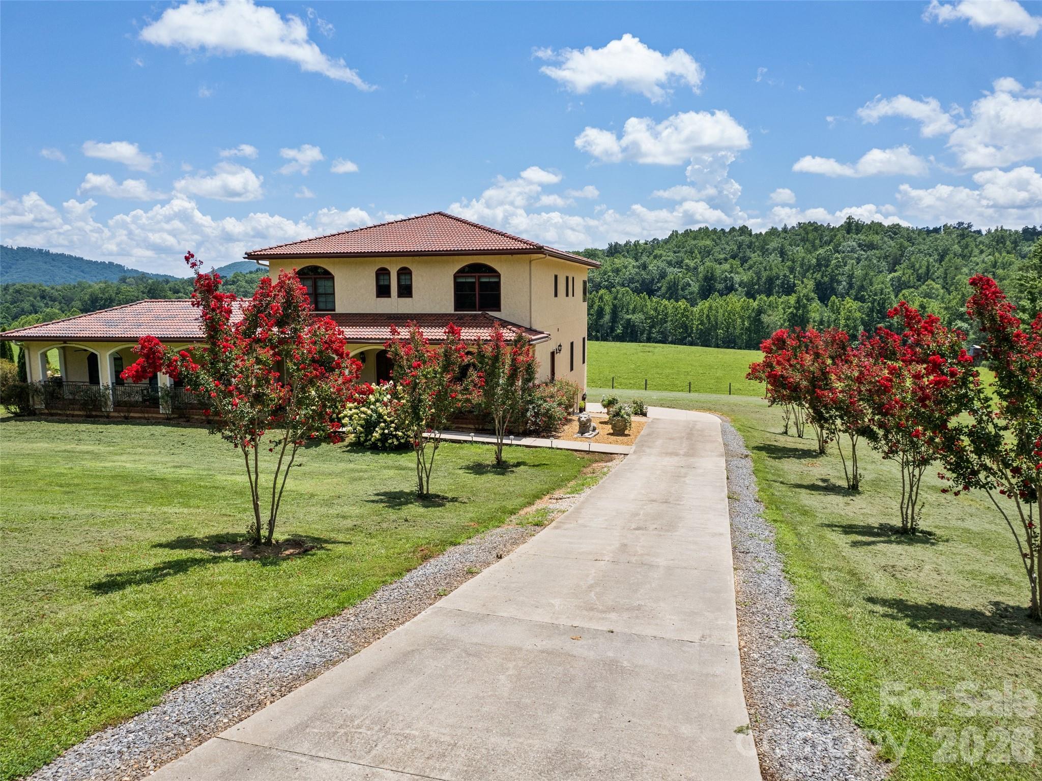Experience the romance of the Italian countryside without leaving Western North Carolina. Inspired by the timeless charm of Tuscany, this extraordinary 105-acre working farm blends refined Mediterranean architecture with productive agricultural infrastructure, creating a property that is as beautiful as it is functional. Approached through rolling pastures framed by mountain views, the estate unfolds across gently rolling acreage thoughtfully designed for livestock operations and luxurious country living. Rotational grazing pastures are equipped with automatic water feeders, while a cattle chute, multiple fenced grazing areas, two wells, well house and extensive farm infrastructure support the property's continued agricultural use. Two fully stocked ponds provide exceptional recreation and natural beauty, featuring bass, bluegill, catfish and minnows. A thriving two-acre vineyard further enhances the estate's Tuscan character and offers opportunity to continue a boutique vineyard operation or simply enjoy the beauty it brings to the landscape. At the heart of the property sits a beautifully renovated Mediterranean-style residence encompassing approximately 4,143 square feet. Extensively updated and thoughtfully expanded, the home seamlessly combines classic craftsmanship with modern conveniences. Rich hickory hardwood flooring flows throughout the main living spaces, while solid wood doors and custom finishes add warmth and authenticity. The chef's kitchen was completely reimagined with custom cherry cabinetry, quartz countertops, double ovens, microwave, dishwasher, gas range with pot filler, oversized pantry and an inviting coffee bar complete with wine cooler. Designed for everyday living and entertainment, the adjoining great room addition creates an expansive gathering space filled with natural light and views of the surrounding countryside. Convenience and accessibility are paramount, with an elevator serving all three levels of the home. Additional interior features include two gas fireplaces, a spacious mudroom with full bath, a Jack-and-Jill bath, zoned heating and air conditioning, Italian ceiling fans, new carpeting, and laundry facilities on the main and upper levels. The private primary suite serves as a retreat, featuring a balcony overlooking the farm, expansive walk-in closets, and sweeping views of the pastures, vineyard, ponds and mountains beyond. With three bedrooms and three-and-a-half baths, the home offers comfortable accommodations for family and guests while maintaining an intimate connection to the surrounding landscape. Outdoor living is equally impressive. A newly constructed heated saltwater pool provides a resort-style setting for relaxation and entertaining, while extensive landscaping creates a vibrant tapestry of seasonal color. Sixty-six rose bushes, walnut trees, apple trees and peach trees enhance the grounds, providing beauty and harvest opportunities throughout the year. Additional improvements include a three-bay garage, a newly constructed outbuilding with concrete flooring, storage building, doghouse, whole-house 20-kilowatt generator, and numerous farm-support structures that make daily operations efficient and convenient. A portion of the property is thoughtfully protected by a conservation easement, preserving the pastoral beauty and natural integrity of the landscape while enhancing the sense of privacy and permanence that makes this farm exceptional. The protected acreage complements the working farm operation and helps ensure the enduring character of the surrounding countryside. Whether envisioned as a working cattle farm, vineyard estate, equestrian property, family compound or private mountain retreat, this exceptional offering combines productive acreage, remarkable improvements and timeless Tuscan-inspired elegance into a rare Western North Carolina legacy property.
