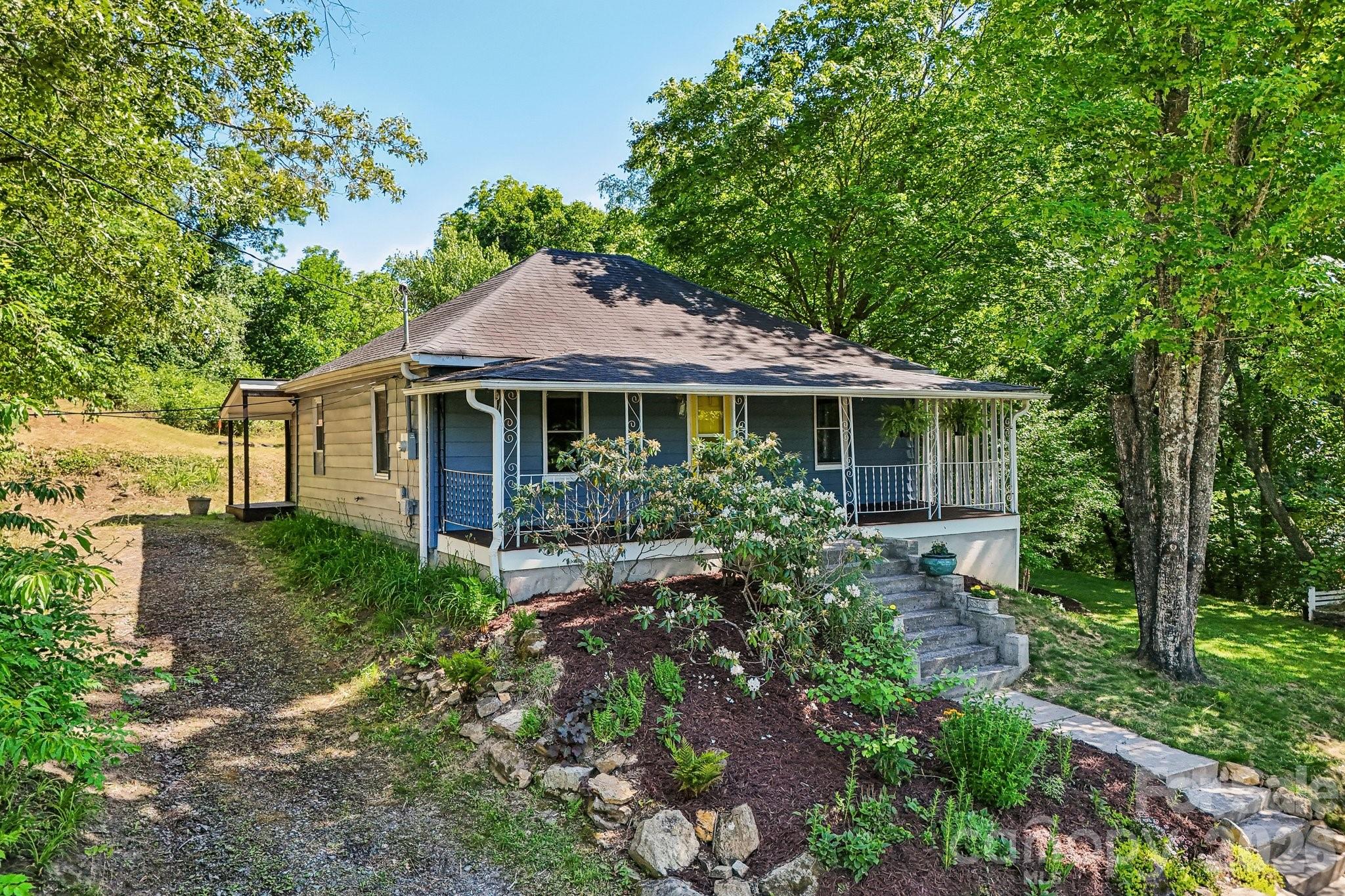 Tucked away on a quiet street in Oakley, just minutes from Biltmore Village and downtown Asheville, this thoughtfully reimagined 100-year-old bungalow blends historic charm with a distinctly modern, design-forward aesthetic. The home features a dramatic open layout with a soaring 12’ vaulted ceiling, creating an expansive feel rarely found in homes this size. The interior is inspired by mid-century modern and Art Deco influences, with warm antique brass accents and high-end light fixtures throughout. Original Red Oak hardwood floors, stained a rich walnut tone, run through much of the home and add warmth and character. The kitchen is a true centerpiece featuring semi-custom cabinetry, granite countertops, a striking waterfall island, and a custom corner pantry featuring a unique lazy susan with full extension wood drawers. Elevated lighting and refined finishes give the space an elevated, designer-quality feel that stands out from typical renovations. The home offers two versatile bedrooms and large closets, including a large primary bedroom and a comfortable second bedroom that easily accommodates a bed and desk, ideal for a guest room, child’s room, or stylish home office. The bathroom features a custom solid-wood vanity, marble top and art deco lighting with a high-end brass faucet. The flexible rear addition is filled with natural light from two large windows and finished with new LVP flooring. This bright, sunlit space is perfect as an office, mudroom, or creative studio. Outside, the 0.41 ac property features a flat and shady lawn with exceptional privacy, a fire pit area, and mature landscaping featuring Blackberries, Raspberries, Serviceberry, and Passion fruit plants.  A flowering shade garden, and a sunny pollinator garden complete the urban oasis feel.  The back of the property contains an additional lot with mountain views, perfect for building an additional home, an ADU/guesthouse, or more gardening and outdoor living space. Additional highlights include a welcoming front porch, a garden shed, and ample crawl space storage. On top of all that, proximity to Asheville’s newest outdoor music venue, Hellbender, the long-awaited new All Day Darling location, Burial Forestry Camp, and all that Biltmore Village offers, makes this property a must see!