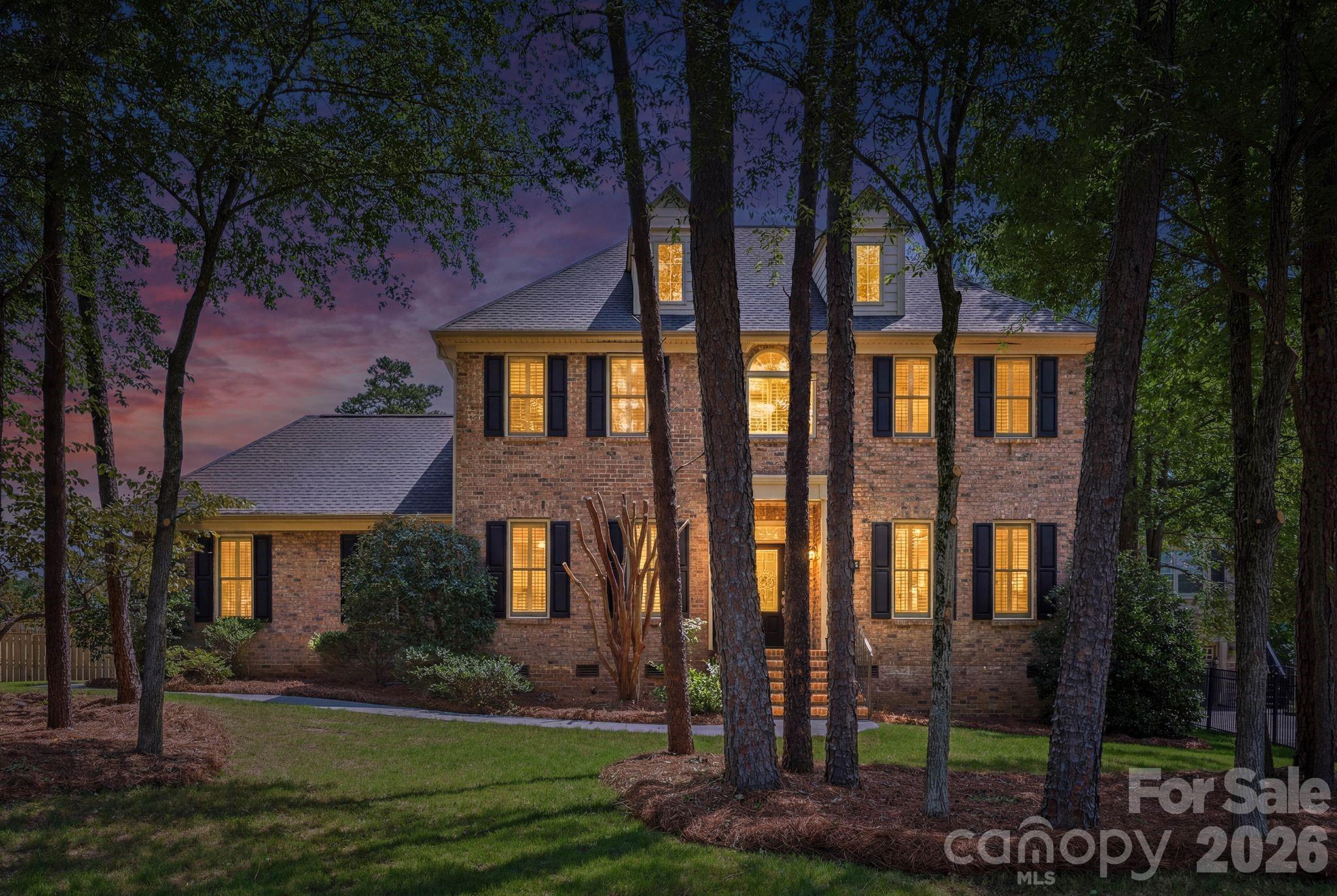 Timeless brick Traditional on a tree-lined corner lot
Set among mature pines and framed by manicured, pine-straw landscaping, this classic two-story brick home makes a striking first impression, twin dormers, black shutters, and a transom-and-sidelight entry give it timeless curb appeal. Step inside to a gracious open entry with a leaded-glass front door and stained-glass transom, gleaming herringbone-laid hardwoods, and elegant decorative columns that frame the space. Crown molding, tray ceilings, plantation shutters throughout, and wrought-iron stair railings carry that refined character across all 2,826 square feet.
The formal living and dining rooms open gracefully on either side of the entry, an ideal layout for entertaining, finished with tray ceilings, wainscoting, picture-frame molding, and a built-in butler's pantry with glass-front cabinetry. From there, the home flows to a kitchen with granite countertops, a center island, stainless steel appliances, raised-panel cabinetry, and a pantry, opening to a sunny breakfast area and a light-filled family room anchored by a floor-to-ceiling stone fireplace. Sliding glass doors lead from the family room out to the covered porch, blending indoor and outdoor living. A convenient half bath completes the main level.
Upstairs, the spacious primary suite is a genuine retreat, with a tray ceiling and an en-suite bath featuring a dual granite vanity, a soaking tub, and a separate shower. Just off the primary, a dedicated office with a charming arched window and built-in window seat makes the perfect work-from-home or study space. Three additional guest bedrooms round out the second floor.
But the outdoors is where this home truly shines. Set on an expansive .36-acre corner lot wrapped in gorgeous mature pines, the property enjoys a rare sense of privacy and seclusion for a corner setting. A striking timber-frame covered porch, with a vaulted cedar ceiling, exposed beams, and a stacked-stone base, steps down to a large circular paver patio made for firepit evenings, all within a fully fenced backyard. A side-load two-car garage and a storage shed add everyday practicality.
At 2,826 square feet on a tree-lined corner lot, with timeless finishes and one of the best outdoor spaces around, this one is special.