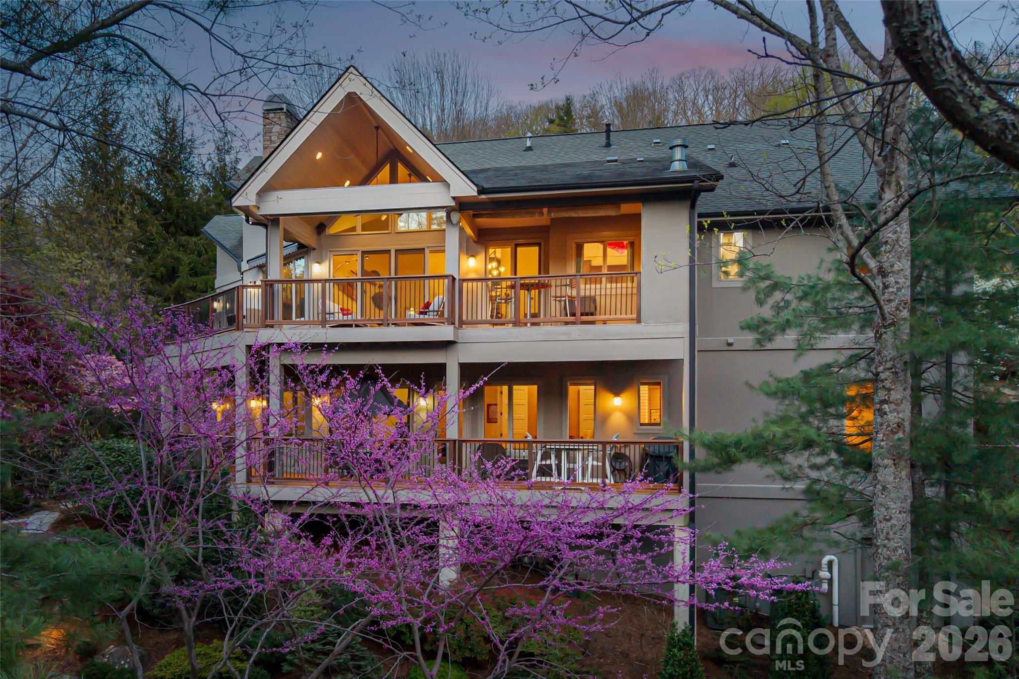 Set within the sought-after enclave of Reynolds Mountain and backing to a protected 16-acre nature preserve, this exceptional residence offers a rare sense of privacy and tranquility just minutes from vibrant downtown Asheville. Here, nature becomes part of everyday living, where rustling leaves, filtered sunlight, and layered mountain vistas create an atmosphere of calm and quiet sophistication. The grounds feel like a private botanical retreat, thoughtfully designed to blend seamlessly with the surrounding landscape. Tiered stone terraces, winding garden paths and curated native plantings unfold across the property, offering beauty in every season. Intimate garden rooms invite moments of reflection, while shaded seating areas and sunlit clearings create inviting spaces for gathering or peaceful solitude. Expansive covered and open-air decks extend the living experience outdoors, framing mountain sunsets, crisp morning air and evenings beneath the trees. A covered outdoor kitchen with a Viking grill elevates alfresco entertaining with understated elegance and ease. Inside, soaring windows draw natural surroundings into the home, filling the interiors with abundant light and a strong connection to the landscape beyond. The vaulted great room, anchored by a striking stone fireplace, creates a warm and welcoming focal point for everyday living and entertaining alike. Thoughtfully designed for comfort and flexibility, the floor plan offers generous living spaces, refined finishes and effortless flow throughout. The primary suite serves as a peaceful retreat, while the lower level is ideally suited for relaxed living, guests, recreation or entertaining. Energy Star efficiency and lock-and-leave convenience further enhance the home’s appeal, making it ideal either as a full-time residence or mountain getaway. This offering also represents one of the most compelling opportunities available in Reynolds Mountain, delivering the squarest footage at the lowest price point in single-family residences within the community and an exceptional value for the setting, quality and lifestyle offered. With the seller relocated and highly motivated, the opportunity is even more attractive for buyers seeking immediate availability and outstanding long-term value. Rarely does a property combine privacy, natural beauty, generous living spaces and proximity to Asheville so seamlessly. This is refined mountain living designed for quiet retreat and effortless connection to everything Western North Carolina has to offer.
