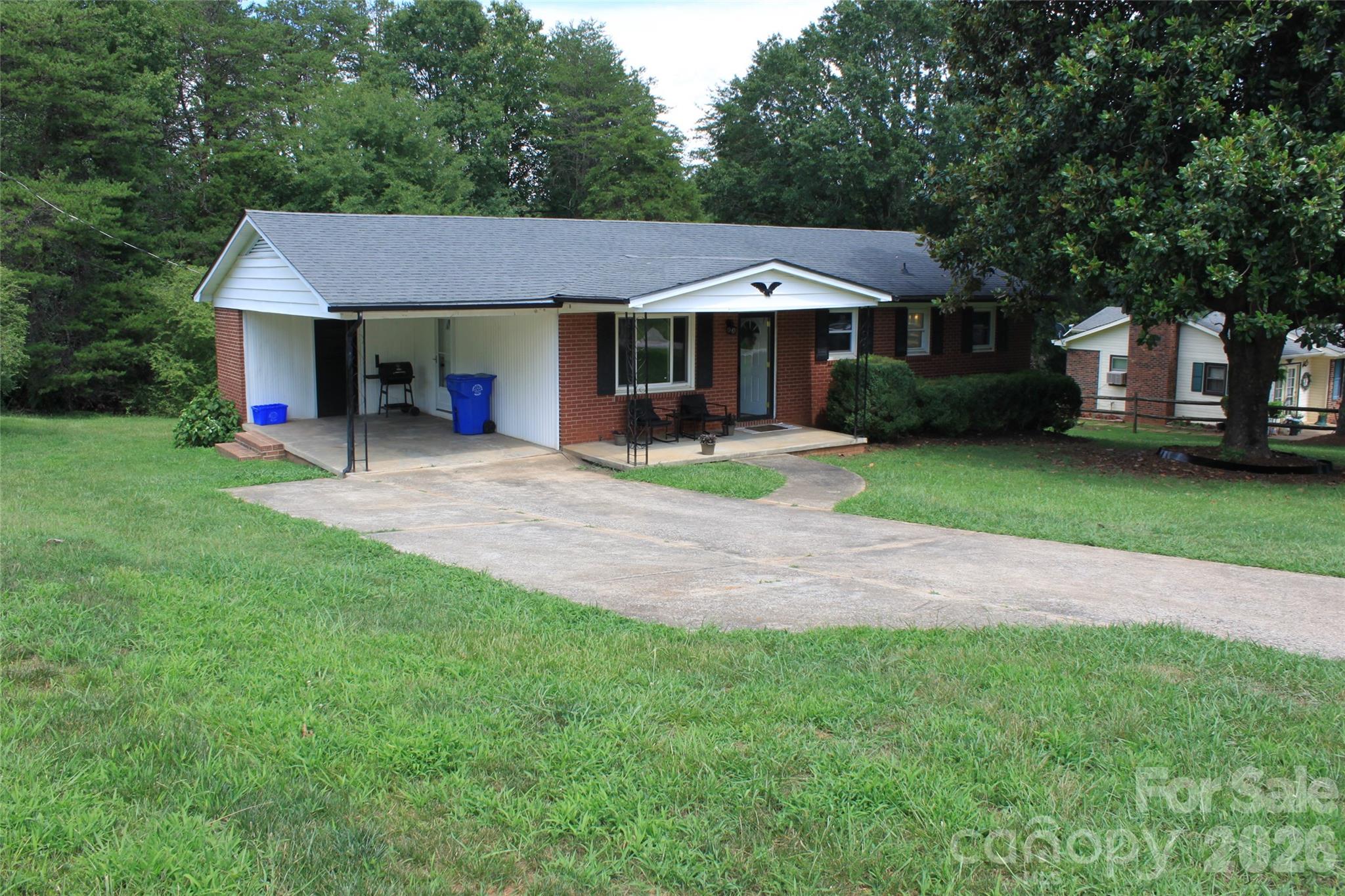 Set on a wooded corner lot along a quiet dead-end street, this 3-bedroom, 1.5-bath brick ranch offers a peaceful setting with convenient access to both Rutherfordton and Forest City. The covered front porch creates a welcoming first impression, while the paved driveway and attached carport provide easy everyday parking. Inside, hardwood floors add warmth to the living spaces, and the spacious eat-in kitchen offers room to gather, dine, and enjoy daily routines, complemented by durable luxury vinyl plank flooring. The primary bedroom includes a private half bath and walk-in closet, while two additional bedrooms provide flexibility for guests, an office, or hobbies. Insulated windows and a smart thermostat enhance comfort and efficiency, and the architectural shingle roof was replaced in 2015. Outside, the large backyard and mature trees create a private natural backdrop with space to relax, garden, or entertain. An exterior laundry room, not included in the heated square footage, adds useful storage and functionality, while the large, easily accessible crawl space offers additional convenience. City water, city sewer, trash pickup, and recycling service complete this well-located home near town.