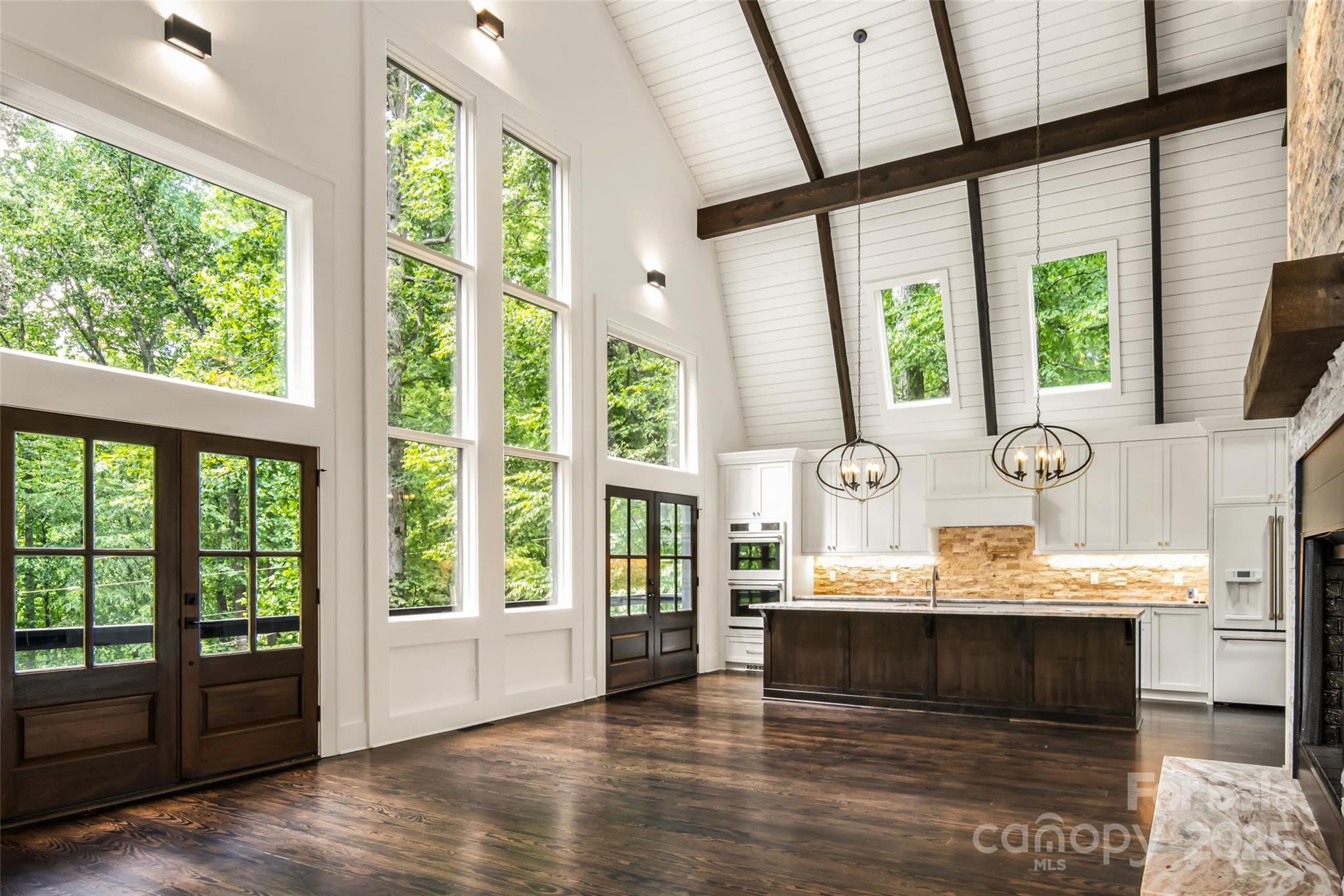 Now offered at an improved price of $899,900, this extraordinary mountain retreat presents the kind of opportunity that rarely comes along—whoever calls it home next is stepping into an exceptional value for the level of renovation, craftsmanship & luxury offered throughout. Tucked among the trees offering a rare blend of refined design just minutes from the heart of Burnsville. A dramatic open living space showcases a 300+ sqft expansion, soaring 30-ft ceilings & walls of windows that flood the home w/natural light & lush treehouse-like views from every vantage point. An open, flowing layout is anchored by the finest finishes throughout, creating an atmosphere that is both grand & inviting. At the heart of the home is a bespoke entertainer’s kitchen featuring extensive custom cabinetry & an oversized island that easily seats 6+. Premium matte white GE Café appliances include electric induction cooktop w/pot filler, French-door refrigerator, apron-front sink, double ovens, microwave drawer, dishwasher, disposal & striking custom pendant lighting—an ideal setting for both everyday living & elevated entertaining. Kitchen opens seamlessly into the sprawling GR, highlighted by a new wood-burning FP w/an impressive 18-ft stacked-stone surround, expansive firebox, rustic mantel w/artisan-crafted iron brackets & granite raised hearth. Fully appointed wet bar w/custom cabinetry (including glass-front uppers), granite countertops, premium hardware, undermount stainless sink & dual wine refrigerators. Adjacent to the GR, newly added den/dining/seating rm features vaulted ceiling & 2nd FP w/shiplap surround, rustic mantel, iron brackets & granite hearth—perfect for intimate gatherings or relaxed evenings by the fire. 2 primary ensuite BRs, one on main level (fully wheelchair accessible) & one on upper level, each featuring elegant electric FPs w/shiplap surrounds & rustic mantels. 2 additional spacious guest BRs located on LL. 3.5 spa-inspired BAs boast custom marble & ceramic tilework, w/heated floors in 2 BAs. Both primary suites include large closets w/custom organizer systems & luxurious BAs w/double vanities & glass-enclosed tiled showers; main-level primary also features a bubble-jet soaking tub. Adding to the home’s versatility are 2 loft spaces. 2nd-level loft, just outside the upper primary suite, includes a granite-topped dry bar w/beverage/wine refrigerator, lighted glass shelving & lounge area. 3rd-floor loft—accessed by a tuck-away ladder—offers exceptional flex space for sleeping, office, or creative retreat, complete w/operational skylights, new windows & wall sconces. Thoughtful up-lighting along ceiling beams gently washes ceilings, creating a warm & inviting evening ambiance throughout. LL features 2 Guest BRs, a beautifully designed shared BA w/heated floors, glass shower enclosure, dual ceiling-mounted rain shower heads, handheld wands, new transom window & double vanity. LL includes multiple storage closets, wine rm w/custom wall-wash lighting (easily convertible to a media rm, home gym, or workshop), utility closet w/water filtration & softening systems & an attached garage. Multiple access points lead to a covered patio w/FP, including direct access from one of the BRs. Outdoor living is equally impressive w/a brand-new firepit & grilling area, exterior driveway & peaceful, private setting ideal for entertaining or unwinding beneath the stars. Additional highlights include new interior & exterior paint, new roof, new gutters w/gutter guards, extensive electrical & plumbing updates, new hybrid hot water tank, newer HVAC, new well & pressure pumps & fully serviced septic system (4-BR permit on file). Ideally located just 5 minutes from downtown Burnsville & Toe River Arts & only 35 minutes from Asheville, this exceptional property offers luxury, privacy & convenience—with no HOA fees & no hurricane damage. A truly remarkable mountain retreat where craftsmanship, comfort & setting come together in perfect harmony.