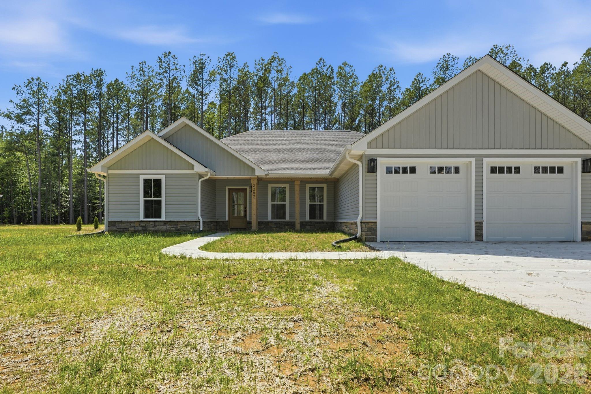 Recently completed and now available with NO HOA, discover North Pines—Lincolnton’s newest collection of thoughtfully crafted single-level homes by Brancer Homes. Located at 2287 Lee Lawing Road, this home blends elevated finishes with the natural privacy of tree-lined surroundings—all just 15 minutes from downtown Lincolnton and convenient to shopping in Sherrills Ford and Denver.

The exterior welcomes you with signature stone accents and stained wood front-porch columns, creating classic curb appeal with a warm farmhouse touch. Inside, the builder’s Modern Farmhouse Designer Package features clean lines, curated lighting selections, stylish cabinetry finishes, and quartz countertops throughout—bringing a fresh yet timeless aesthetic to every space.

The open-concept kitchen offers a spacious island with pendant lighting and flows seamlessly into the vaulted main living area, creating an airy and inviting environment ideal for both everyday living and entertaining. The primary suite is thoughtfully designed with a beautifully tiled shower wall and designer finishes that blend farmhouse character with modern convenience.

Additional highlights include a well-appointed laundry room with cabinetry and quartz counters, added recessed lighting, and designer neutral paint selections with crisp white ceilings. An extended two-car garage with exterior exit door, along with additional driveway parking, enhances everyday functionality.

Now that construction is complete, this home is part of a newly released collection in North Pines—offering a rare opportunity to own move-in ready new construction with elevated design, no HOA, and a peaceful rural setting in one of Lincolnton’s fastest-growing areas.