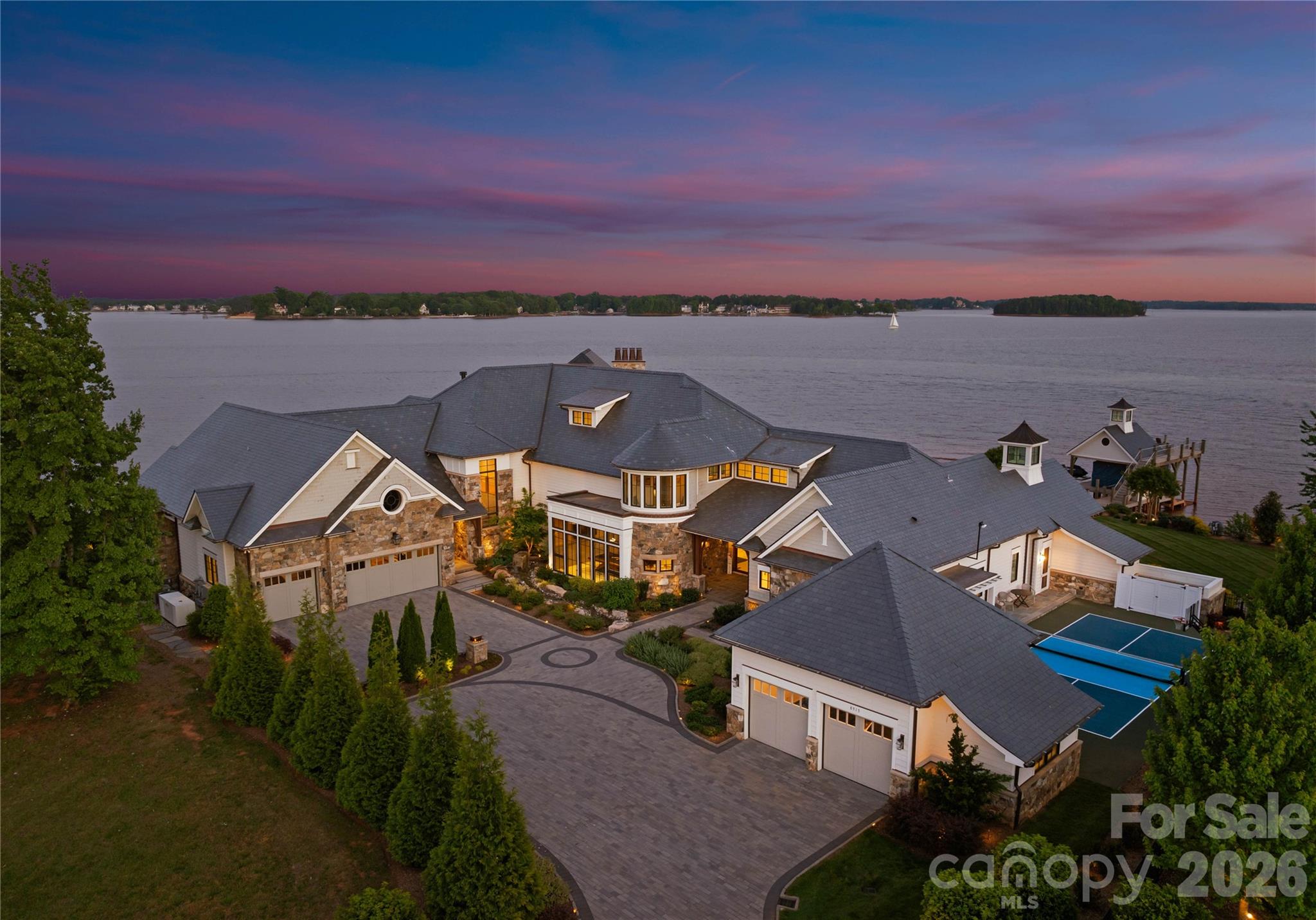An architectural masterpiece designed by renowned architect Harry Schrader and custom built by Kingswood Custom Homes, this extraordinary waterfront estate represents the pinnacle of luxury living on Lake Norman. Positioned on a breathtaking peninsula point lot within the exclusive gated community of Norman Estates, the residence captures sweeping panoramic open-water views while delivering a rare blend of timeless design, exceptional craftsmanship, and resort-inspired amenities. Spanning more than 11,000 square feet, the home was thoughtfully designed to maximize natural light and seamless indoor-outdoor living through dramatic floor-to-ceiling windows and expansive entertaining spaces overlooking the lake. Sophisticated architectural details, curated finishes, soaring ceilings, and rich textures create an atmosphere that is both grand and inviting. Every element of the home was intentionally crafted to balance elevated entertaining with comfortable everyday living. The main level features a luxurious lakeside primary suite, elegant dining spaces, private office, fitness studio, billiards lounge, custom wine cellar, and a chef’s kitchen appointed with premium appliances and expansive gathering areas designed for effortless entertaining. Additional guest suites, media spaces, and custom bunk accommodations provide exceptional flexibility for hosting family and guests in comfort and style. Outdoor living rivals a private luxury resort with expansive covered terraces, vaulted entertaining spaces, a screened porch, built-in fire features, outdoor kitchen, manicured grounds, and a stunning infinity-edge pool and spa overlooking the waters of Lake Norman. A private dock complete with a boat lift, dual jet ski lifts, and upper-level sun deck further enhances the extraordinary waterfront lifestyle while maximizing the property’s breathtaking long-range lake views. Thoughtfully designed to feel equally suited for two as it is for hosting over 100 guests, the estate balances refined luxury with effortless livability. Curated for elevated living, the home also includes a regulation pickleball court, private theater, full entertaining bar, five-car garage, whole-home generator, surround sound, and security system. Offered fully furnished and turnkey, this is a once-in-a-generation opportunity to own one of Lake Norman’s most iconic and architecturally significant waterfront estates.