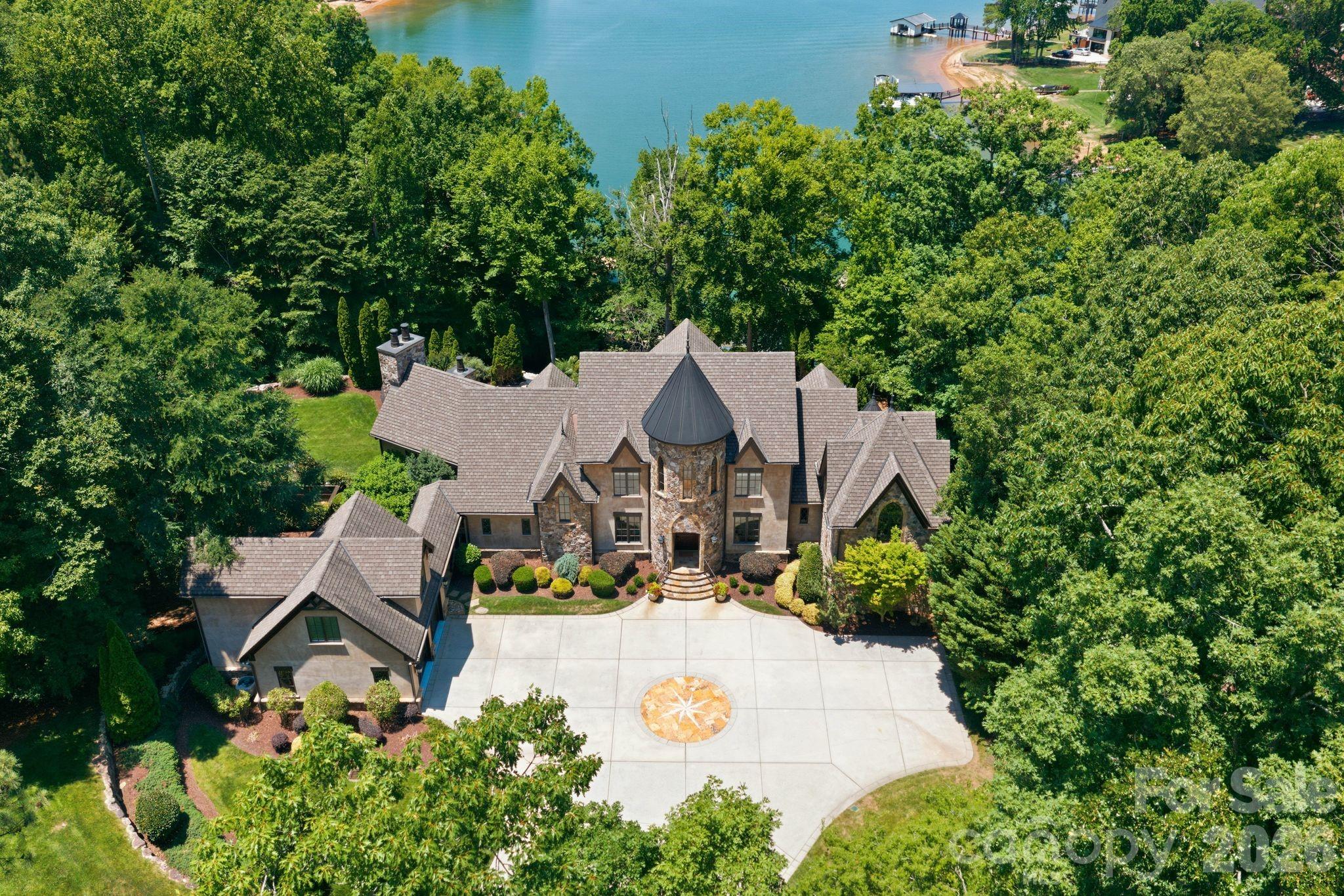Home to NASCAR champion Martin Truex Jr., this extraordinary European-inspired estate is a rare offering on the shores of Lake Norman, blending timeless elegance with the warmth and comfort of true lakefront living. Privately nestled behind gates on nearly five waterfront acres, the estate spans more than 14,000 square feet and offers an unparalleled sense of serenity, privacy, and craftsmanship.

A picturesque, tree-lined drive welcomes you to the impressive main residence, complemented by a charming carriage house with guest apartment and an expansive workshop and garage ideal for collectors and automotive enthusiasts alike. Inside, the home is both grand and inviting, featuring a breathtaking living room with soaring ceilings and panoramic lake views, a chef’s kitchen designed for gathering, elegant formal dining spaces, and a luxurious main-level primary suite complete with a spa-inspired bath and dramatic two-story dressing room.

Upstairs, beautifully appointed en-suite guest accommodations and a private office with loft provide comfort and flexibility for both family and guests. The fully finished lower level was designed for entertaining on every scale, offering a custom bar, private theater, fitness studio, and spacious recreation area.

Outdoors, the estate transforms into a resort-style retreat with an infinity-edge pool, cascading waterfall, fire pit, and private dock with boat lift — all perfectly positioned to capture the beauty of the water and unforgettable sunsets. A detached garage with finished space above adds even more versatility for guests, hobbies, or additional entertaining space.

Equal parts sophisticated and welcoming, this remarkable property offers the ultimate luxury lake lifestyle with a championship pedigree.