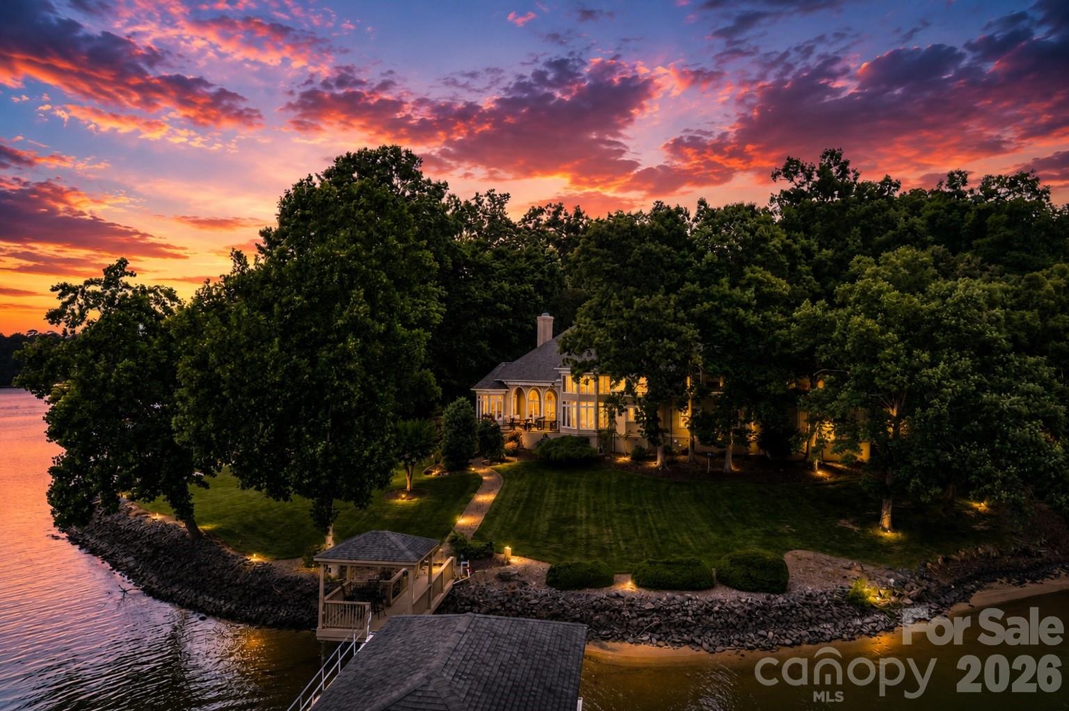 Experience the best of Lake Wylie living—where luxury, privacy, and an unmatched waterfront lifestyle come together just minutes from Charlotte. Whether you're relocating to the Charlotte area, searching for a private waterfront retreat, or looking for a home designed for effortless entertaining and multi-generational living, this extraordinary estate offers a rare opportunity to own one of the lake's most exceptional properties.
Nestled on a private road shared by only five homes, this remarkable waterfront estate boasts over 450 feet of flat shoreline, breathtaking main-channel views, deep water, and exceptional privacy. Located just minutes from Charlotte, Charlotte Douglas International Airport, premier dining, shopping, and everyday conveniences, it offers the perfect balance of peaceful lakefront living and city accessibility. Designed for today's lifestyle, the home features two luxurious main-level primary suites, making it ideal for multi-generational living, long-term guests, or those seeking the ease of main-level living without compromise.
Waterfront & Grounds
One of the property's most remarkable features is its over 450 feet of flat, usable shoreline, offering deep-water access, a private sandy beach, and breathtaking long-range lake views—a combination rarely found on Lake Wylie. Enjoy boating, fishing, paddleboarding, kayaking, and swimming directly from your backyard while taking in unforgettable sunsets.
A private dock complete with a boat lift, floating dock, pier, and additional electrical service provides effortless access to the lake.
The beautifully landscaped grounds feature mature specimen plantings including Blue Atlas Cedars, Mugo Pines, Colorado Blue Spruce, Japanese Maples, and numerous ornamental trees and shrubs connected by winding stone walkways that enhance the waterfront setting.
Main Residence
Designed to maximize the stunning lake views, the home showcases dramatic floor-to-ceiling windows, soaring ceilings, extensive custom millwork, and abundant natural light throughout.
A standout feature of the home is its two luxurious main-level primary suites—an incredibly rare offering that provides exceptional flexibility for multi-generational living, visiting family, aging parents, or long-term guests. The lakeside owner's suite offers panoramic water views, a spa-inspired bathroom, and dual custom walk-in closets with extensive built-ins, while the second main-level primary suite provides its own private retreat with beautifully appointed finishes and easy accessibility.
Formal dining spaces feature a stunning double tray ceiling with uplighting and designer fixtures.
At the heart of the home is a chef's kitchen featuring custom Canadian maple cabinetry, premium appliances, an oversized island, wet bar, walk-in pantry, and a fully equipped scullery designed for effortless entertaining.
Upstairs, spacious guest suites offer beautifully appointed bathrooms, generous storage, abundant natural light, and a dedicated home theater with stadium seating.
Perfect for buyers relocating to Charlotte, this home combines the serenity of lakefront living with unmatched convenience. Enjoy lower South Carolina property taxes, award-winning Fort Mill schools, and an easy commute to Uptown Charlotte, Charlotte Douglas International Airport, premier golf clubs, and the region's top dining and shopping destinations—all while living on one of Lake Wylie's most coveted waterfront properties.