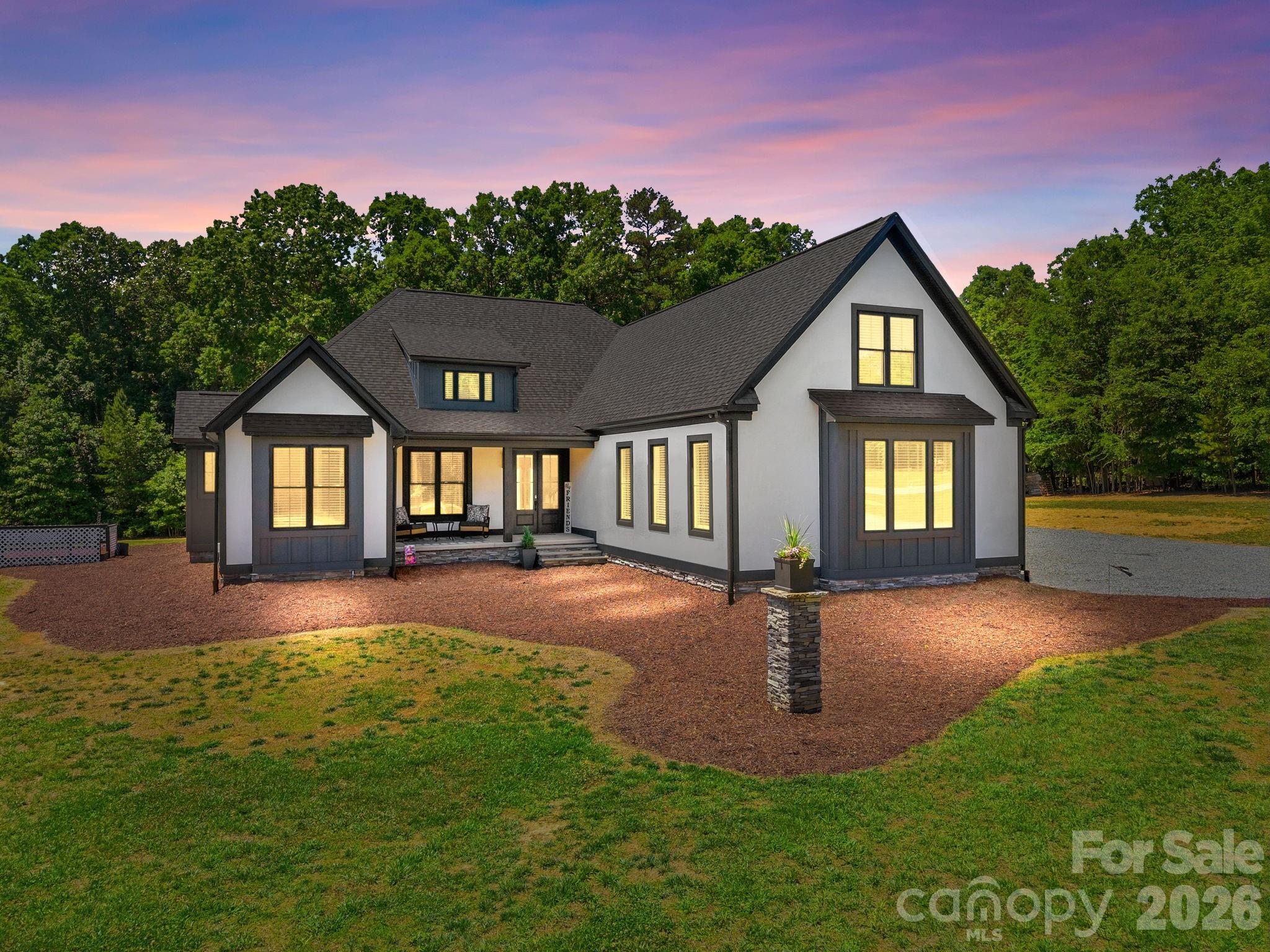 Completed in 2023 and set on nearly 5 acres along one of Rowan County's most sought-after corridors, this 3,502 sq ft masterpiece blends bold architectural style with thoughtful, high-end finishes at every turn. From the striking white stucco exterior with dark board-and-batten accents and dramatic roofline to the covered rear porch with timber-frame gable, vaulted tongue-and-groove ceiling, and stacked stone base — this home was built to impress inside and out. Step through the front door into an open-concept main level where the great room, kitchen, and dining area flow seamlessly together. The chef's kitchen is a showstopper, featuring floor-to-ceiling white shaker cabinetry, quartz countertops, a large center island with farmhouse-style detail, dual wall ovens, a pot filler, custom tile backsplash, and stainless steel appliances all anchored by dramatic matte black pendant lighting. Just off the kitchen, a dedicated coffee and beverage bar with floating wood shelves, under-counter wine/beverage cooler, and built-in sconce lighting adds a boutique hotel feel to everyday living. The great room centers around a sleek linear fireplace set into a custom dark shiplap surround with built-in shelving, and expansive sliding glass doors open directly onto the covered outdoor living area making indoor-outdoor entertaining effortless. The main-level primary suite is a true retreat, featuring a designer accent wall with board and batten detail, private exterior access, and a spa-caliber en suite bath with dual vanities, quartz countertops, a freestanding soaker tub framed by a picture window, a floor-to-ceiling marble tile walk-in shower with frameless glass, and designer pendant lighting. Three additional bedrooms and 2.5 more baths round out the 4-bedroom, 3.5-bath layout across two levels, including a flex space and bonus room upstairs. The 3-car attached garage is oversized and polished with finished floors, a barn-style interior access door, and abundant natural light  the perfect space for vehicles, hobbies, or a workshop. Outside, the rear covered porch with outdoor dining and lounge areas overlooks the private, wooded lot — a peaceful setting that feels miles away from everything, yet sits right on the Bringle Ferry Road corridor connecting Salisbury to High Rock Lake. Well and septic, conditioned crawl space, no HOA, and no city taxes round out the appeal.