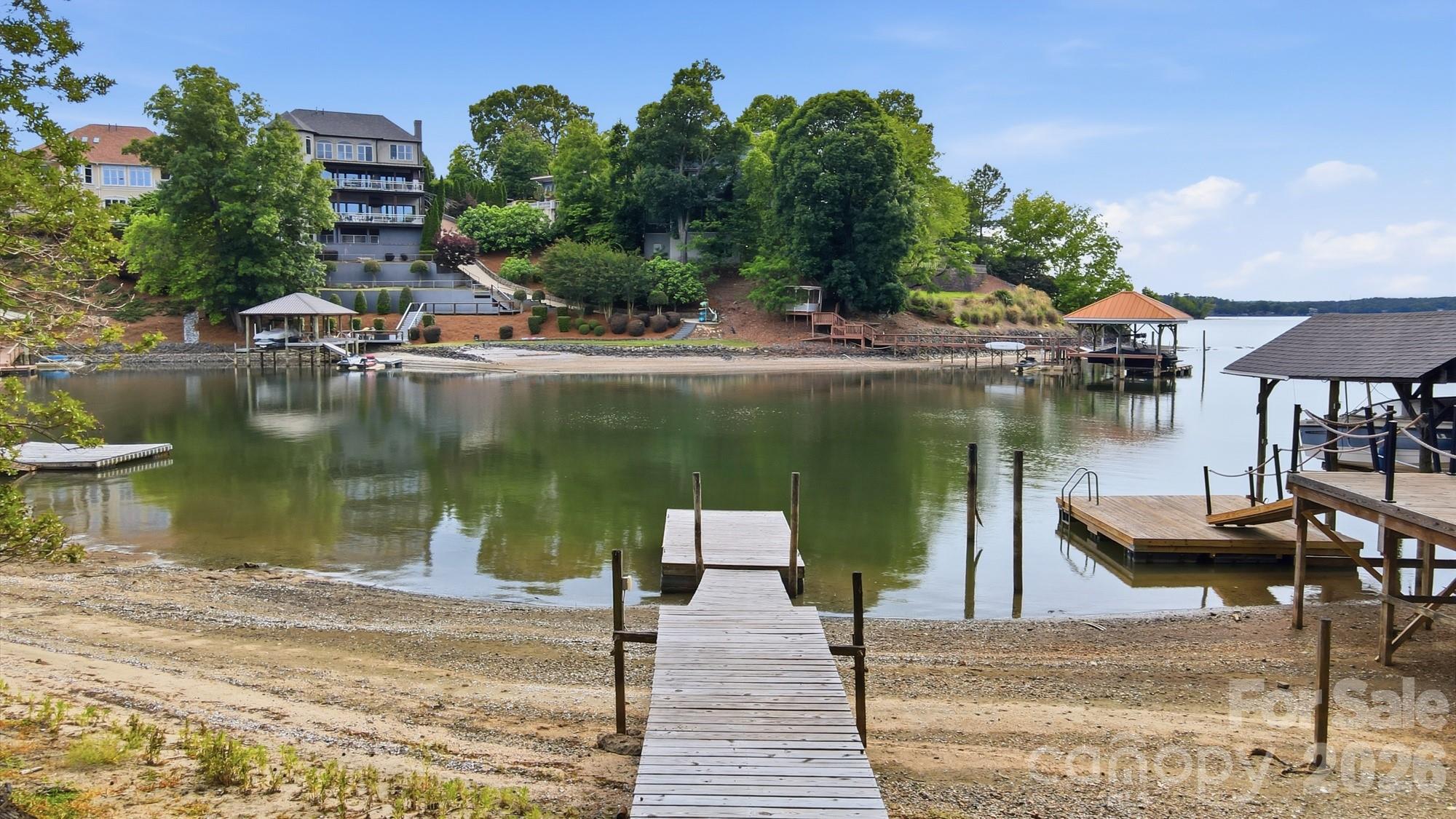 Where every day feels like a vacation—welcome to this stunning Lake Wylie retreat! Tucked just off the main channel, this beautiful waterfront home offers the perfect balance of peaceful cove living and sweeping big-water views. Designed to fully embrace the outdoors, the property features over 100 feet of waterfront and multiple expansive decks spanning the back of the home across three levels. With sleek wire railing and unobstructed sightlines, each space is perfectly positioned to take in breathtaking sunsets and panoramic lake views. A balcony off the second-level office adds yet another vantage point to enjoy the scenery. Follow the wooden walkway down to your own sandy beach and fire pit area—ideal for relaxing evenings by the water. A newly replaced PRIVATE floating dock provides immediate access to lake life, whether it’s morning coffee by the water, afternoon boating, or sunset cruises. Inside, the home has been completely remodeled, blending modern upgrades with timeless character. The two-story great room is a showstopper, featuring a stunning stone wood-burning fireplace, soaring beamed cathedral ceilings, and a wall of windows showcasing the lake. The open-concept layout flows seamlessly into a chef’s kitchen outfitted with high-end quartz countertops, stainless steel appliances, custom cabinetry, a deep apron-front sink, and an oversized breakfast bar perfect for gathering. The main-level primary suite is a private retreat with deck access, a spacious walk-in closet, and a beautifully updated en-suite bath with a large tiled shower. The upper level offers a loft/office space with balcony access and incredible views. Downstairs, you’ll find three additional bedrooms (one ideal as a bonus room), along with a laundry area and two full bathrooms—providing plenty of space for guests and entertaining. Set beneath a canopy of mature trees on over a quarter-acre lot, this property offers rare privacy with no HOA along with the convenience of a spacious two-car garage. Extensive upgrades include a newer roof, newer HVAC, tankless hot water heater, new doors, flooring, and high-end finishes throughout. Enjoy the best of Lake Wylie living with easy access to dining, shopping, and top-rated schools—all just 20–25 minutes from Uptown Charlotte. This is more than a home—it’s a lifestyle!