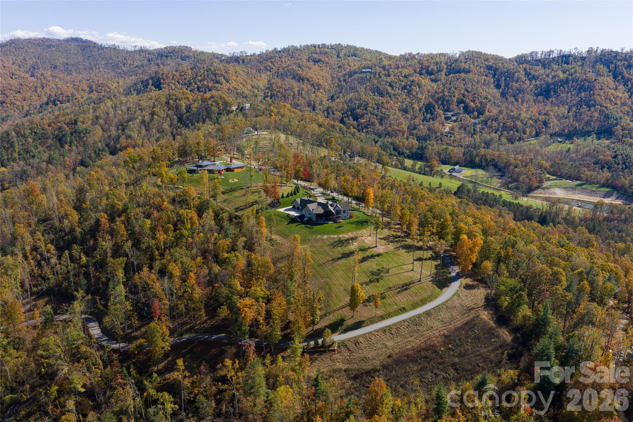 Across 38.45 acres overlooking Weaverville's desired Reems Creek Valley, this exceptional estate offering combines a luxury mountain residence with an adjoining 19.43-acre parcel, creating a rare opportunity for those seeking privacy, flexibility and the ability to expand beyond a traditional mountain home. The combined acreage introduces a unique blend of long-range mountain views, usable land, mature hardwood forests, a private pond, and extensive estate potential just minutes from downtown Weaverville and Asheville. A circular driveway winds through natural landscaping, where stone elements are artfully integrated to create a striking and private arrival. Inside, the residence showcases a level of fit and finish that defines luxury mountain living. A dramatic entry with herringbone-patterned hardwood floors introduces the home, flanked by a richly appointed office with custom built-ins and a formal dining room with tailored millwork. The great room unfolds with vaulted ceilings, exposed wood beams, and antler chandeliers, anchored by a statement fireplace with integrated cabinetry. Framed by soaring timber beams, the covered rear porch is a seamless extension of the home's design, offering scale and comfort. Automated screens create an indoor-outdoor experience while preserving the sweeping mountain views, and a stone fireplace anchors the space for year-round enjoyment. Just beyond, an open-air grilling deck adds function and flow, ideal for effortless entertaining in an elevated setting. The kitchen is a showpiece and a functional culinary space, anchored by an oversized island with quartz surfaces and custom beam detailing. A curated suite of Hestan appliances includes a commercial-grade range with griddle and dual ovens, wall oven, warming drawer, microwave and dishwasher, complemented by a built-in Miele espresso system. The walk-in scullery elevates functionality with extensive built-ins, a prep sink, quartz counters and a dedicated wine tower, while the adjacent breakfast nook captures morning light and views of the landscape. Privately positioned, the primary suite offers a retreat with vaulted ceilings, wood beam accents, a fireplace and direct access to a private deck overlooking the mountains. The spa-inspired bath features herringbone tile flooring, a freestanding soaking tub, dual vanities with under-cabinet lighting and quartz countertops, and an oversized walk-in shower with dual heads and integrated seating. Barnwood accents, curated lighting and a custom walk-in closet complete the experience. Two additional guest suites on the main level provide comfort and privacy, while the lower level continues the home's sense of scale with a spacious family room, full bar and secondary kitchen, additional guest accommodations, and seamless access to outdoor living spaces. The addition of the adjoining 19.43-acre parcel elevates the property into an estate offering. Featuring gently rolling wooded terrain, a picturesque pond with dock, and a substantial outbuilding used for tractor and equipment storage, the expanded acreage provides exceptional flexibility for a guest house, caretaker's residence, family compound, equestrian pursuits, recreational amenities, private trails or future estate expansion. The combination of open view corridors, usable terrain, and natural privacy creates opportunities rarely available in such proximity to Asheville. Designed for everyday living and elevated entertaining, the estate includes an attached one-car garage connected by a breezeway to a two-car garage outfitted as a private gym, along with the peace of mind provided by a whole-home generator. Combining luxury craftsmanship, panoramic mountain views, a private pond, versatile outbuilding and 38.45 acres of usable mountain land, this offering presents a compelling opportunity to create a legacy property in one of Western North Carolina's desirable settings.