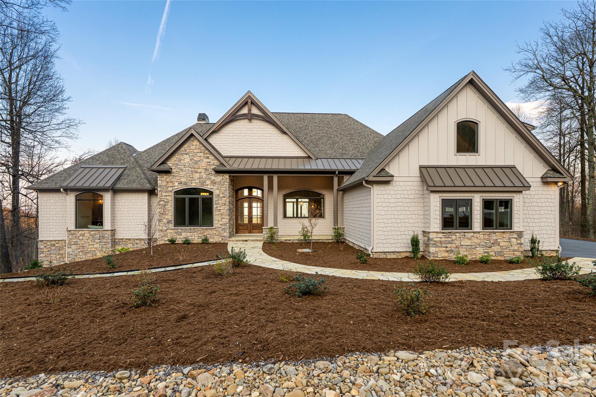 Set in the mountain enclave of Cobblestone Village, this new custom residence offers a rare balance of privacy and convenience — just five minutes to Kenmure Country Club, six minutes to Flat Rock, and ten minutes to downtown Hendersonville, with easy access to Asheville and Greenville. On over three acres, the home commands expansive, long-range, layered mountain views across the Blue Ridge, making it a compelling option for buyers relocating to western North Carolina for retirement or seeking a low-maintenance second home in the Hendersonville–Flat Rock–Zirconia corridor.

A flagstone walkway, Hardie-shake siding, and stone accents introduce a home defined by craftsmanship and scale. Inside, oak hardwood floors run through a light-filled, open-concept main level anchored by a vaulted great room with exposed beams, a gas fireplace, and custom built-ins, all oriented toward the mountain backdrop. The kitchen pairs granite countertops and a large island with a curated appliance suite, including a Fulgor Milano 36-inch range and wall oven, a walk-in pantry, and a built-in banquette. Living spaces extend to a covered deck with vaulted ceilings and a stone fireplace, built for year-round outdoor living.

The primary suite functions as a private retreat, with a coffered ceiling, sitting area, dual walk-in closets, and direct deck access. The en-suite bath includes heated tile floors, dual vanities, a soaking tub, and a walk-in shower. An executive office, well-appointed laundry room, and drop zone off the three-car garage round out the main level's everyday livability. An elevator connects to a lower-level recreation room with a gas fireplace, wet bar, and covered patio access, along with additional bedrooms, flexible living space, and a steam shower for guests. Above the garage, a private en-suite studio offers further flexibility as a guest suite, office, or creative space.

Systems throughout reflect the same attention to detail: a zoned Trane gas furnace with humidifier, tankless water heater, central vacuum, and a whole-home Generac generator. Outside, the acreage allows room to expand outdoor living, including a fire pit area, while the surrounding privacy and mature landscape preserve the mountain setting.

Just minutes from Kenmure Country Club — with Full Golf, Sports, and Social Membership categories available separately — 527 Falkirk Way places residents close to a signature golf course, clubhouse dining, tennis, pickleball, and year-round social programming, in addition to the shops, dining, and healthcare of Hendersonville and Flat Rock. This turnkey mountain residence pairs new-construction quality with timeless design, exceptional long-range views, and genuine proximity to everything western North Carolina mountain living offers.