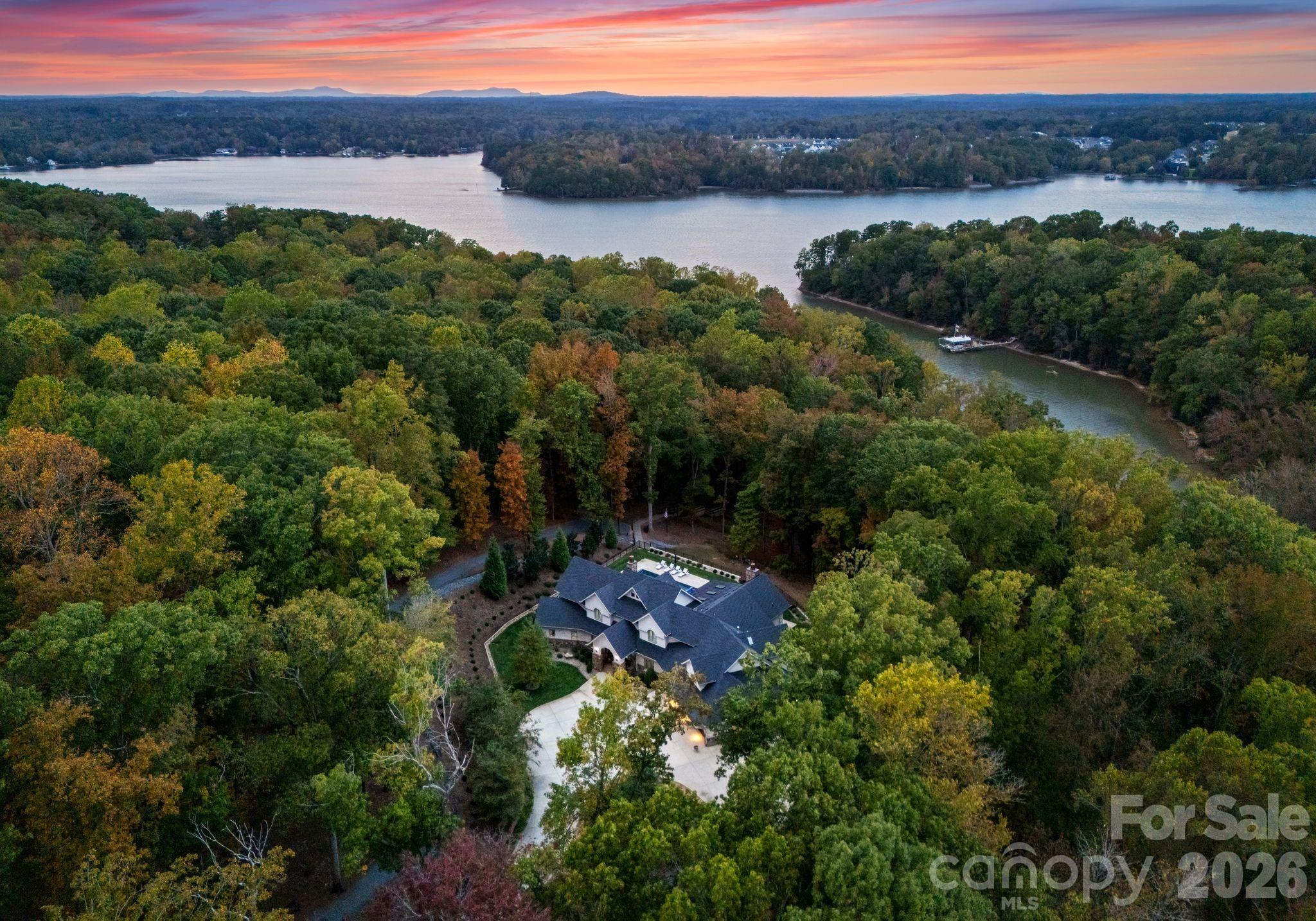 Tucked deep within the prestigious Sanctuary community at Lake Wylie, this extraordinary waterfront estate offers the rare combination of 9.6 acres, ultimate privacy, and resort-level living. A long, tree-lined drive sets the tone as you approach the stately stone and wood exterior, complete with an expansive motor court and multiple garage bays. Inside, timeless architecture meets modern refinement with wide-plank hardwoods, detailed millwork, coffered and tray ceilings, and expansive windows framing serene wooded views. The primary suite is privately positioned on the main level and feels like a retreat of its own—featuring a spa-inspired bath with marble finishes, soaking tub, oversized glass shower, dual vanities, and exceptional his and hers custom dressing room. The heart of the home is designed for gathering, with an open-concept chef’s kitchen boasting a large center island, professional appliances, custom cabinetry, and seamless flow into the great room with exposed beams and a statement fireplace. A formal dining space and dedicated office add elegance and function. Upstairs offers generously sized secondary bedrooms and additional flexible living areas, while the layout provides ideal separation for guests or multigenerational living. Outdoor living is simply spectacular. A covered stone veranda overlooks the resort-style pool and spa, expansive travertine terrace, and lush wooded backdrop. Beyond, a private path leads to the covered dock, offering peaceful waterfront access in one of Charlotte’s most coveted nature-focused communities. This is estate living redefined—space, privacy, craftsmanship, and waterfront lifestyle—all within The Sanctuary. Only minutes to shopping, dining and airport.