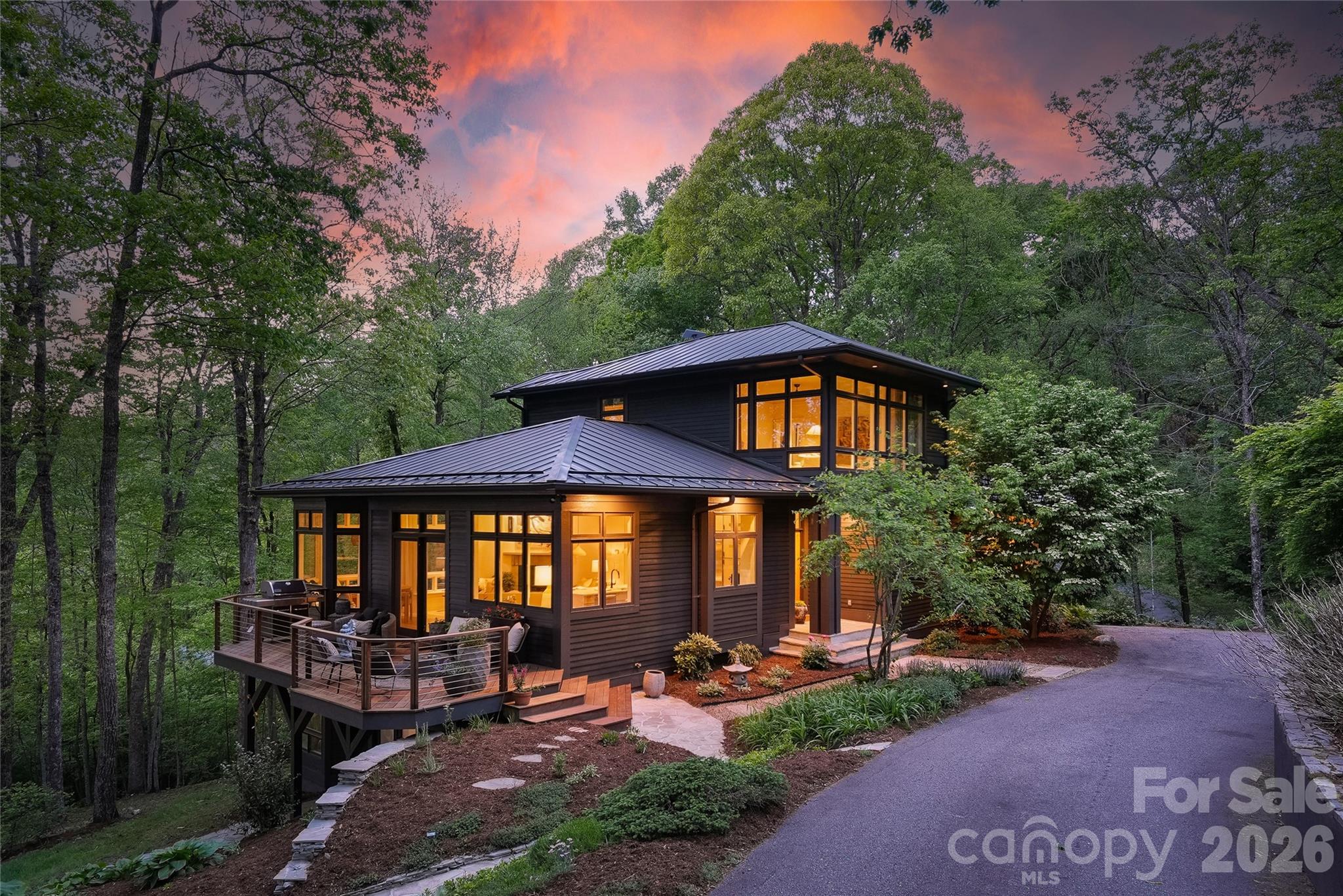 Tucked into over two private acres in the coveted Elk Mountain corridor, this custom residence is a rare convergence of intentional design, natural beauty, and elevated living. Fully reimagined by an interior designer, every element has been thoughtfully curated—layering handmade tile, natural stone, and bespoke finishes into a home that feels both grounded and refined. Thoughtfully designed, the home is positioned perfectly to capture the long-range sunset views from multiple vantage points - including the living room, kitchen, dining, primary suite and all 3 outdoor living spaces.

The main level unfolds with an effortless flow between living, dining, and a chef’s kitchen anchored by a Wolf range, Sub-Zero refrigeration, and striking quartzite surfaces. A guest suite or secondary primary just off the foyer, along with a walk-in pantry and laundry, offers true main-level living without compromise.

Upstairs, a dedicated primary retreat feels like a sanctuary—complete with dual walk-in closets and a spa-inspired bath designed for restoration. The lower level extends the experience with two additional bedrooms, a custom theater, wet bar, and a fully realized wellness suite featuring a sauna and cold plunge. 

Expansive Ipe hardwood decking spans all three levels, inviting year-round connection to the landscape. Designed by a landscape architect, the grounds are a living tapestry of native plantings, perennials, and edible herbs—recognized as a certified pollinator habitat, butterfly garden, and wildlife sanctuary. A gentle creek winds through the property, while long-range views, filtered morning light, and unforgettable sunsets create a dynamic natural backdrop.

Additional features include an elevator servicing all three levels, a standing seam metal roof, and a whole-house generator supported by a buried 1,000-gallon propane tank—capable of sustaining the home for extended periods.

Located just moments from the Blue Ridge Parkway and less than 15 minutes to downtown Asheville, this property offers the rare balance of seclusion and accessibility. With access to miles of neighborhood trails and preserved green space, 15 Hunters Way is more than a home—it’s an experience, intentionally crafted.