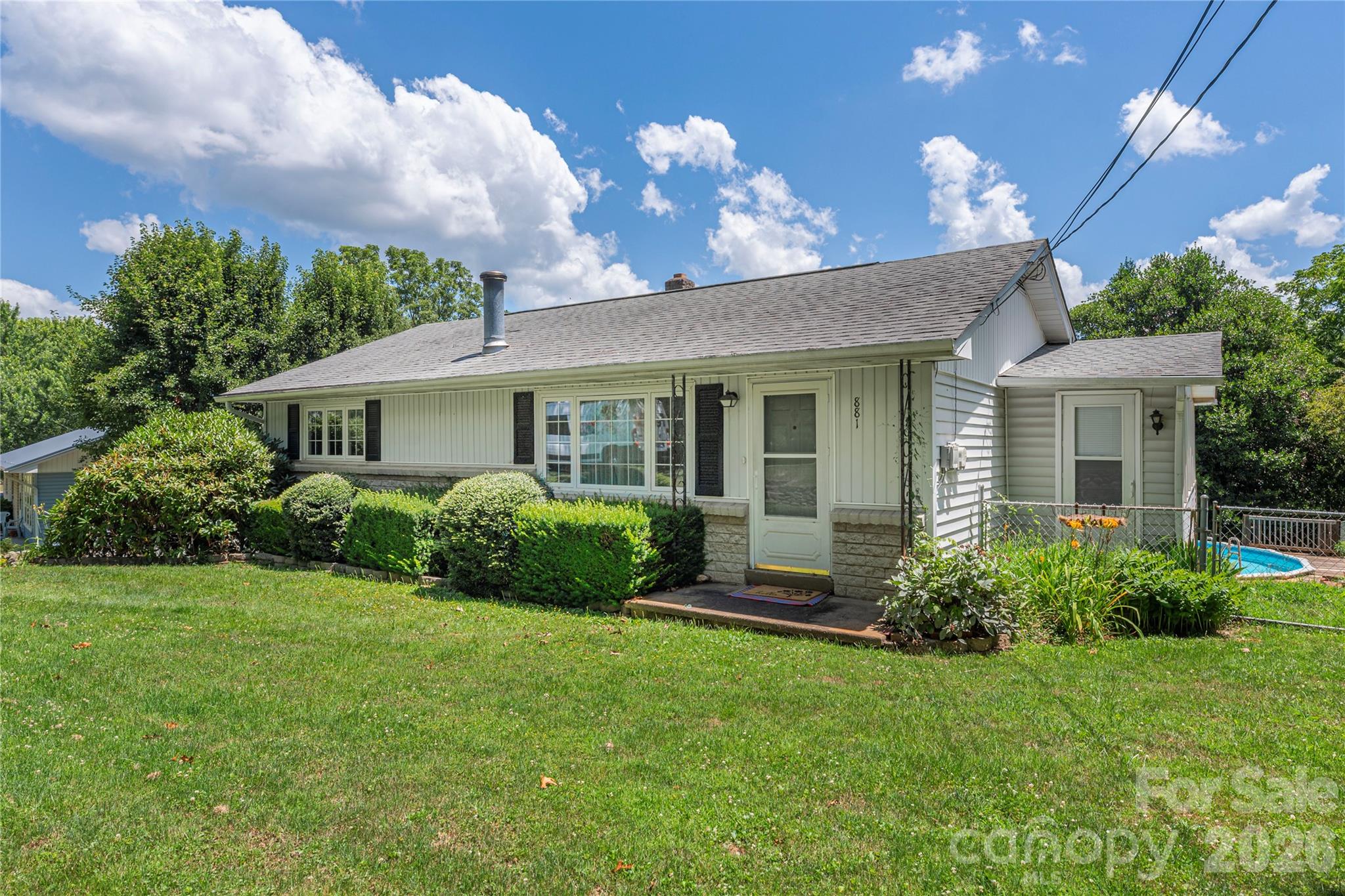 Welcome home to this charming gem in the heart of Clyde! Nestled on a level 0.34-acre lot, this thoughtfully redesigned 2-bedroom, 1-bath home offers comfortable one-level living with the added bonus of a full walk-out basement, providing exceptional storage and flexible space.

Inside, you'll find an inviting living space featuring laminate plank flooring over original hardwood floors throughout, with LVP flooring in the kitchen and vinyl tile in the enclosed back porch/sunroom. Insulated windows and cozy living areas complete with a gas log fireplace insert and wood-burning stove create the perfect setting for relaxing year-round. The kitchen comes equipped with an electric range, oven, microwave, and refrigerator, making this home move-in ready.

The above-grade walk-out basement features new carpet and offers endless possibilities for a recreation room, hobby space, home gym, or additional storage. Step outside to enjoy the enclosed porch and patio overlooking a fully fenced backyard complete with an above-ground pool—an ideal setting for summer fun, entertaining, pets, gardening, or simply relaxing outdoors.

Parking is plentiful with an attached 1-car garage, a detached 2-car carport with electricity and excellent workshop potential, and a paved asphalt driveway.

Enjoy the convenience of city water, central air, multiple heating options (oil, propane, and wood stove), and a publicly maintained paved road.

Conveniently located just minutes from the Town of Clyde, you'll enjoy quick access to local restaurants, shopping, schools, and everyday amenities while remaining a short drive to Waynesville, Canton, and the endless outdoor recreation of Western NC.