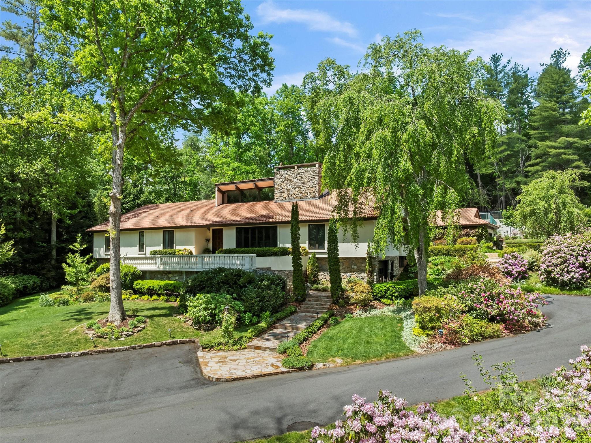 Nestled along the prestigious border of the Biltmore Estate, 69 Forest Road is an oasis of comfort and privacy situated on 1.88 acres of meticulously landscaped grounds and perennial gardens. This 6-bedroom, 6-bathroom sanctuary offers an unparalleled outdoor lifestyle, featuring a heated swimming pool centered between a massive rear patio and a fully equipped outdoor kitchen. Located above the pool area, find tennis and pickleball courts plus a basketball practice area, complemented by a fenced garden patch for cultivating fresh berries and vegetables. Inside, the home exudes warmth, highlighted by an oak-paneled Great Room with vaulted wood-beam ceilings, a wet bar, and original chandeliers from the historic Battery Park Hotel. A dual-sided wood-burning fireplace anchors both the Great Room and the vaulted dining room, creating a seamless flow for grand entertaining. The chef’s kitchen is a culinary dream with custom cabinetry and a large quartz center island, while a cozy gas-fired den offers a quiet retreat nearby. The main-floor primary suite is a true oasis, recently updated with new marble flooring in the bathroom and boasting three walk-in closets, a dressing room, a sunken tub, and a steam bath shower. A heated sunroom off the primary with outdoor access provides ideal storage for winter plants. The home includes two offices: an upper-level private office and a main-level smaller office just off the primary suite. An additional two suites on the lower level are each comprised of a bedroom, bath, and living room. Many system upgrades have been made throughout, including a 22KW generator and tankless water heaters for added comfort. A detached two-car garage off the main level and an additional basement garage complete an estate that offers a rare and sophisticated combination of space, amenities, and prestige.