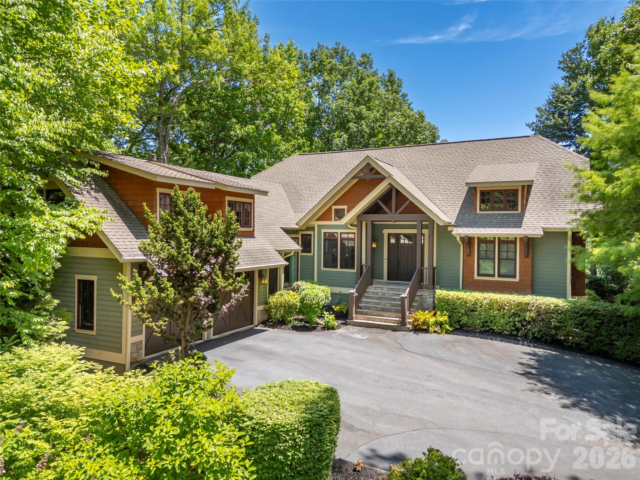 Perched above Tom Fazio’s signature 13th hole, 161 Chattooga Run captures the essence of mountain golf course living within Champion Hills, Hendersonville’s premier golf community. Thoughtfully crafted by respected builder Mike McDermott and later enhanced by renowned builder Paul Taylor, this home blends timeless craftsmanship with inviting spaces designed for gathering, relaxation, and enjoying the beauty of Western North Carolina.
From the moment you arrive, the setting feels special. Tucked into a private homesite with stair-step views overlooking holes #13 and portions of #12, the property offers a rare sense of seclusion with no neighboring homes in sight. Lush landscaping, layered outdoor living areas, and the peaceful sound of water create a true mountain retreat atmosphere.

At the heart of the home, the great room opens effortlessly onto the rear patio where summer dinner parties, evening cocktails, and quiet mornings become part of everyday life. A double-sided fireplace adds warmth and ambiance both indoors and out, while the adjacent side deck overlooks one of the property’s most captivating features—a stunning approximately 37-foot waterfall designed and maintained by Water Dance, featuring 12 individual cascades that blend naturally into the landscape.

The kitchen and dining spaces are warm, functional, and rich with custom details, including thoughtfully designed built-ins and elegant pullout serving boards that add charm and practicality. Just beyond, the temperature-controlled sunroom an addition completed in 2016 provides the perfect setting for morning coffee, reading, birdwatching, or catching up with friends while surrounded by natural light and tranquil views.
The 2016 addition by Paul Taylor also transformed the detached garage into an attached garage through an enclosed breezeway and created a spacious suite above the garage complete with a full bath, closet, and storage. Whether used as a guest suite, office, media room, or private retreat, the flexibility enhances the home’s livability.

Designed for entertaining and relaxed mountain living, the lower level offers inviting spaces for game nights, wine tastings, and gatherings around the custom wine cellar with its beautifully arched handcrafted door. Guest suites, walkout access to the outdoors, and a golf cart garage complete this exceptional mountain retreat.

With 3–4 bedrooms depending on lifestyle needs, exceptional privacy, curated outdoor living, and direct connection to Champion Hills’ celebrated golf course lifestyle, 161 Chattooga Run offers a rare opportunity to enjoy mountain living in comfort, elegance, and style just minutes from Hendersonville’s charming downtown, dining, shopping, hiking, and cultural attractions.
