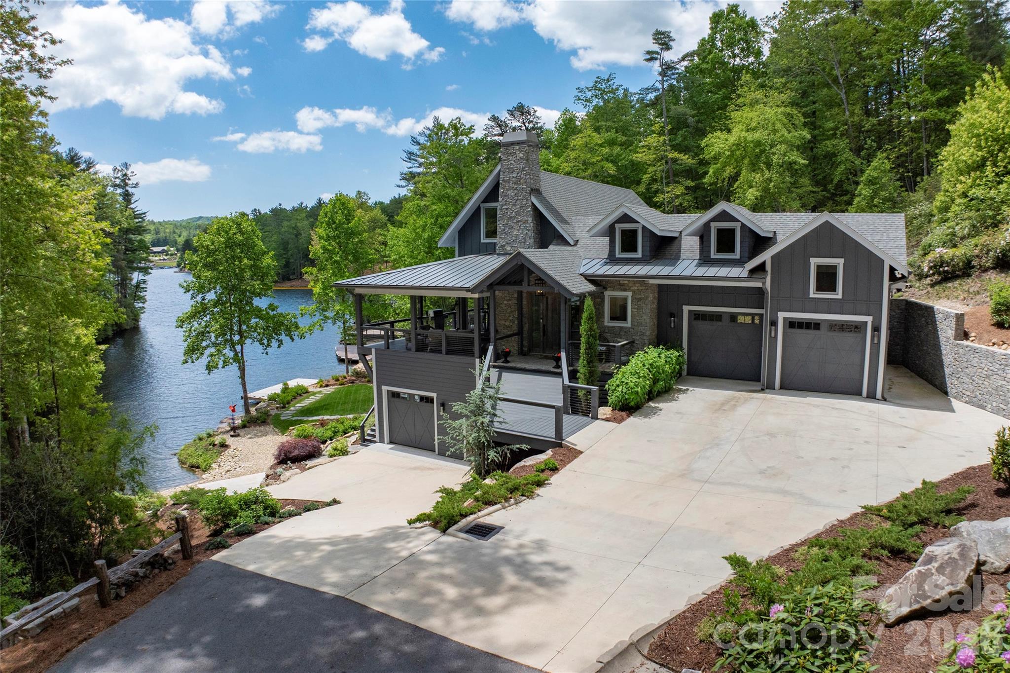 Nestled along the pristine shores of Lake Toxaway, this extraordinary custom-designed lakefront residence, completed in 2022, blends refined mountain-modern architecture with exceptional craftsmanship and luxurious amenities. Designed to maximize breathtaking water views and seamless indoor-outdoor living, the home features expansive walls of glass, an open-concept floor plan, and soaring cathedral ceilings accented by exposed wooden beams and a dramatic floor-to-ceiling stone fireplace in the great room coupled with folding glass doors that seamlessly extends the living area from inside to out.
The living room opens completely to the exterior porch through retractable doors, creating an inviting entertainment space that effortlessly connects the home to the surrounding landscape and tranquil lakefront setting. Three fireplaces located in the living room, covered porch, and recreation room provide warmth and ambiance throughout the home.
Every detail was thoughtfully curated, from the custom-designed front door crafted from reclaimed aged barn wood to the elegant 8-foot interior doors adorned with Emtek oil-rubbed bronze hardware from the Hercules Collection. The gourmet kitchen boasts Dolomite Marble countertops and is equipped with premium Bosch and Thermador appliances, while Italian tile and marble enhance the spa-inspired bathrooms featuring curb less showers and illuminated mirrors with adjustable color and brightness controls.
Designed for comfort and convenience, the home includes laundry rooms on each floor, hand-scraped and brushed European White Oak engineered hardwood flooring in a sophisticated Grey Mist finish, and a fully encapsulated crawl space with dehumidification. Advanced lighting features include an abundance of 4-inch hi-hats, automatic closet lighting, stair step illumination, exterior landscape lighting, and power service extending to both the driveway and private dock.
Built with superior efficiency, durability, and convenience in mind, the home features 2x6 exterior walls with full insulation, spray foam attic insulation, and a robust 400-amp electrical service. Plumbing amenities include dual-zone propane recirculating instant hot water systems, six frost-free exterior hose bibs, and premium Grohe, Moen, and Kohler fixtures throughout. The bathroom off the downstairs rec room is a Cabana Bath that features a very convenient outdoor shower.
Heating and cooling are equally impressive, with two complete Trane 18-SEER HVAC systems serving the upper and lower levels, including gas furnace and humidification on the main floor, Wi-Fi-enabled thermostats, and a Mitsubishi ductless heating and cooling system in the studio space.
Outside, a private dock provides effortless access to boating and lake activities, while the adjacent lakeside lawn offers the perfect setting for entertaining, family gatherings, and outdoor recreation. A security system and whole-home water purification system complete this remarkable turnkey lakefront retreat where luxury, comfort, and timeless design come together in one exceptional property.