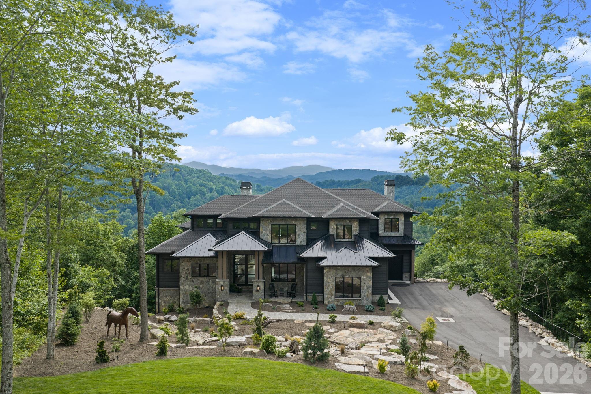 Welcome to Iron Horse Lodge, a newly constructed custom estate offering 8,817 square feet of heated living area within The Lodges at Eagles Nest, just minutes from downtown Banner Elk, Great Camp Amphitheater, and Epic Chophouse. Designed as a primary residence with an uncompromising approach to quality, the home showcases refined mountain-modern architecture with natural stone, horizontal wood siding, architectural shingles, standing seam metal accents, timber columns, and Edge Vesta steel siding in select hard-to-reach areas for added durability. A custom-engineered steel beam foundation allows for a cantilevered design over the mountainside, maximizing structural integrity and long-range Blue Ridge Mountain views. An easily accessible driveway provides ample guest parking, complemented by an oversized two-car garage and an additional single-car garage. A thoughtfully designed mudroom with built-in laundry, drop zone, and custom dog wash adds everyday function. Inside, oversized glass barn-style doors open to a welcoming foyer and wine/cocktail lounge. A dedicated office with custom architectural doors leads into an expansive living and dining area, where fully retractable glass doors connect to a sprawling deck with sunset views. The chef’s kitchen features Thermador Professional Series appliances, dual dishwashers, a wet bar/coffee station with sink and refrigerated drawers, and a well-appointed butler’s pantry with built-in desk, storage, and prep space. The main-level primary suite offers a fireplace, coffee bar, beverage fridge, sink, expansive mountain views, and direct deck access to a Bullfrog 6+ person hot tub. The spa-like bath includes a soaking tub, dual-head shower, double vanities, and a walk-in closet with its own washer and dryer. Upstairs, a second en suite bedroom is joined by an additional bedroom with nursery, hidden door access, and spacious walk-in closet. A large shared bath offers a soaking tub and dual-head shower, while a covered deck captures elevated views. The lower level expands the home’s lifestyle offerings with a spacious family room, bunkroom suite with full bath, gym, half bath, wellness room with cold plunge and infrared sauna, theater room, and additional heated flex space. A partially covered deck extends the living area outdoors for quiet mornings, cool summer afternoons, and year-round mountain enjoyment. Offered fully furnished with select exclusions, Iron Horse Lodge presents a rare opportunity to own a move-in ready, professionally designed mountain retreat without the wait. Interior design by Lucy and Company delivers a bold, curated aesthetic recognized for its presence in luxury publications.