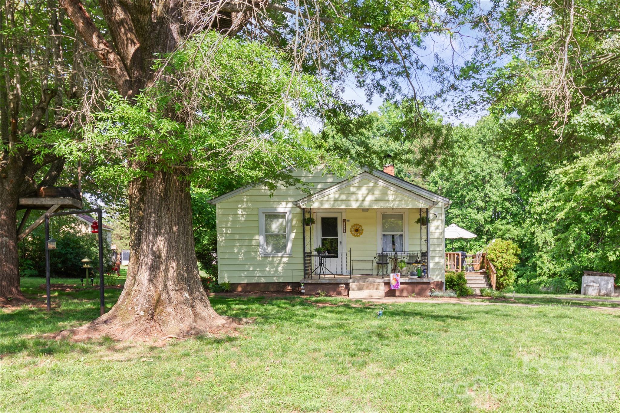 Welcome home to this charming bungalow nestled on a spacious nearly 3/4-acre cleared lot, offering room to relax, garden, play, or simply enjoy the peaceful setting surrounded by mature trees. A covered front porch creates a welcoming first impression and leads into a cozy home filled with character and thoughtful updates, including a keypad entry lock and storm door. Inside, the living room features a decorative brick fireplace, ceiling fan, and a classic arched opening that connects the space to the kitchen and dining area. The kitchen offers an abundance of cabinetry and countertop space for a home of this size, plus open shelving for added charm and functionality. The refrigerator conveys for added convenience. Two bedrooms share a spacious full bath with a tub/shower combination and additional storage cabinet. At the rear of the home, the large mudroom provides valuable flex space and doubles as a laundry area with washer and electric dryer hookups. Step outside to enjoy the back deck, perfect for relaxing or entertaining, with a metal awning providing cover over the back entry. The expansive backyard also includes a 10x10 storage shed for tools, hobbies, and outdoor essentials. With its generous lot, mature surroundings, and inviting bungalow character, this home offers a wonderful opportunity to enjoy a quieter pace of life while still being close to area conveniences.