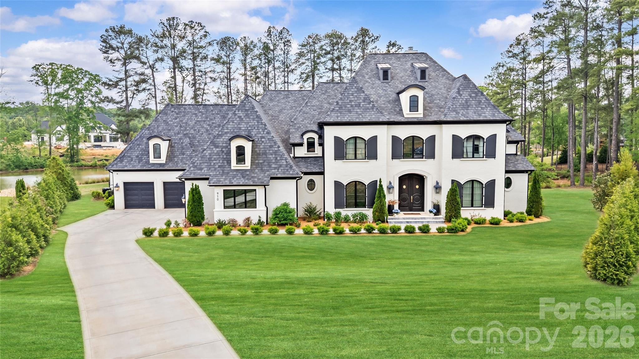 Why wait to build when your dream home is move in ready now? This exceptional lakefront estate, built in 2023, is perfectly positioned on 1.36 acres in Weddington’s premier Twin Lakes community, offering breathtaking water views, over 6,100  square feet of thoughtfully designed living space and fabulous pool house. Crafted for both everyday living and elevated entertaining, this 4-bedroom, 5.5-bath home showcases designer finishes and custom details throughout. The light-filled, open floor plan features soaring ceilings and seamless indoor-outdoor flow. At the heart of the home, the gourmet kitchen impresses with an oversized waterfall island, professional-grade appliances, and floor-to-ceiling cabinetry, complemented by a fully equipped scullery with double ovens, prep sink, dishwasher, and abundant storage. The main-level primary suite is a private retreat, offering a spa-inspired bath, sauna, three custom walk-in closets, and a dedicated laundry room. A striking navy study with built-ins provides the perfect work-from-home space. The inviting family room features a full-length accordion glass door and retractable screens, creating effortless year-round indoor-outdoor living. Upstairs, dual staircases lead to three spacious bedrooms, each with ensuite baths and custom walk-in closets, along with a bonus room, fitness/playroom, loft, additional laundry, and two oversized walk-in storage areas. Outdoor living is truly resort-inspired, with two covered patios, fireplace, firepit, outdoor kitchen, and a stunning saltwater pool with spa overlooking the lake. The pool house enhances the experience with a wet bar, recreation room, and full bath—perfect for hosting friends and family. Additional features include garage space for up to four cars, ample storage, and a well-designed drop zone for everyday organization. Residents of Twin Lakes enjoy resort-style amenities including scenic walking trails, a waterfront gazebo, championship pickleball courts, and a community dock for kayaking, canoeing, and paddleboarding. A rare opportunity to own a nearly new, lakefront luxury home with exceptional design, function, and lifestyle.