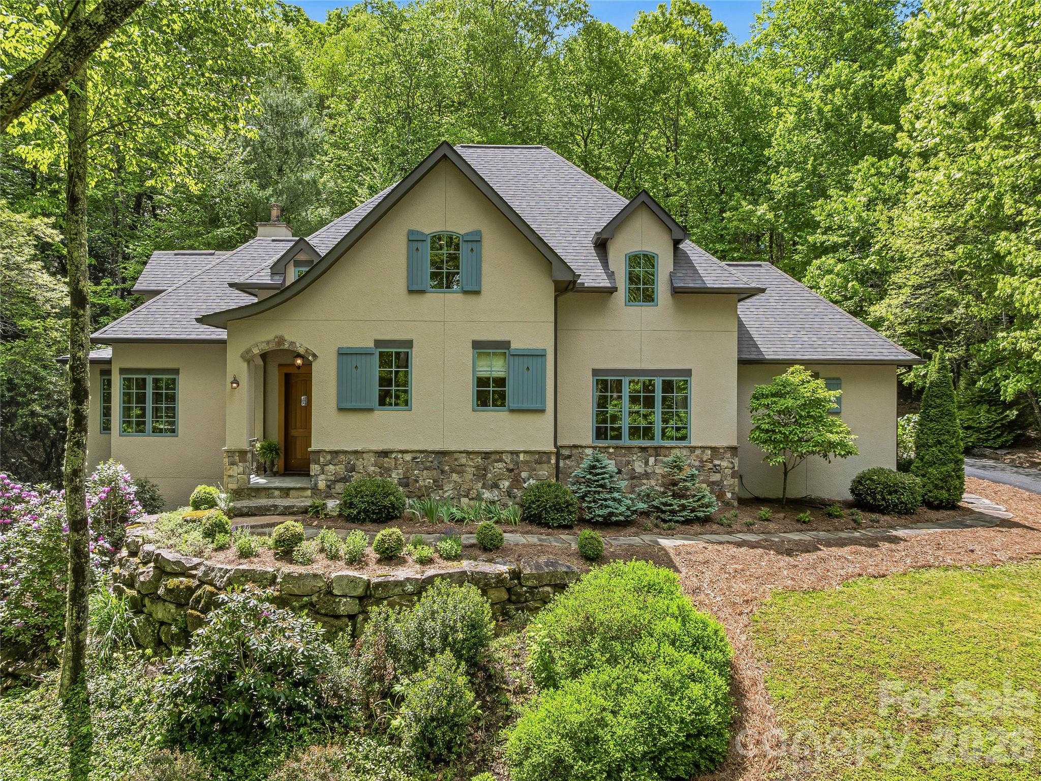 Located in the premier gated enclave of Avery Park, just 10 minutes from South Asheville, this French Country, custom-built home strikes a delicate balance between rustic elegance and modern functionality. The design emphasizes Old World authenticity, anchored by a two-story vaulted ceiling, artisanal millwork, exposed wooden beams, wrought-iron chandeliers, and exquisite hardwood floors. Tall, paned casement windows overlook lush mountain laurel and blooming rhododendrons. A masterclass in culinary design, the chef’s kitchen boasts a massive 32-square-foot granite island, custom cabinetry, a KitchenAid Pro range, and a large walk-in pantry. The versatile floor plan features two bedrooms on the main floor—including the primary suite—and a screened-in porch with a gas fireplace. Upstairs, you'll find a truly lovely, airy family room, plenty of easily accessed storage, and two bedrooms that share a shower-tub space but have separate entrances, vanities, and water closets. For effortless peace of mind, smart home integration allows for remote monitoring of security and water management from anywhere. Avery Park residents enjoy direct access to Pisgah National Forest trails alongside community swimming and a sports court for tennis and pickleball.