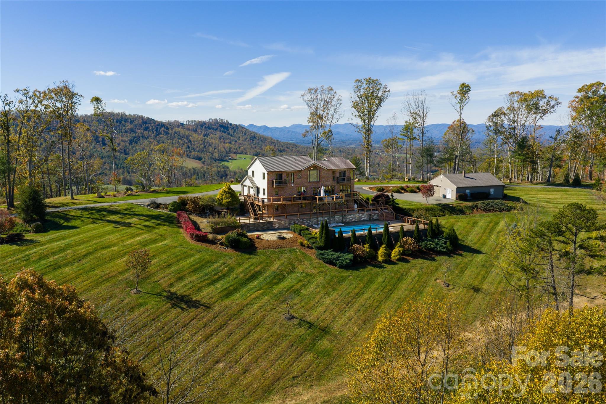 Welcome to 83 Cozy Mountain Lane, a private gated mountain estate encompassing approximately 26.93 acres in the Blue Ridge Mountains and offering a rare blend of refined mountain living, expansive scale and exceptional 360-degree views. Ideally just minutes from downtown Weaverville and approximately 15 minutes from Asheville, the property provides convenient access to dining, arts and culture while remaining close to outdoor destinations including the Blue Ridge Parkway and Pisgah National Forest. Anchored by a thoughtfully positioned residence spanning approximately 4,963 square feet, the estate captures sweeping long-range mountain views from the moment you enter the driveway and carries them through nearly every room. A striking great room with a stone gas fireplace sets the tone upon entry, seamlessly flowing into a light-filled living area framed by expansive picture windows. From here, enter onto the Trex deck with a gas fire pit overlooking the resort-style in-ground pool, patio and custom stone fire pit, creating an exceptional setting for year-round entertaining. The kitchen serves as the heart of the home, featuring a suite of KitchenAid appliances, including a wall oven, microwave, five-burner gas cooktop and refrigerator, complemented by a Bosch dishwasher. Leathered granite countertops, a large island, stainless apron-front sink and under-cabinet lighting balance function with understated luxury. A dedicated office, integrated speakers and a well-appointed mudroom and laundry suite complete a main level designed for comfort and practicality. Upstairs, the primary suite offers a private retreat with vaulted ceilings, transom windows and a Juliet balcony overlooking the pool and surrounding mountains. The spa-inspired bath features a freestanding soaking tub positioned before a picture window, dual marble vanities and a spacious walk-in shower with pebble stone flooring and refined stone accents. Two additional guest bedrooms, a full bath and a loft living area complete the upper level. The lower level expands the home's versatility with full secondary living quarters, including a recreation room, living room with wood-burning stove, complete kitchen with stainless appliances, dining area, guest bedroom and full bath. Dedicated systems, including dual water heaters and mini-split climate control, make this space ideal for guests, extended stays or flexible living arrangements. A detached, fully climate-controlled outbuilding/garage provides additional space for vehicles, hobbies, fitness, creative pursuits or a private office. Beyond the residence, the estate's rarity unfolds across the combined 26.93 acres, including an adjoining 17.78-acre parcel now offered as part of the property. This exceptional tract features a stunning, largely level building site positioned to capture breathtaking long-range mountain views, creating a unique opportunity for a guest house, family compound, additional residence or future estate expansion. Rarely found in the mountains of Western North Carolina, the land combines privacy, usability and remarkable view corridors, with gently rolling ridge-top terrain offering ample space for recreation, gardens, hobby farming or creation of a legacy property. Offering an extraordinary combination of acreage, privacy, proximity, usable land and commanding mountain views, 83 Cozy Mountain Lane presents a rare opportunity to own a mountain estate of exceptional scale and potential.